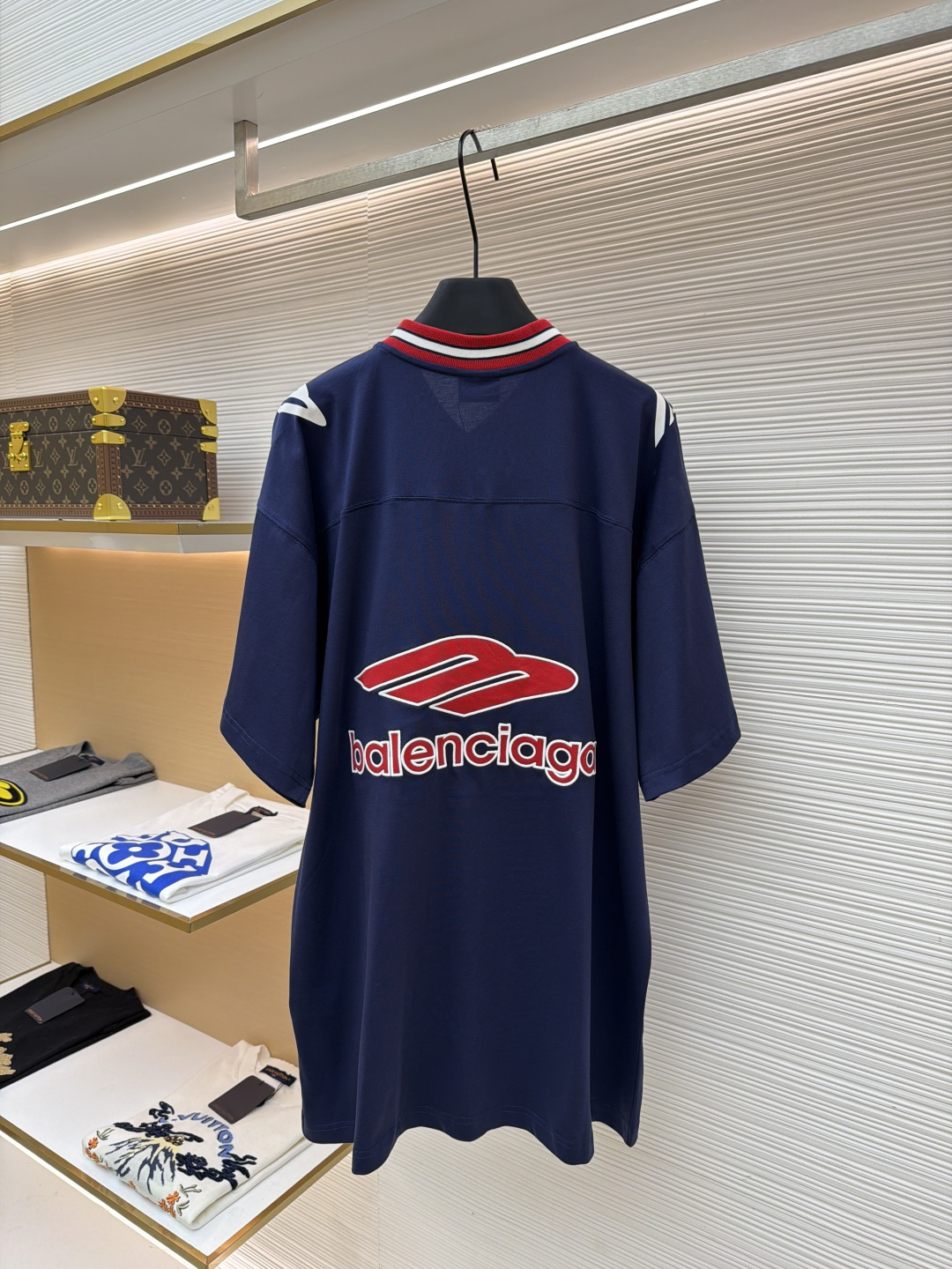 P180 Balenciaga 球队系列V领长袖
●原版：5699购入开发
●货号：1682041-A50
●面料：平纹针织紧密棉面料
●工艺：胶浆印花制作
●颜色：蓝色
●版型：宽松版型
●克重：约300克
●尺码：XS-S-M-L
●描述：主体采用24支特纺紧密棉，克重为185g/㎡。在纺纱环节应用了紧密纺技术，显著减少了纱线毛羽，使得纱线更光滑、强韧。这赋予了面料结构异常密实、表面光洁平整、抗起球性优异的特点，同时保留了纯棉的柔软透气性。185g的克重属于轻至中量级，确保了衣物轻盈、垂坠且活动自如的特性，非常适合打造兼具运动感与日常舒适度的长袖衫。V领部分由两种不同颜色的高弹罗纹面料拼接而成。其工艺步骤是先分别织造出两种颜色的罗纹带，再通过精准的剪裁与拼接，形成具有鲜明色彩对比的V形领口。打破了纯色衣身的单调，以强烈的色彩对比塑造出年轻、活力的视觉焦点，并优化了颈部线。将图案在不同材质或颜色的布料上预先裁剪成型贴布，然后将其覆盖在衣身上，最后用高密度绣线锁边固定并勾勒内部细节。其作用在于：创造色彩鲜明、质感对比强烈且极具立体感和耐用性的图案，图案边缘牢固，不易磨损。将特制的弹性浆料通过网版印刷在袖部的工艺，色彩鲜艳且具有轻微涂层感的图案。弹力浆料保证了印花区域能随面料一起拉伸而不开裂。与贴布绣的立体感形成一平一凸的质感对比，增加了设计的趣味性和复杂度。整体走线平直细腻，面料舒适柔软，颜色一致无色差 能与同款搭配营造时尚造型，驾驭各种场合，定制辅料，三标齐全，男女同款！