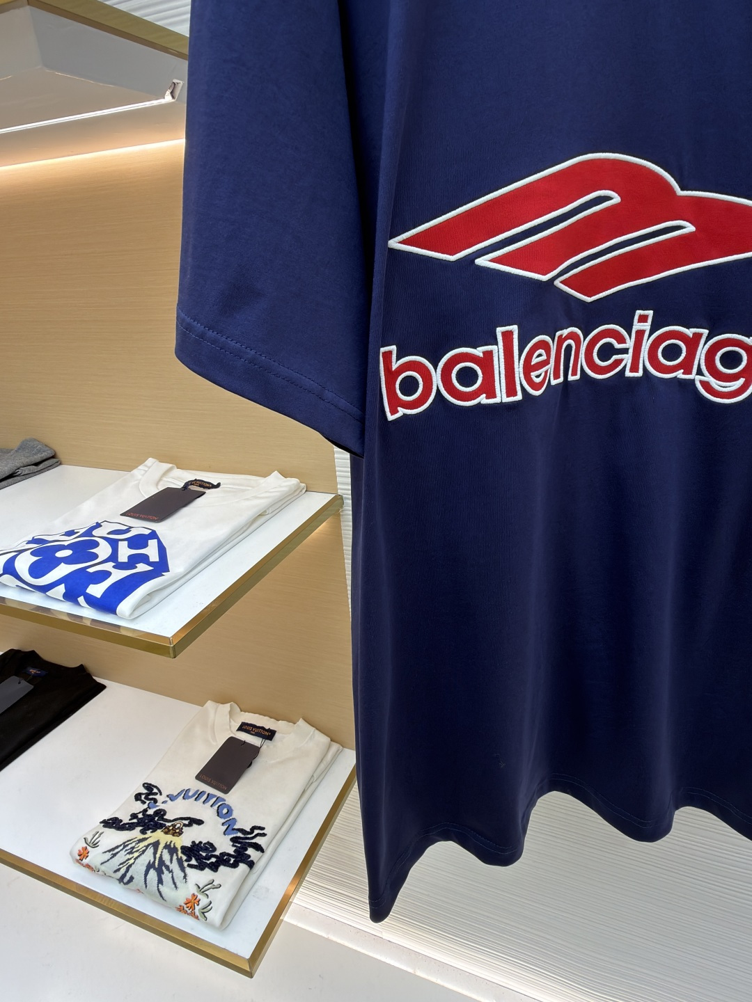 P180 Balenciaga 球队系列V领长袖
●原版：5699购入开发
●货号：1682041-A50
●面料：平纹针织紧密棉面料
●工艺：胶浆印花制作
●颜色：蓝色
●版型：宽松版型
●克重：约300克
●尺码：XS-S-M-L
●描述：主体采用24支特纺紧密棉，克重为185g/㎡。在纺纱环节应用了紧密纺技术，显著减少了纱线毛羽，使得纱线更光滑、强韧。这赋予了面料结构异常密实、表面光洁平整、抗起球性优异的特点，同时保留了纯棉的柔软透气性。185g的克重属于轻至中量级，确保了衣物轻盈、垂坠且活动自如的特性，非常适合打造兼具运动感与日常舒适度的长袖衫。V领部分由两种不同颜色的高弹罗纹面料拼接而成。其工艺步骤是先分别织造出两种颜色的罗纹带，再通过精准的剪裁与拼接，形成具有鲜明色彩对比的V形领口。打破了纯色衣身的单调，以强烈的色彩对比塑造出年轻、活力的视觉焦点，并优化了颈部线。将图案在不同材质或颜色的布料上预先裁剪成型贴布，然后将其覆盖在衣身上，最后用高密度绣线锁边固定并勾勒内部细节。其作用在于：创造色彩鲜明、质感对比强烈且极具立体感和耐用性的图案，图案边缘牢固，不易磨损。将特制的弹性浆料通过网版印刷在袖部的工艺，色彩鲜艳且具有轻微涂层感的图案。弹力浆料保证了印花区域能随面料一起拉伸而不开裂。与贴布绣的立体感形成一平一凸的质感对比，增加了设计的趣味性和复杂度。整体走线平直细腻，面料舒适柔软，颜色一致无色差 能与同款搭配营造时尚造型，驾驭各种场合，定制辅料，三标齐全，男女同款！