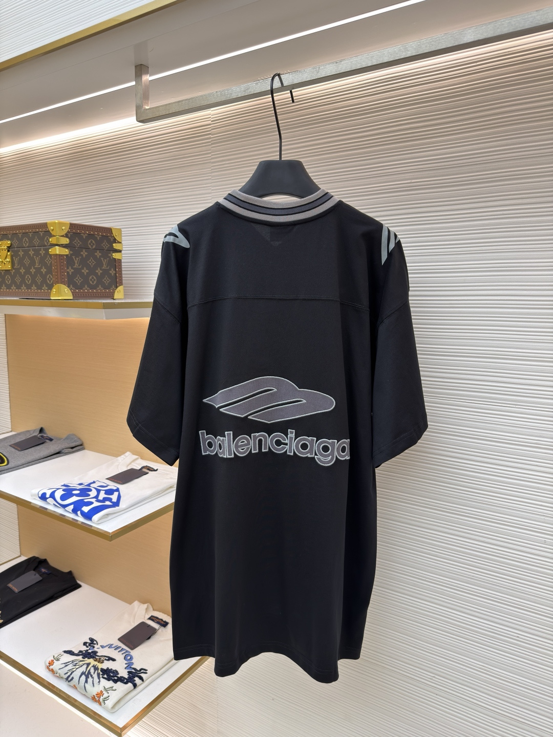 P180 Balenciaga 球队系列V领长袖
●原版：6898购入开发
●货号：1682042-A50
●面料：平纹针织紧密棉面料
●工艺：胶浆印花制作
●颜色：黑色
●版型：宽松版型
●克重：约310克
●尺码：XS-S-M-L
●描述：主体采用24支特纺紧密棉，克重为185g/㎡。在纺纱环节应用了紧密纺技术，显著减少了纱线毛羽，使得纱线更光滑、强韧。这赋予了面料结构异常密实、表面光洁平整、抗起球性优异的特点，同时保留了纯棉的柔软透气性。185g的克重属于轻至中量级，确保了衣物轻盈、垂坠且活动自如的特性，非常适合打造兼具运动感与日常舒适度的长袖衫。V领部分由两种不同颜色的高弹罗纹面料拼接而成。其工艺步骤是先分别织造出两种颜色的罗纹带，再通过精准的剪裁与拼接，形成具有鲜明色彩对比的V形领口。打破了纯色衣身的单调，以强烈的色彩对比塑造出年轻、活力的视觉焦点，并优化了颈部线。将图案在不同材质或颜色的布料上预先裁剪成型贴布，然后将其覆盖在衣身上，最后用高密度绣线锁边固定并勾勒内部细节。其作用在于：创造色彩鲜明、质感对比强烈且极具立体感和耐用性的图案，图案边缘牢固，不易磨损。将特制的弹性浆料通过网版印刷在袖部的工艺，色彩鲜艳且具有轻微涂层感的图案。弹力浆料保证了印花区域能随面料一起拉伸而不开裂。与贴布绣的立体感形成一平一凸的质感对比，增加了设计的趣味性和复杂度。整体走线平直细腻，面料舒适柔软，颜色一致无色差 能与同款搭配营造时尚造型，驾驭各种场合，定制辅料，三标齐全，男女同款！