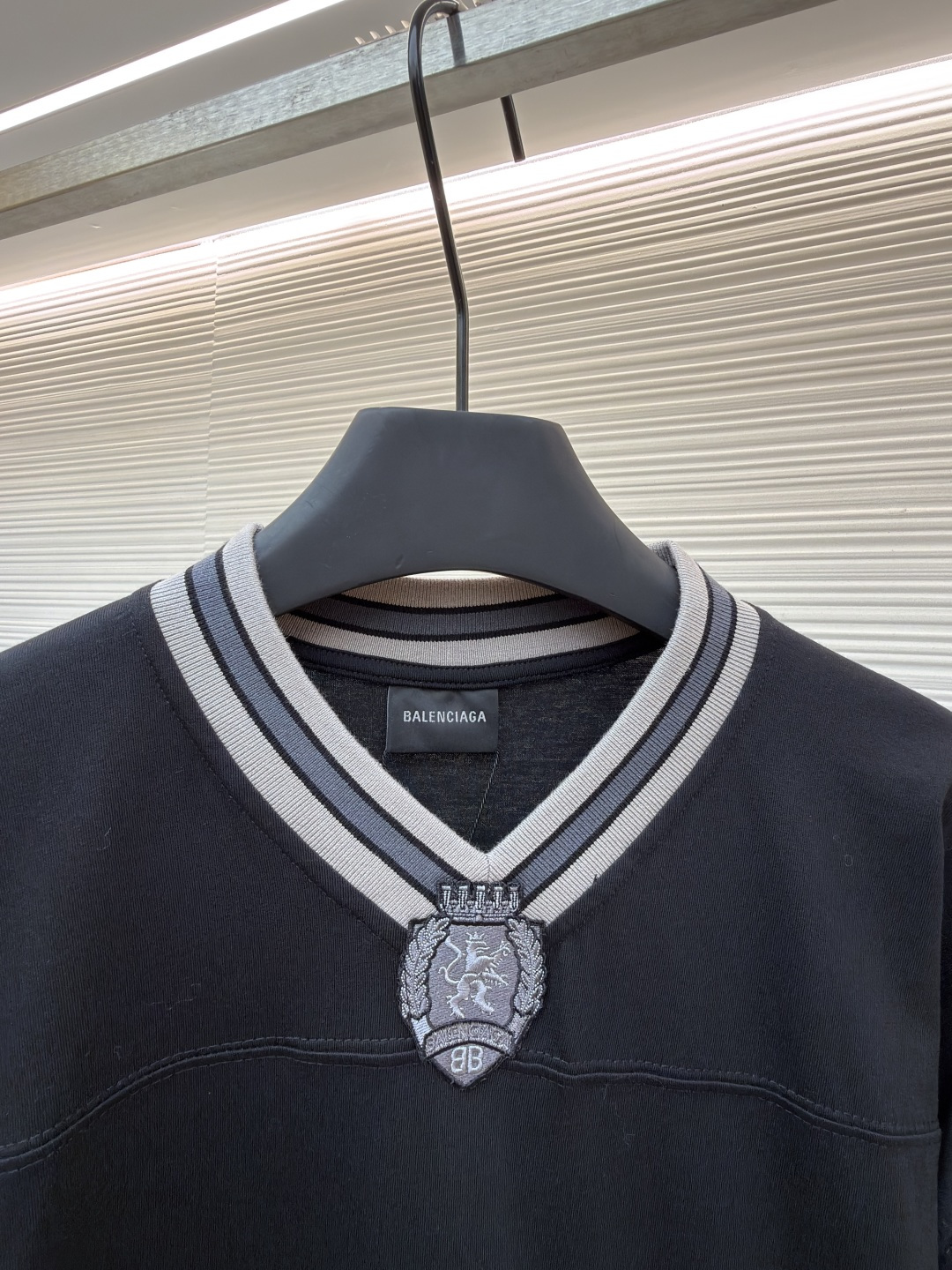 P180 Balenciaga 球队系列V领长袖
●原版：6898购入开发
●货号：1682042-A50
●面料：平纹针织紧密棉面料
●工艺：胶浆印花制作
●颜色：黑色
●版型：宽松版型
●克重：约310克
●尺码：XS-S-M-L
●描述：主体采用24支特纺紧密棉，克重为185g/㎡。在纺纱环节应用了紧密纺技术，显著减少了纱线毛羽，使得纱线更光滑、强韧。这赋予了面料结构异常密实、表面光洁平整、抗起球性优异的特点，同时保留了纯棉的柔软透气性。185g的克重属于轻至中量级，确保了衣物轻盈、垂坠且活动自如的特性，非常适合打造兼具运动感与日常舒适度的长袖衫。V领部分由两种不同颜色的高弹罗纹面料拼接而成。其工艺步骤是先分别织造出两种颜色的罗纹带，再通过精准的剪裁与拼接，形成具有鲜明色彩对比的V形领口。打破了纯色衣身的单调，以强烈的色彩对比塑造出年轻、活力的视觉焦点，并优化了颈部线。将图案在不同材质或颜色的布料上预先裁剪成型贴布，然后将其覆盖在衣身上，最后用高密度绣线锁边固定并勾勒内部细节。其作用在于：创造色彩鲜明、质感对比强烈且极具立体感和耐用性的图案，图案边缘牢固，不易磨损。将特制的弹性浆料通过网版印刷在袖部的工艺，色彩鲜艳且具有轻微涂层感的图案。弹力浆料保证了印花区域能随面料一起拉伸而不开裂。与贴布绣的立体感形成一平一凸的质感对比，增加了设计的趣味性和复杂度。整体走线平直细腻，面料舒适柔软，颜色一致无色差 能与同款搭配营造时尚造型，驾驭各种场合，定制辅料，三标齐全，男女同款！