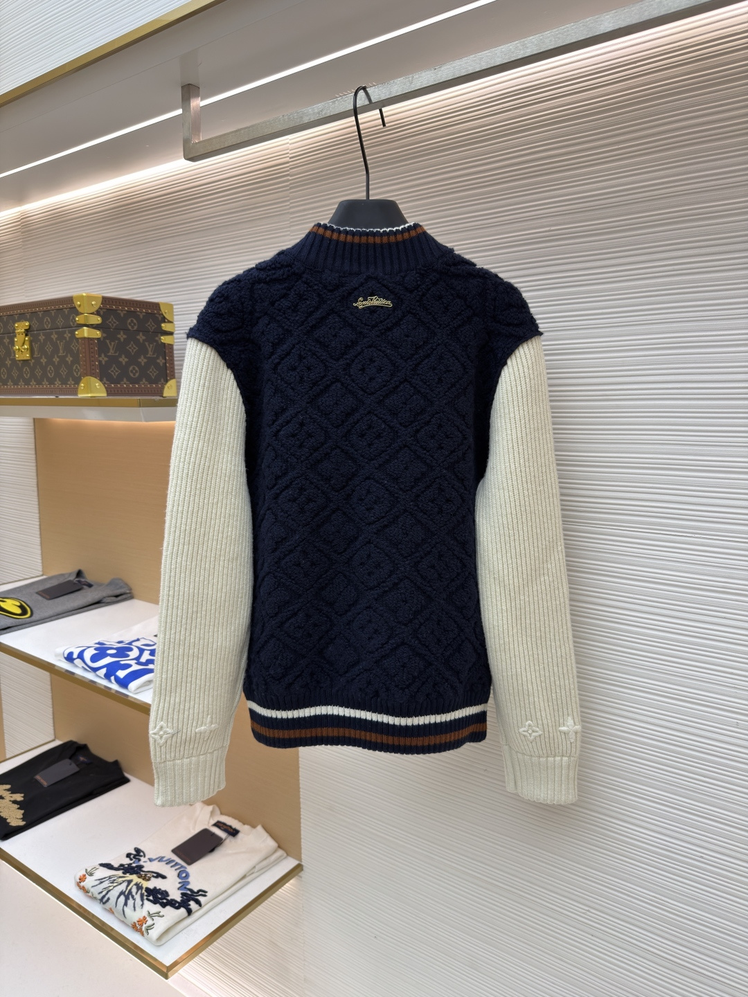 P815 LOUIS VUITTON SKI滑雪系列拼色条纹棒球长袖外套
●原版：22999购入开发
●面料：羊毛混纺面料
●工艺：针织制作
●颜色：蓝白
●版型：合身版型
●克重：约1070克
●尺码：XS-S-M-L
●描述：这款路易威登拼色针织开衫采用立体绞花编织工艺打造主体衣身，选用高支数美利奴羊毛混纺面料，通过双针床针织机织造出凹凸有致的菱格纹理，每平方厘米编织密度达32针，让纹理兼具立体感与柔软度；衣身主体为藏青色定纺纱线，经三次水洗固色处理，有效防止褪色。袖子部分采用米白色竖坑条罗纹针织，单股纱线捻度控制在800捻/米，保证回弹性与贴合度。金属按扣为定制黄铜材质，经镀金封釉工艺处理；领口、下摆的撞色罗纹采用嵌花编织，精准对接品牌经典三色织带比例，袖口处还暗藏激光雕刻的品牌标识，整体工艺融合传统针织技法与现代精工，细节处尽显匠造水准。整体走线平直细腻，面料舒适柔软，颜色一致无色差 能与同款搭配营造时尚造型，驾驭各种场合，定制辅料，三标齐全，男女同款！