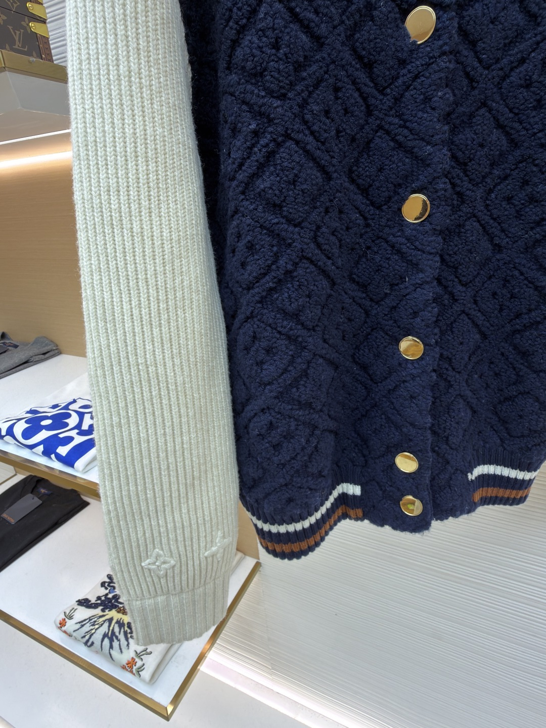 P815 LOUIS VUITTON SKI滑雪系列拼色条纹棒球长袖外套
●原版：22999购入开发
●面料：羊毛混纺面料
●工艺：针织制作
●颜色：蓝白
●版型：合身版型
●克重：约1070克
●尺码：XS-S-M-L
●描述：这款路易威登拼色针织开衫采用立体绞花编织工艺打造主体衣身，选用高支数美利奴羊毛混纺面料，通过双针床针织机织造出凹凸有致的菱格纹理，每平方厘米编织密度达32针，让纹理兼具立体感与柔软度；衣身主体为藏青色定纺纱线，经三次水洗固色处理，有效防止褪色。袖子部分采用米白色竖坑条罗纹针织，单股纱线捻度控制在800捻/米，保证回弹性与贴合度。金属按扣为定制黄铜材质，经镀金封釉工艺处理；领口、下摆的撞色罗纹采用嵌花编织，精准对接品牌经典三色织带比例，袖口处还暗藏激光雕刻的品牌标识，整体工艺融合传统针织技法与现代精工，细节处尽显匠造水准。整体走线平直细腻，面料舒适柔软，颜色一致无色差 能与同款搭配营造时尚造型，驾驭各种场合，定制辅料，三标齐全，男女同款！