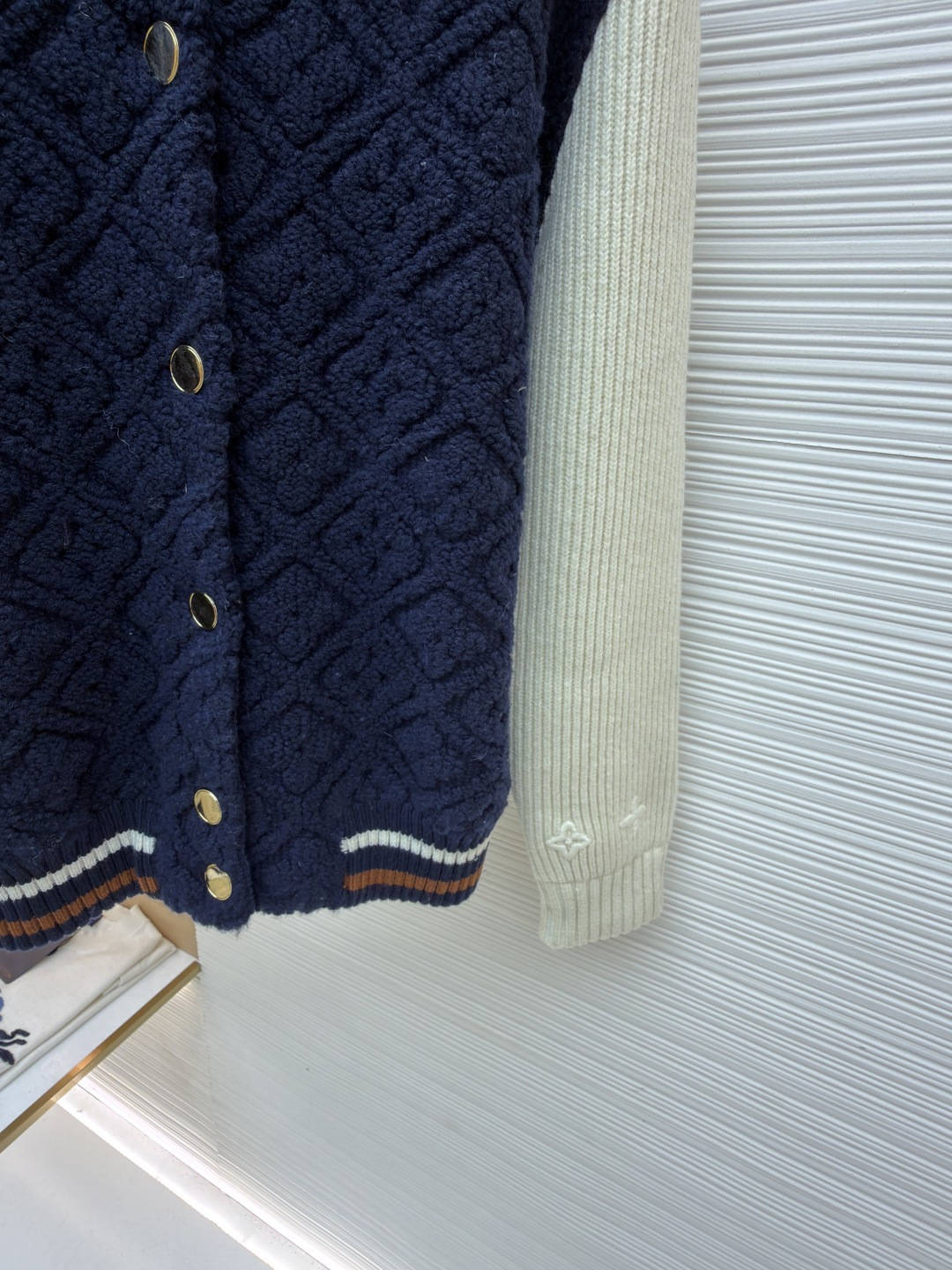 P815 LOUIS VUITTON SKI滑雪系列拼色条纹棒球长袖外套
●原版：22999购入开发
●面料：羊毛混纺面料
●工艺：针织制作
●颜色：蓝白
●版型：合身版型
●克重：约1070克
●尺码：XS-S-M-L
●描述：这款路易威登拼色针织开衫采用立体绞花编织工艺打造主体衣身，选用高支数美利奴羊毛混纺面料，通过双针床针织机织造出凹凸有致的菱格纹理，每平方厘米编织密度达32针，让纹理兼具立体感与柔软度；衣身主体为藏青色定纺纱线，经三次水洗固色处理，有效防止褪色。袖子部分采用米白色竖坑条罗纹针织，单股纱线捻度控制在800捻/米，保证回弹性与贴合度。金属按扣为定制黄铜材质，经镀金封釉工艺处理；领口、下摆的撞色罗纹采用嵌花编织，精准对接品牌经典三色织带比例，袖口处还暗藏激光雕刻的品牌标识，整体工艺融合传统针织技法与现代精工，细节处尽显匠造水准。整体走线平直细腻，面料舒适柔软，颜色一致无色差 能与同款搭配营造时尚造型，驾驭各种场合，定制辅料，三标齐全，男女同款！