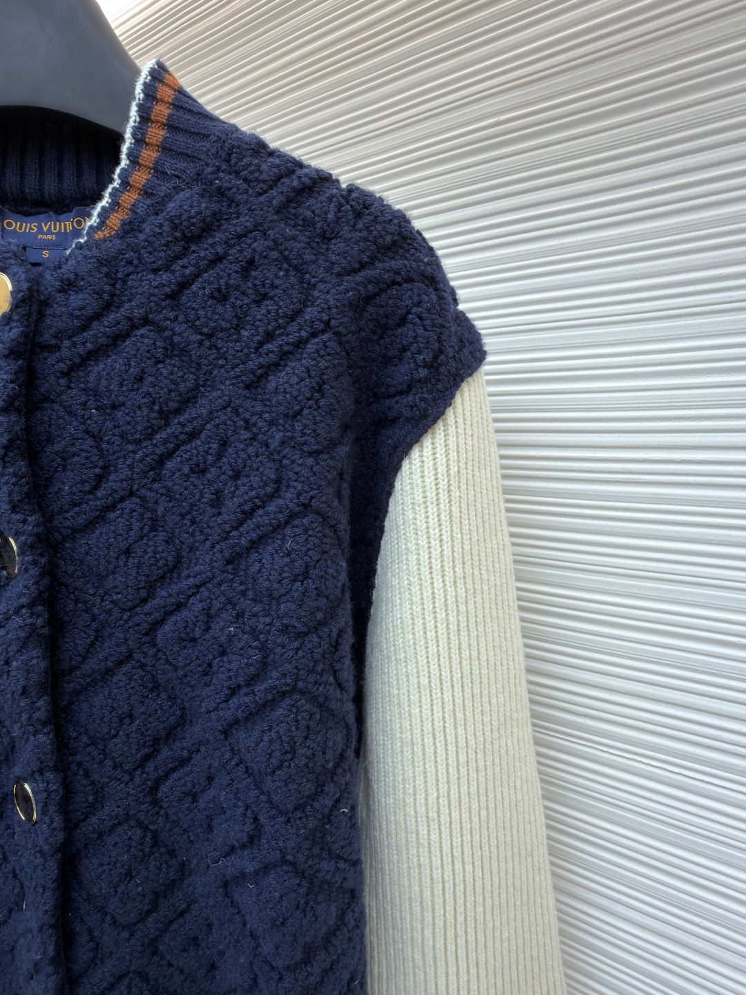 P815 LOUIS VUITTON SKI滑雪系列拼色条纹棒球长袖外套
●原版：22999购入开发
●面料：羊毛混纺面料
●工艺：针织制作
●颜色：蓝白
●版型：合身版型
●克重：约1070克
●尺码：XS-S-M-L
●描述：这款路易威登拼色针织开衫采用立体绞花编织工艺打造主体衣身，选用高支数美利奴羊毛混纺面料，通过双针床针织机织造出凹凸有致的菱格纹理，每平方厘米编织密度达32针，让纹理兼具立体感与柔软度；衣身主体为藏青色定纺纱线，经三次水洗固色处理，有效防止褪色。袖子部分采用米白色竖坑条罗纹针织，单股纱线捻度控制在800捻/米，保证回弹性与贴合度。金属按扣为定制黄铜材质，经镀金封釉工艺处理；领口、下摆的撞色罗纹采用嵌花编织，精准对接品牌经典三色织带比例，袖口处还暗藏激光雕刻的品牌标识，整体工艺融合传统针织技法与现代精工，细节处尽显匠造水准。整体走线平直细腻，面料舒适柔软，颜色一致无色差 能与同款搭配营造时尚造型，驾驭各种场合，定制辅料，三标齐全，男女同款！