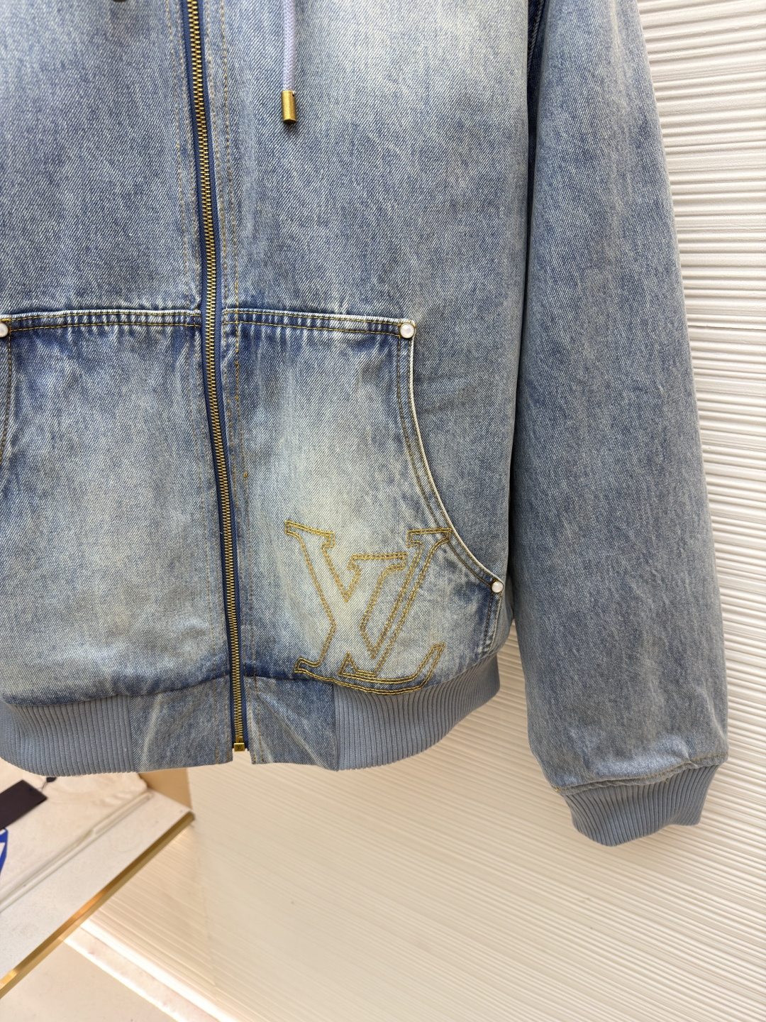 P360 LOUIS VUITTON 口袋字母刺绣连帽牛仔外套
●原版：21579购入开发
●货号：1682616-C25
●面料：牛仔面料
●工艺：刺绣制作
●颜色：洗水蓝
●版型：合身版型
●克重：约1390克
●尺码：46-48-50-52
●描述：这件LOUIS VUITTON连帽抽绳拉链徽标刺绣工装长袖牛仔外套，选用重磅复古水洗牛仔布打造，经过多道酵洗与石磨工艺，呈现自然柔和的浅蓝褪色效果与细腻做旧纹理。外套采用宽松落肩版型，搭配罗纹收边袖口与下摆，兼顾复古工装感与日常穿着舒适度。连帽设计配备同色系抽绳，金属拉链头镌刻品牌标识，前幅立体贴袋处饰有低调的LV刺绣徽标，袋口以金属铆钉加固，兼具装饰性与耐用性。内里采用格纹棉质面料提升穿着体验，每一处缝线都经过精细处理，既保留了牛仔的硬朗质感，又融入了LV标志性的精致细节，是打造随性街头造型的高阶选择。整体走线平直细腻，面料舒适柔软，颜色一致无色差 能与同款搭配营造时尚造型，驾驭各种场合，定制辅料，三标齐全，男女同款！