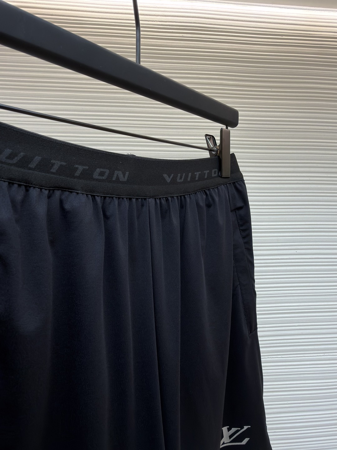 P205 LOUIS VUITTON 双层松紧腰拉链侧袋徽标运动短裤
●原版：9350购入开发
●货号：1682617-A75
●面料：速干面料
●工艺：定位裁床制作
●颜色：黑色
●版型：合身版型
●克重：约285克
●尺码：S-M-L-XL
●描述：这款LV男士短裤采用高密锦纶速干面料，兼具挺括质感与透气性能，面料经抗皱、抗静电处理，日常穿着不易起球变形。腰头采用双层弹力织带设计，织带表面采用立体压印工艺呈现品牌标识，既强化品牌辨识度，又保证了穿着的贴合度与舒适度。裤身采用双线包边工艺，侧缝隐藏式口袋运用激光切割与高温热压技术封边，边缘平整无毛边。裤脚采用撞色包边设计，与腰头形成视觉呼应，裤腿外侧的LV标识采用硅胶立体烫印工艺，触感饱满且不易脱落，整体工艺兼具实用性与品牌标志性，满足日常休闲与轻运动场景需求。整体走线平直细腻，面料舒适柔软，颜色一致无色差 能与同款搭配营造时尚造型，驾驭各种场合，定制辅料，三标齐全，男女同款！