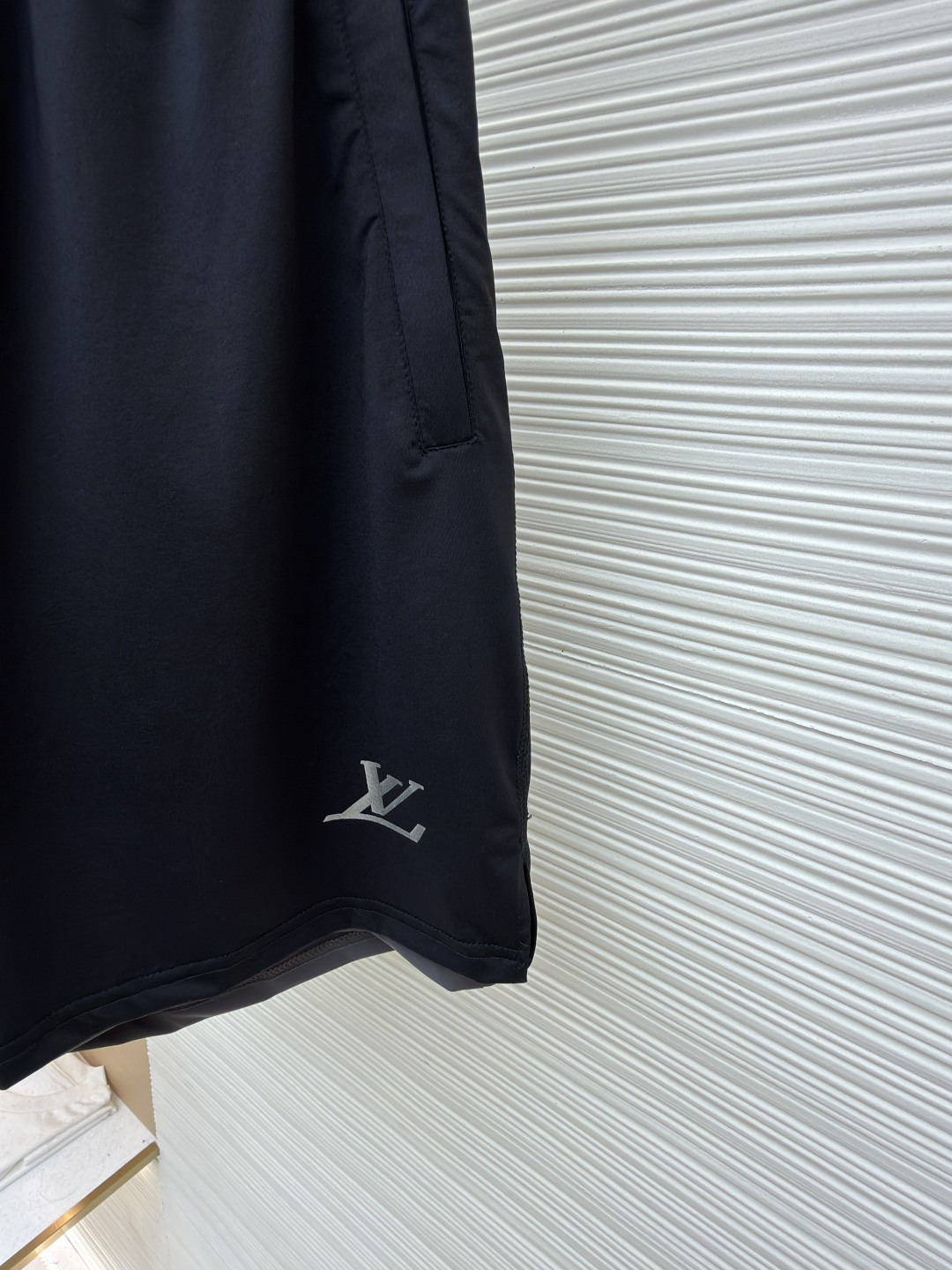 P205 LOUIS VUITTON 双层松紧腰拉链侧袋徽标运动短裤
●原版：9350购入开发
●货号：1682617-A75
●面料：速干面料
●工艺：定位裁床制作
●颜色：黑色
●版型：合身版型
●克重：约285克
●尺码：S-M-L-XL
●描述：这款LV男士短裤采用高密锦纶速干面料，兼具挺括质感与透气性能，面料经抗皱、抗静电处理，日常穿着不易起球变形。腰头采用双层弹力织带设计，织带表面采用立体压印工艺呈现品牌标识，既强化品牌辨识度，又保证了穿着的贴合度与舒适度。裤身采用双线包边工艺，侧缝隐藏式口袋运用激光切割与高温热压技术封边，边缘平整无毛边。裤脚采用撞色包边设计，与腰头形成视觉呼应，裤腿外侧的LV标识采用硅胶立体烫印工艺，触感饱满且不易脱落，整体工艺兼具实用性与品牌标志性，满足日常休闲与轻运动场景需求。整体走线平直细腻，面料舒适柔软，颜色一致无色差 能与同款搭配营造时尚造型，驾驭各种场合，定制辅料，三标齐全，男女同款！