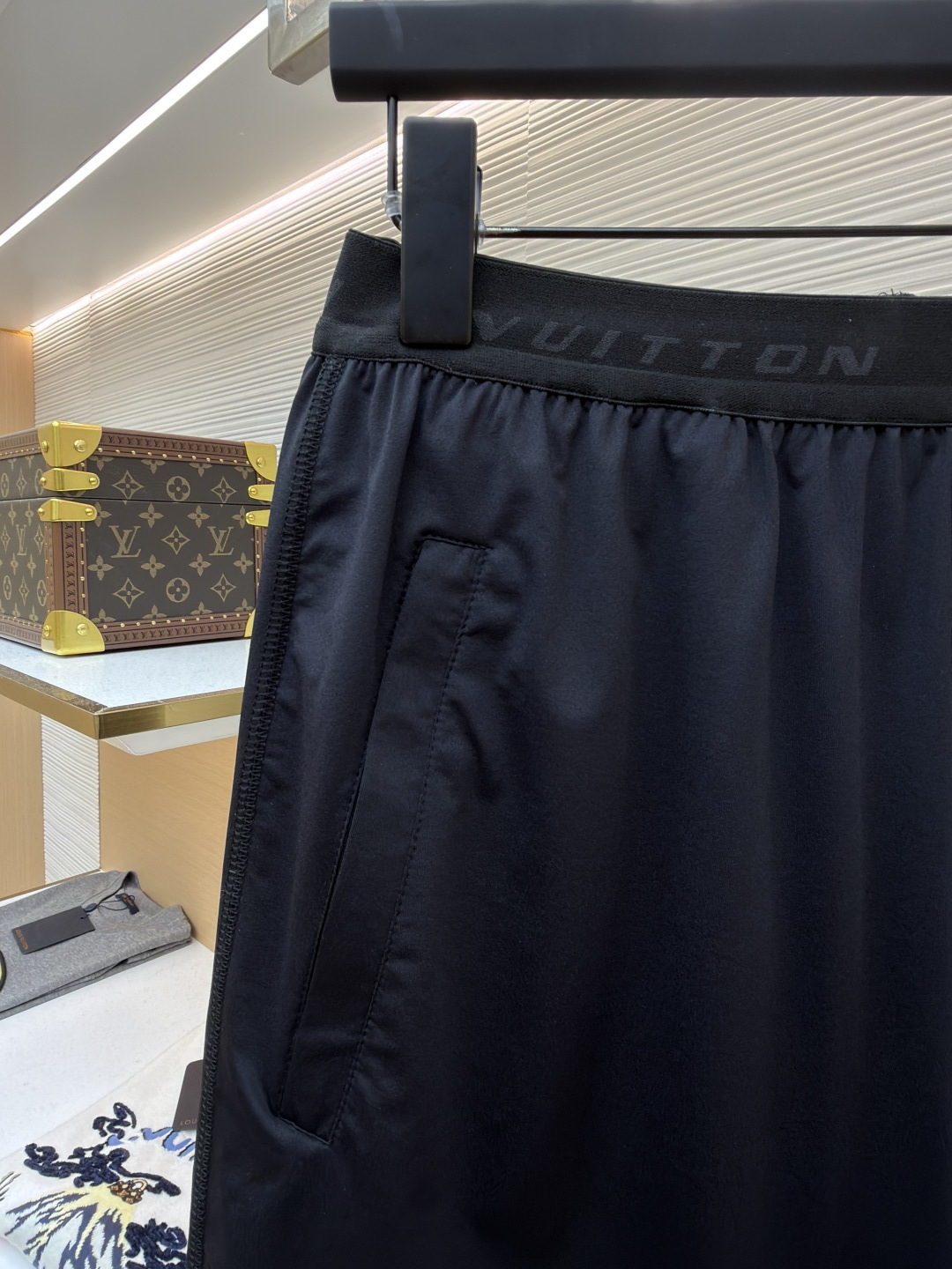 P205 LOUIS VUITTON 双层松紧腰拉链侧袋徽标运动短裤
●原版：9350购入开发
●货号：1682617-A75
●面料：速干面料
●工艺：定位裁床制作
●颜色：黑色
●版型：合身版型
●克重：约285克
●尺码：S-M-L-XL
●描述：这款LV男士短裤采用高密锦纶速干面料，兼具挺括质感与透气性能，面料经抗皱、抗静电处理，日常穿着不易起球变形。腰头采用双层弹力织带设计，织带表面采用立体压印工艺呈现品牌标识，既强化品牌辨识度，又保证了穿着的贴合度与舒适度。裤身采用双线包边工艺，侧缝隐藏式口袋运用激光切割与高温热压技术封边，边缘平整无毛边。裤脚采用撞色包边设计，与腰头形成视觉呼应，裤腿外侧的LV标识采用硅胶立体烫印工艺，触感饱满且不易脱落，整体工艺兼具实用性与品牌标志性，满足日常休闲与轻运动场景需求。整体走线平直细腻，面料舒适柔软，颜色一致无色差 能与同款搭配营造时尚造型，驾驭各种场合，定制辅料，三标齐全，男女同款！