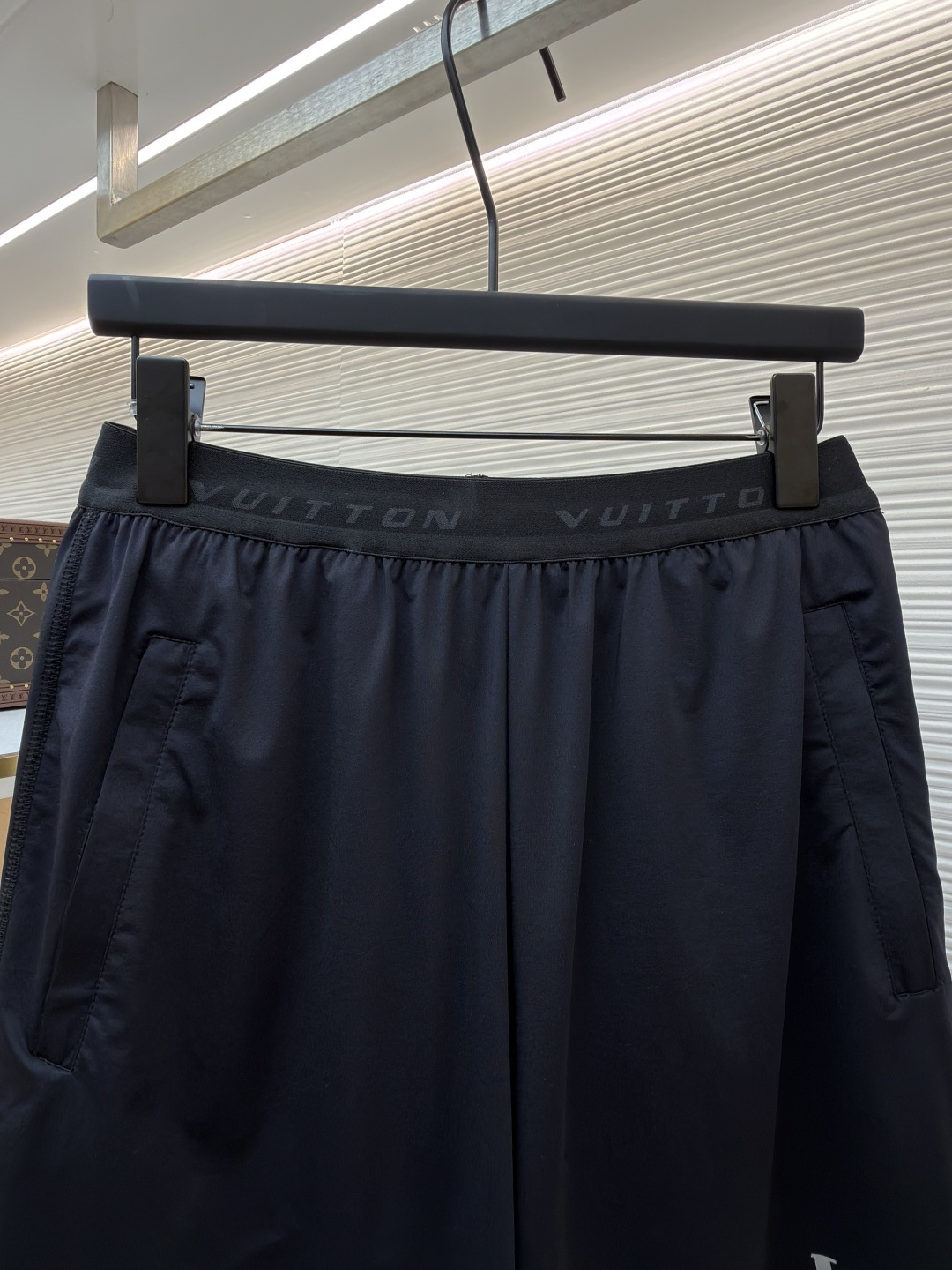 P205 LOUIS VUITTON 双层松紧腰拉链侧袋徽标运动短裤
●原版：9350购入开发
●货号：1682617-A75
●面料：速干面料
●工艺：定位裁床制作
●颜色：黑色
●版型：合身版型
●克重：约285克
●尺码：S-M-L-XL
●描述：这款LV男士短裤采用高密锦纶速干面料，兼具挺括质感与透气性能，面料经抗皱、抗静电处理，日常穿着不易起球变形。腰头采用双层弹力织带设计，织带表面采用立体压印工艺呈现品牌标识，既强化品牌辨识度，又保证了穿着的贴合度与舒适度。裤身采用双线包边工艺，侧缝隐藏式口袋运用激光切割与高温热压技术封边，边缘平整无毛边。裤脚采用撞色包边设计，与腰头形成视觉呼应，裤腿外侧的LV标识采用硅胶立体烫印工艺，触感饱满且不易脱落，整体工艺兼具实用性与品牌标志性，满足日常休闲与轻运动场景需求。整体走线平直细腻，面料舒适柔软，颜色一致无色差 能与同款搭配营造时尚造型，驾驭各种场合，定制辅料，三标齐全，男女同款！