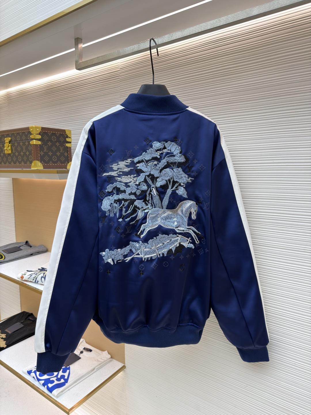 P325 LOUIS VUITTON 马年限定撞色饰带刺绣单排扣长袖夹克
●原版：27975购入开发
●货号：1682618-B90
●面料：全棉面料
●工艺：刺绣制作
●颜色：蓝白
●版型：合身版型
●克重：约1165克
●尺码：46-48-50-52
●描述：这款LV马年限定撞色饰带刺绣夹克，采用重磅哑光缎面面料，兼具挺括垂坠感与柔滑触感，表面经抗皱防泼水处理，日常打理便捷。立领与袖口、下摆采用高弹罗纹针织，紧密贴合且不易松弛变形，门襟选用定制哑光金属单排扣，扣面刻有品牌标识，兼具质感与辨识度。肩部与袖身的撞色饰带采用斜纹拼接工艺，边缘经包边处理避免脱线，左胸的品牌标识采用立体刺绣工艺，以多股线迹呈现饱满纹理，内里采用透气衬里，所有缝线处均做包边与锁边处理，整体工艺将传统棒球服版型与马年专属设计元素结合，兼具典藏价值与实穿性。整体走线平直细腻，面料舒适柔软，颜色一致无色差 能与同款搭配营造时尚造型，驾驭各种场合，定制辅料，三标齐全，男女同款！