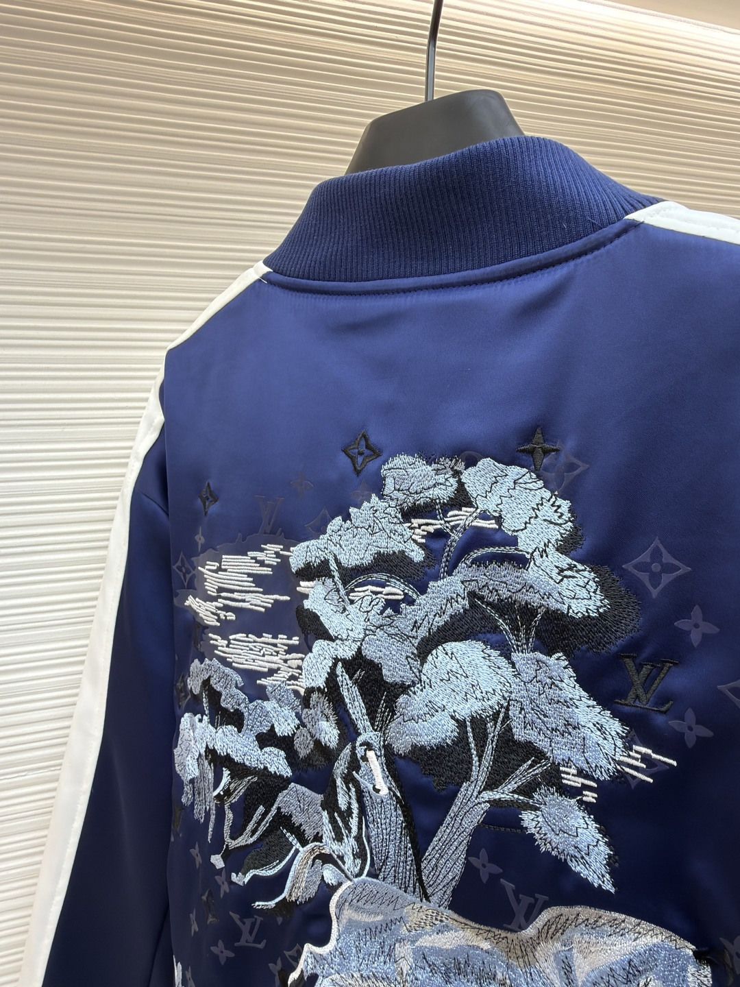 P325 LOUIS VUITTON 马年限定撞色饰带刺绣单排扣长袖夹克
●原版：27975购入开发
●货号：1682618-B90
●面料：全棉面料
●工艺：刺绣制作
●颜色：蓝白
●版型：合身版型
●克重：约1165克
●尺码：46-48-50-52
●描述：这款LV马年限定撞色饰带刺绣夹克，采用重磅哑光缎面面料，兼具挺括垂坠感与柔滑触感，表面经抗皱防泼水处理，日常打理便捷。立领与袖口、下摆采用高弹罗纹针织，紧密贴合且不易松弛变形，门襟选用定制哑光金属单排扣，扣面刻有品牌标识，兼具质感与辨识度。肩部与袖身的撞色饰带采用斜纹拼接工艺，边缘经包边处理避免脱线，左胸的品牌标识采用立体刺绣工艺，以多股线迹呈现饱满纹理，内里采用透气衬里，所有缝线处均做包边与锁边处理，整体工艺将传统棒球服版型与马年专属设计元素结合，兼具典藏价值与实穿性。整体走线平直细腻，面料舒适柔软，颜色一致无色差 能与同款搭配营造时尚造型，驾驭各种场合，定制辅料，三标齐全，男女同款！