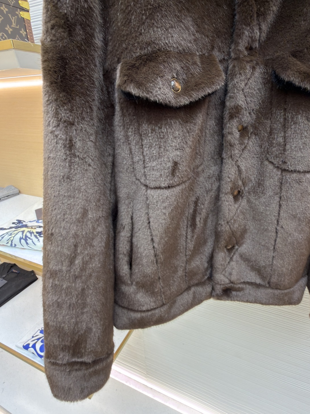 P455 LOUIS VUITTON 纯色长袖尖领皮草
●原版：171000购入开发
●货号：1682619-D15
●面料：水貂毛面料
●工艺：定位裁床制作
●颜色：棕色
●版型：合身版型
●克重：约1220克
●尺码：46-48-50-52
●描述：这款LV棕色仿水貂毛翻领夹克，采用高密仿水貂毛绒面料，绒毛浓密且富有光泽，触感柔软亲肤，兼具保暖性与高级质感。翻领设计沿用经典工装版型，领面与衣身采用同料一体剪裁，边缘经锁边处理防止脱线。门襟选用复古铜色金属按扣，扣面光滑且耐用，两侧翻盖口袋采用隐形缝线工艺，袋口的金属扣与门襟扣呼应，增强整体协调感。左胸的品牌标识牌采用真皮压印工艺，与毛绒面料形成材质对比，袖口与下摆的弹力包边紧密贴合身形，内里采用亲肤衬里避免静电，所有接缝处均做双针加固，兼顾保暖性与工装风格的硬朗质感，是冬季兼具造型感与实用性的单品。整体走线平直细腻，面料舒适柔软，颜色一致无色差 能与同款搭配营造时尚造型，驾驭各种场合，定制辅料，三标齐全，男女同款！