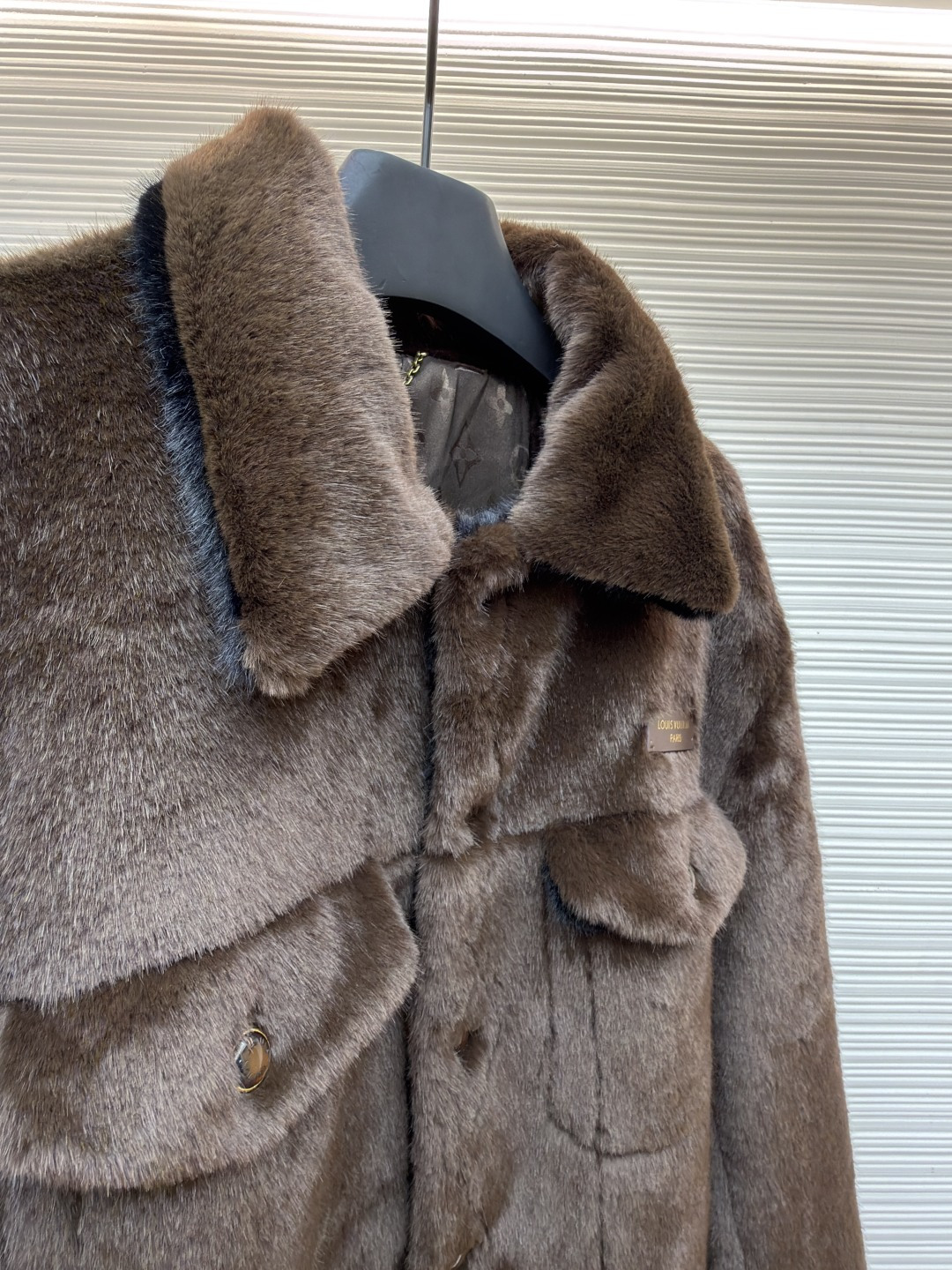 P455 LOUIS VUITTON 纯色长袖尖领皮草
●原版：171000购入开发
●货号：1682619-D15
●面料：水貂毛面料
●工艺：定位裁床制作
●颜色：棕色
●版型：合身版型
●克重：约1220克
●尺码：46-48-50-52
●描述：这款LV棕色仿水貂毛翻领夹克，采用高密仿水貂毛绒面料，绒毛浓密且富有光泽，触感柔软亲肤，兼具保暖性与高级质感。翻领设计沿用经典工装版型，领面与衣身采用同料一体剪裁，边缘经锁边处理防止脱线。门襟选用复古铜色金属按扣，扣面光滑且耐用，两侧翻盖口袋采用隐形缝线工艺，袋口的金属扣与门襟扣呼应，增强整体协调感。左胸的品牌标识牌采用真皮压印工艺，与毛绒面料形成材质对比，袖口与下摆的弹力包边紧密贴合身形，内里采用亲肤衬里避免静电，所有接缝处均做双针加固，兼顾保暖性与工装风格的硬朗质感，是冬季兼具造型感与实用性的单品。整体走线平直细腻，面料舒适柔软，颜色一致无色差 能与同款搭配营造时尚造型，驾驭各种场合，定制辅料，三标齐全，男女同款！