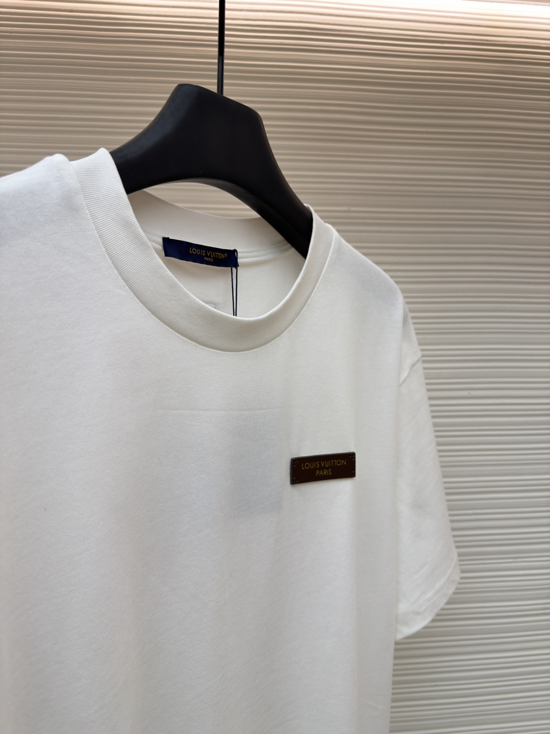 P125 LOUIS VUITTON 皮标标识短袖
●货号：1682622-A00
●面料：全棉面料
●工艺：手工缝标制作
●颜色：白色
●版型：合身版型
●克重：约255克
●尺码：S-M-L-XL
●描述：这款LV白色短袖T恤采用高支双股精梳棉面料，经预缩水处理，触感柔软亲肤且久洗不易变形，圆领采用双层罗纹针织工艺，弹力适中贴合颈部，边缘经加固锁边处理防止松弛卷边。左胸的品牌标识牌选用头层牛皮材质，表面压印品牌标识，通过高温热压工艺与衣身牢固贴合，兼具辨识度与高级质感。衣身采用平缝工艺拼接，缝线细密平整，袖口与下摆采用同料包边处理，避免磨损脱线，整体版型为宽松落肩设计，兼顾舒适体感与简约调性，所有细节均遵循品牌严苛工艺标准，是兼具实穿性与品牌辨识度的日常单品。整体走线平直细腻，面料舒适柔软，颜色一致无色差 能与同款搭配营造时尚造型，驾驭各种场合，定制辅料，三标齐全，男女同款！