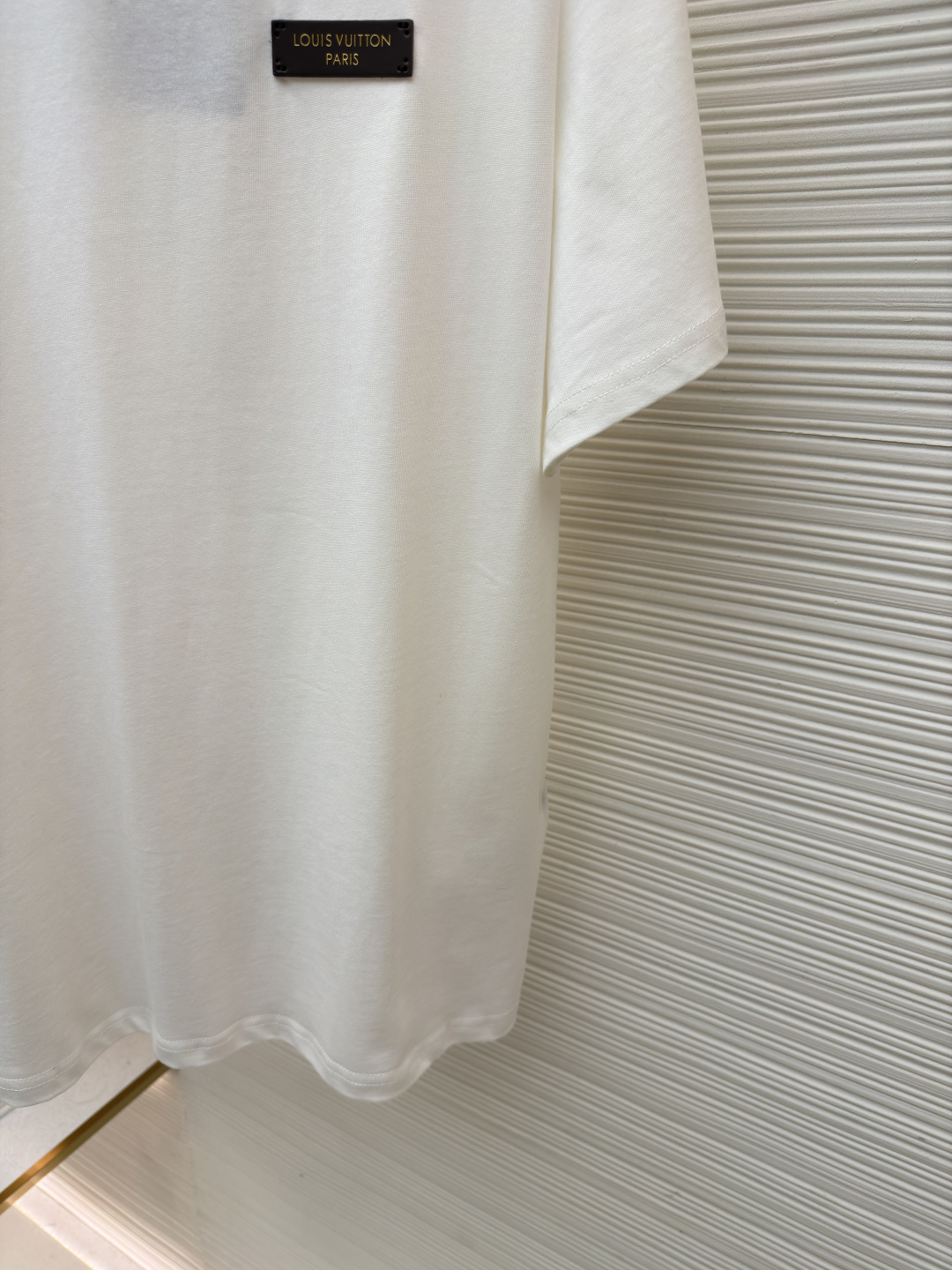 P125 LOUIS VUITTON 皮标标识短袖
●货号：1682622-A00
●面料：全棉面料
●工艺：手工缝标制作
●颜色：白色
●版型：合身版型
●克重：约255克
●尺码：S-M-L-XL
●描述：这款LV白色短袖T恤采用高支双股精梳棉面料，经预缩水处理，触感柔软亲肤且久洗不易变形，圆领采用双层罗纹针织工艺，弹力适中贴合颈部，边缘经加固锁边处理防止松弛卷边。左胸的品牌标识牌选用头层牛皮材质，表面压印品牌标识，通过高温热压工艺与衣身牢固贴合，兼具辨识度与高级质感。衣身采用平缝工艺拼接，缝线细密平整，袖口与下摆采用同料包边处理，避免磨损脱线，整体版型为宽松落肩设计，兼顾舒适体感与简约调性，所有细节均遵循品牌严苛工艺标准，是兼具实穿性与品牌辨识度的日常单品。整体走线平直细腻，面料舒适柔软，颜色一致无色差 能与同款搭配营造时尚造型，驾驭各种场合，定制辅料，三标齐全，男女同款！