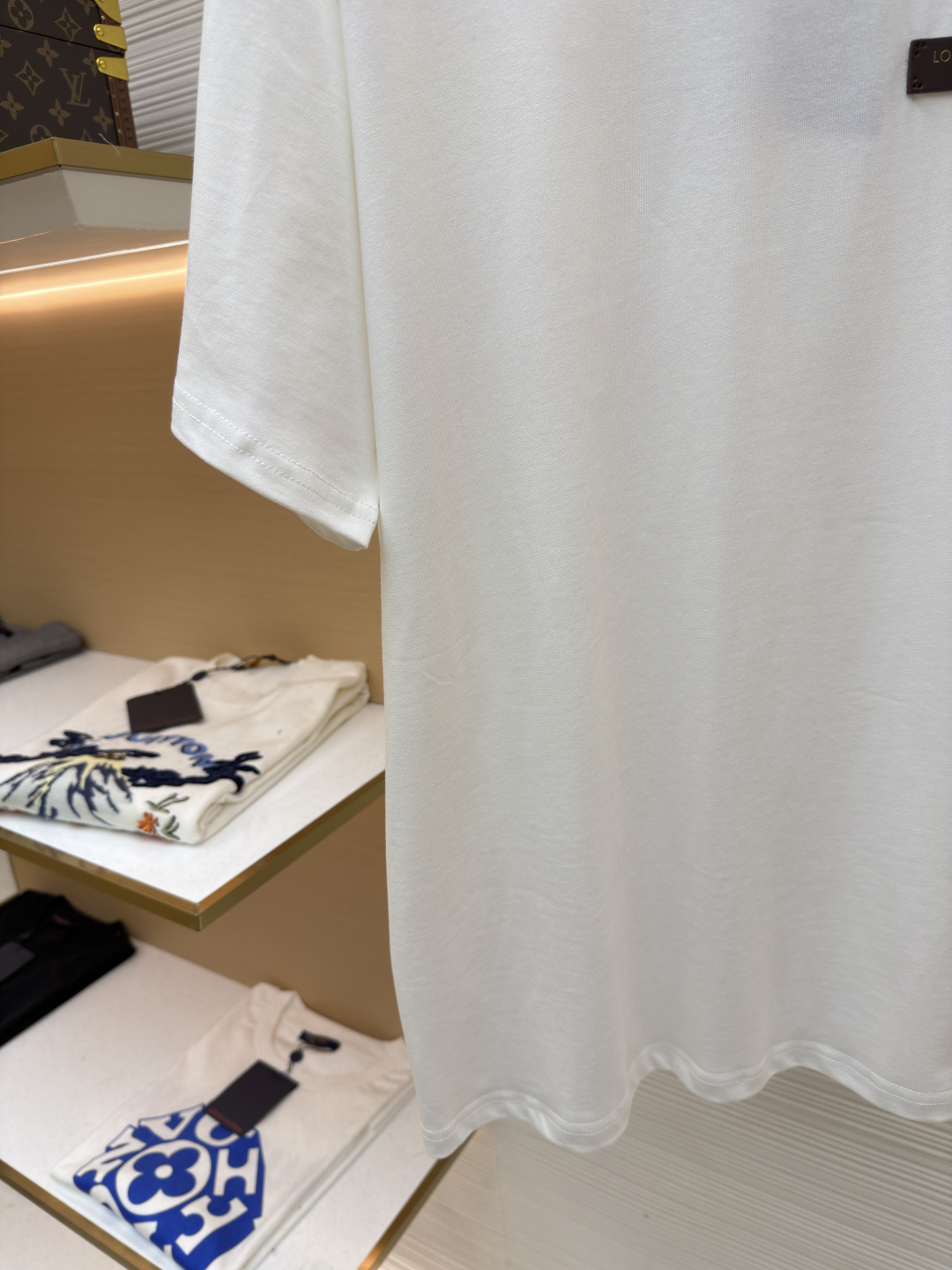 P125 LOUIS VUITTON 皮标标识短袖
●货号：1682622-A00
●面料：全棉面料
●工艺：手工缝标制作
●颜色：白色
●版型：合身版型
●克重：约255克
●尺码：S-M-L-XL
●描述：这款LV白色短袖T恤采用高支双股精梳棉面料，经预缩水处理，触感柔软亲肤且久洗不易变形，圆领采用双层罗纹针织工艺，弹力适中贴合颈部，边缘经加固锁边处理防止松弛卷边。左胸的品牌标识牌选用头层牛皮材质，表面压印品牌标识，通过高温热压工艺与衣身牢固贴合，兼具辨识度与高级质感。衣身采用平缝工艺拼接，缝线细密平整，袖口与下摆采用同料包边处理，避免磨损脱线，整体版型为宽松落肩设计，兼顾舒适体感与简约调性，所有细节均遵循品牌严苛工艺标准，是兼具实穿性与品牌辨识度的日常单品。整体走线平直细腻，面料舒适柔软，颜色一致无色差 能与同款搭配营造时尚造型，驾驭各种场合，定制辅料，三标齐全，男女同款！