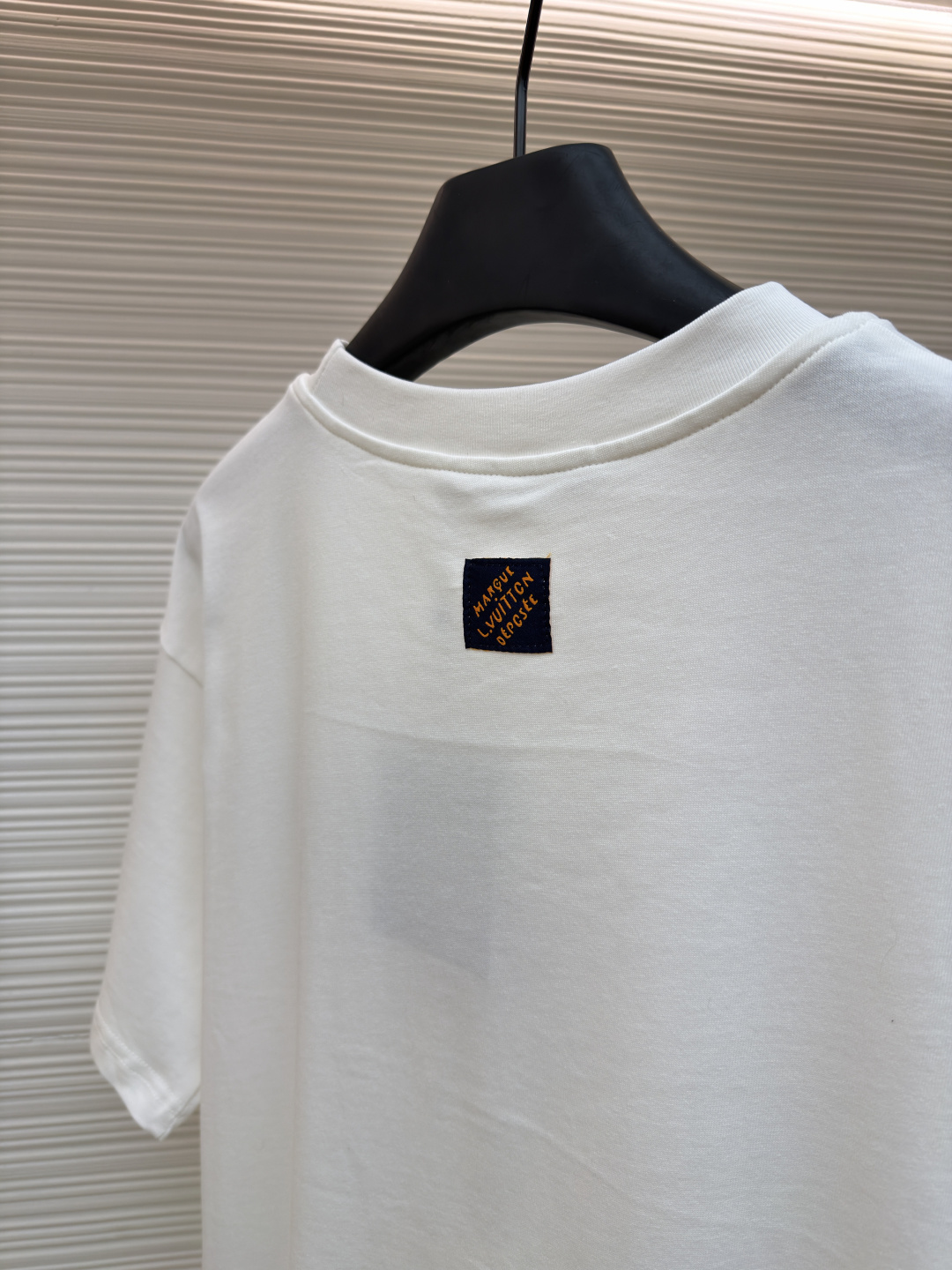 P125 LOUIS VUITTON 皮标标识短袖
●货号：1682622-A00
●面料：全棉面料
●工艺：手工缝标制作
●颜色：白色
●版型：合身版型
●克重：约255克
●尺码：S-M-L-XL
●描述：这款LV白色短袖T恤采用高支双股精梳棉面料，经预缩水处理，触感柔软亲肤且久洗不易变形，圆领采用双层罗纹针织工艺，弹力适中贴合颈部，边缘经加固锁边处理防止松弛卷边。左胸的品牌标识牌选用头层牛皮材质，表面压印品牌标识，通过高温热压工艺与衣身牢固贴合，兼具辨识度与高级质感。衣身采用平缝工艺拼接，缝线细密平整，袖口与下摆采用同料包边处理，避免磨损脱线，整体版型为宽松落肩设计，兼顾舒适体感与简约调性，所有细节均遵循品牌严苛工艺标准，是兼具实穿性与品牌辨识度的日常单品。整体走线平直细腻，面料舒适柔软，颜色一致无色差 能与同款搭配营造时尚造型，驾驭各种场合，定制辅料，三标齐全，男女同款！