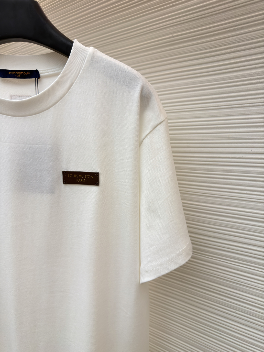 P125 LOUIS VUITTON 皮标标识短袖
●货号：1682622-A00
●面料：全棉面料
●工艺：手工缝标制作
●颜色：白色
●版型：合身版型
●克重：约255克
●尺码：S-M-L-XL
●描述：这款LV白色短袖T恤采用高支双股精梳棉面料，经预缩水处理，触感柔软亲肤且久洗不易变形，圆领采用双层罗纹针织工艺，弹力适中贴合颈部，边缘经加固锁边处理防止松弛卷边。左胸的品牌标识牌选用头层牛皮材质，表面压印品牌标识，通过高温热压工艺与衣身牢固贴合，兼具辨识度与高级质感。衣身采用平缝工艺拼接，缝线细密平整，袖口与下摆采用同料包边处理，避免磨损脱线，整体版型为宽松落肩设计，兼顾舒适体感与简约调性，所有细节均遵循品牌严苛工艺标准，是兼具实穿性与品牌辨识度的日常单品。整体走线平直细腻，面料舒适柔软，颜色一致无色差 能与同款搭配营造时尚造型，驾驭各种场合，定制辅料，三标齐全，男女同款！