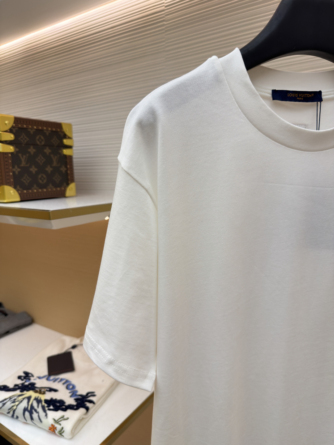 P125 LOUIS VUITTON 皮标标识短袖
●货号：1682622-A00
●面料：全棉面料
●工艺：手工缝标制作
●颜色：白色
●版型：合身版型
●克重：约255克
●尺码：S-M-L-XL
●描述：这款LV白色短袖T恤采用高支双股精梳棉面料，经预缩水处理，触感柔软亲肤且久洗不易变形，圆领采用双层罗纹针织工艺，弹力适中贴合颈部，边缘经加固锁边处理防止松弛卷边。左胸的品牌标识牌选用头层牛皮材质，表面压印品牌标识，通过高温热压工艺与衣身牢固贴合，兼具辨识度与高级质感。衣身采用平缝工艺拼接，缝线细密平整，袖口与下摆采用同料包边处理，避免磨损脱线，整体版型为宽松落肩设计，兼顾舒适体感与简约调性，所有细节均遵循品牌严苛工艺标准，是兼具实穿性与品牌辨识度的日常单品。整体走线平直细腻，面料舒适柔软，颜色一致无色差 能与同款搭配营造时尚造型，驾驭各种场合，定制辅料，三标齐全，男女同款！