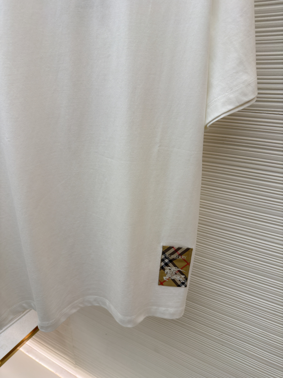 P110 Burberry 经典圆领人字车标格纹标签棉质T恤衫
●原版：3350购入开发
●货号：1682625-X85
●面料：全棉面料
●工艺：人字车标制作
●颜色：白色
●版型：合身版型
●克重：约255克
●尺码：S-M-L-XL
●描述：此款T恤采用高支精梳棉质面料为基底，经过酵素洗水工艺处理，使面料触感更柔软亲肤，同时增强了成衣的抗皱性与穿着舒适度。领口采用双针包边工艺，搭配加固缝线，耐洗不易变形，贴合颈部曲线的同时保证了持久的穿着寿命。衣身侧面的标志性格纹标签采用精密锁边工艺固定，边缘平整牢固；胸前的品牌标识则以人字车线工艺缝制，针脚细密均匀、线条流畅立体，兼具装饰性与辨识度。整体剪裁为宽松版型，车线工整且线头处理干净，结合专业的预缩水处理，有效降低了穿着洗涤后的缩水率，建议手洗以更好地保护面料与精致工艺。整体走线平直细腻，面料舒适柔软，颜色一致无色差 能与同款搭配营造时尚造型，驾驭各种场合，定制辅料，三标齐全，男女同款！