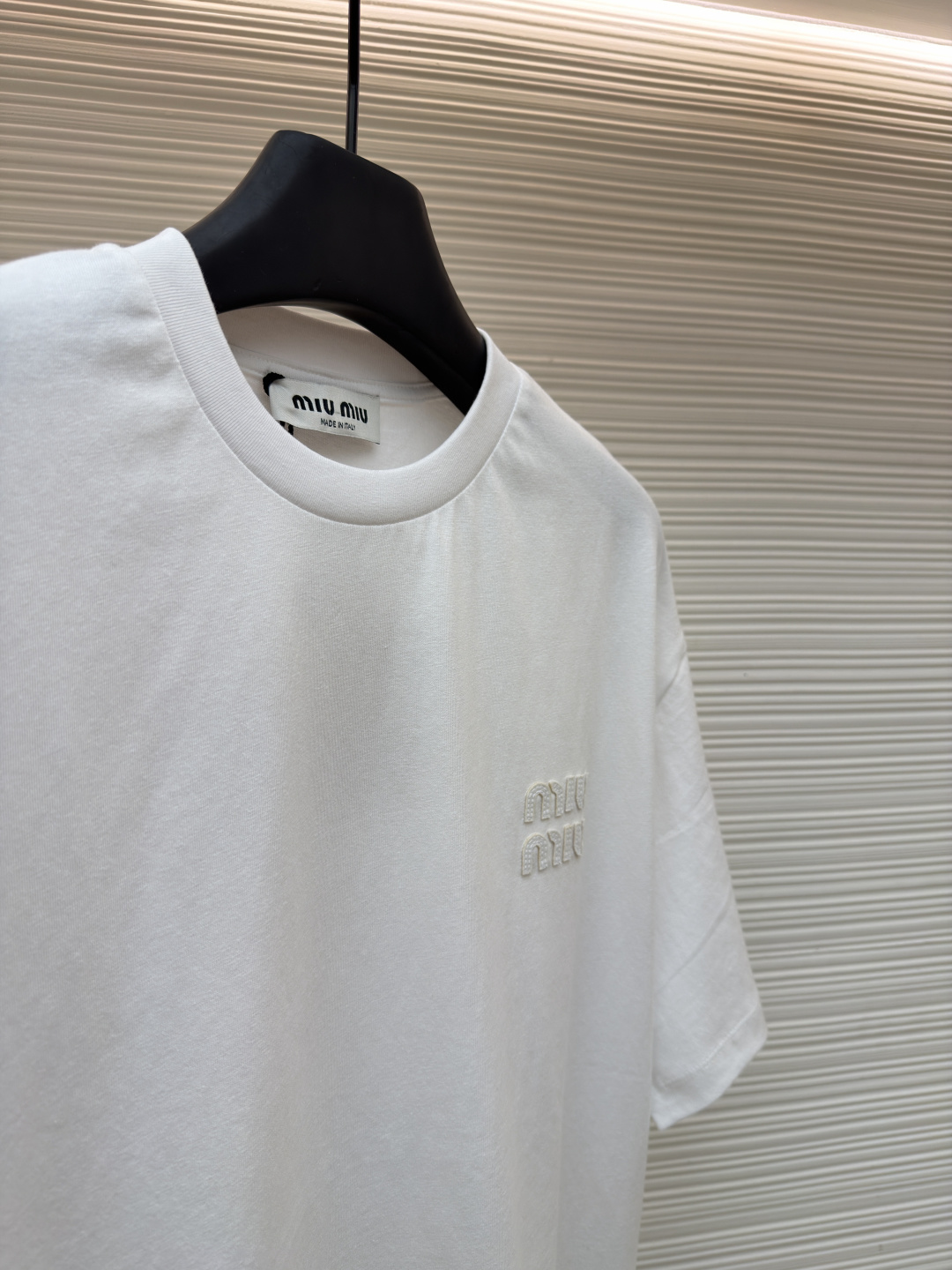 P125 MIU MIU经典字母logo图案短袖
●原版：5350购入开发
●货号：1682626-A00
●面料：精梳棉面料
●工艺：刺绣制作
●颜色：白色
●版型：合身版型
●克重：约220克
●尺码：S-M-L-XL
●描述：这款MIU MIU字母LOGO图案短袖以高支数精梳棉为面料基底，通过酵素洗水工艺处理，使布面触感更柔软顺滑，同时提升了面料的抗皱性与透气性，减少穿着紧绷感。胸前的品牌字母LOGO采用进口刺绣工艺，选用高光泽度的优质绣线，针脚细密均匀、图案立体饱满，兼具细腻质感与品牌辨识度，且经加固处理不易脱线。领口采用双针包边工艺，搭配同色系缝线，耐洗不易变形，贴合颈部曲线的同时保障了穿着舒适度。整体剪裁为宽松落肩版型，车线工整且线头处理干净，结合预缩水处理有效降低了洗涤后的缩水率，建议手洗以更好地保护刺绣细节与面料质感。整体走线平直细腻，面料舒适柔软，颜色一致无色差 能与同款搭配营造时尚造型，驾驭各种场合，定制辅料，三标齐全，男女同款！