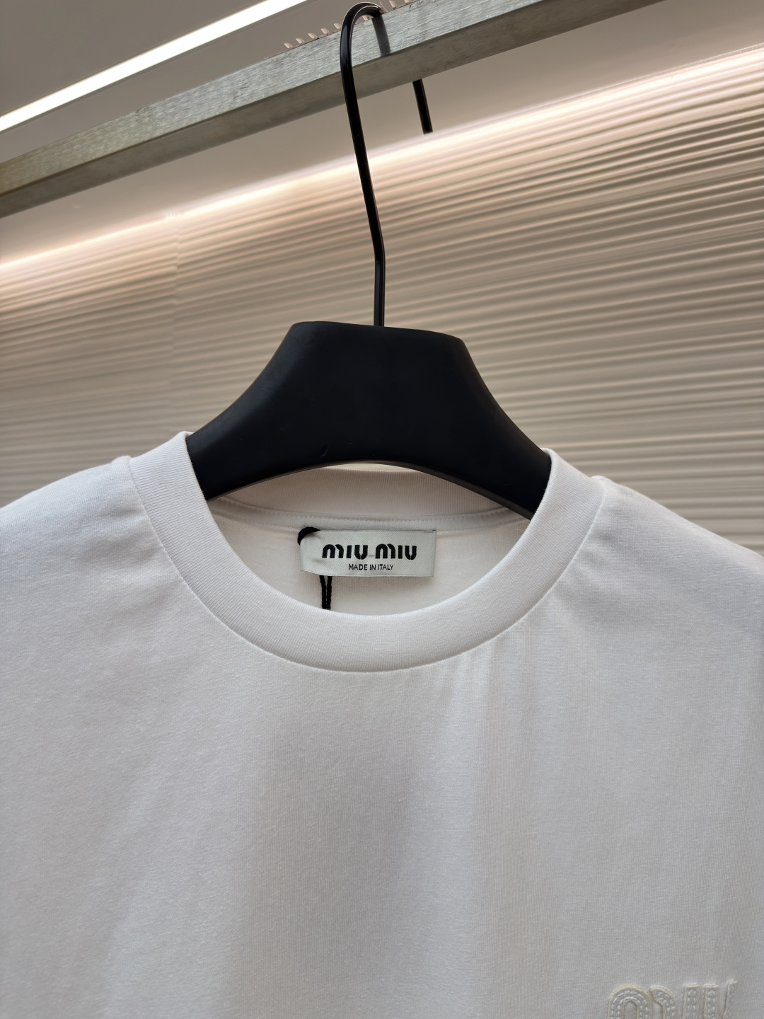 P125 MIU MIU经典字母logo图案短袖
●原版：5350购入开发
●货号：1682626-A00
●面料：精梳棉面料
●工艺：刺绣制作
●颜色：白色
●版型：合身版型
●克重：约220克
●尺码：S-M-L-XL
●描述：这款MIU MIU字母LOGO图案短袖以高支数精梳棉为面料基底，通过酵素洗水工艺处理，使布面触感更柔软顺滑，同时提升了面料的抗皱性与透气性，减少穿着紧绷感。胸前的品牌字母LOGO采用进口刺绣工艺，选用高光泽度的优质绣线，针脚细密均匀、图案立体饱满，兼具细腻质感与品牌辨识度，且经加固处理不易脱线。领口采用双针包边工艺，搭配同色系缝线，耐洗不易变形，贴合颈部曲线的同时保障了穿着舒适度。整体剪裁为宽松落肩版型，车线工整且线头处理干净，结合预缩水处理有效降低了洗涤后的缩水率，建议手洗以更好地保护刺绣细节与面料质感。整体走线平直细腻，面料舒适柔软，颜色一致无色差 能与同款搭配营造时尚造型，驾驭各种场合，定制辅料，三标齐全，男女同款！