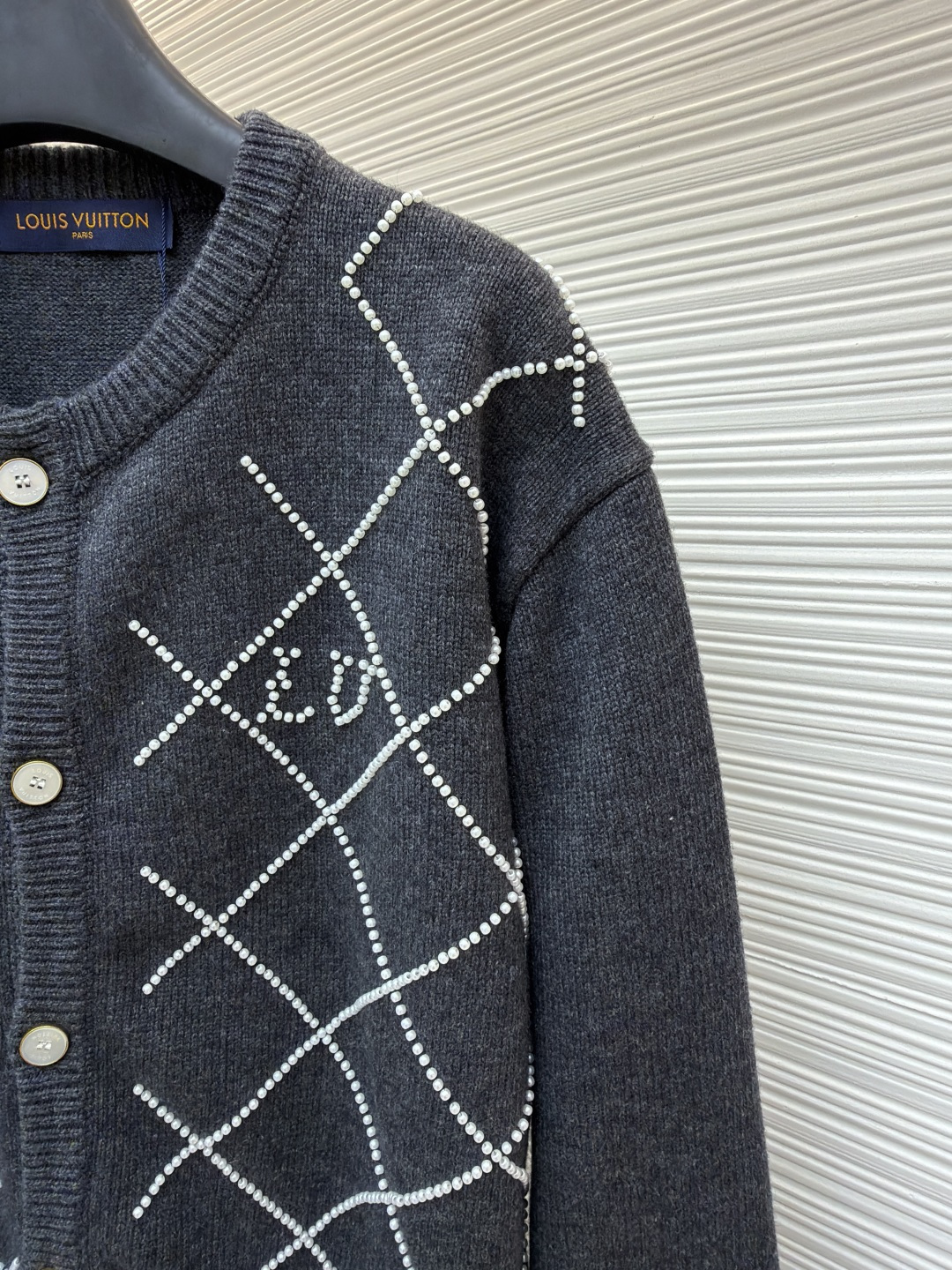 p610 LOUIS VUITTON 字母串珠格纹针织开衫毛衣
●原版：18049购入开发
●面料：羊毛面料
●工艺：针织制作
●颜色：灰色
●版型：合身版型
●克重：约790克
●尺码：S-M-L-XL
●描述：这款圆领开衫采用重磅羊毛混纺面料，深灰色基底质感软糯且保暖性优异，衣身通过手工钉珠工艺打造出立体菱格纹图案，每颗珍珠饰钉经精密定位固定，牢固不易脱落，兼具精致感与辨识度。门襟选用定制天然贝母纽扣，光泽细腻且开合顺滑，圆领及袖口、下摆均采用同色系高弹罗纹收边，经过预缩水处理，久穿不易变形松垮。衣身采用德国斯托尔针织机一体成型工艺，减少拼接缝线，穿着更贴合舒适，同时通过抗起球处理，日常穿着不易起毛起球，整体版型为微宽松剪裁，适配多种身形，是打造秋冬精致通勤造型的质感单品。整体走线平直细腻，面料舒适柔软，颜色一致无色差 能与同款搭配营造时尚造型，驾驭各种场合，定制辅料，三标齐全，男女同款！