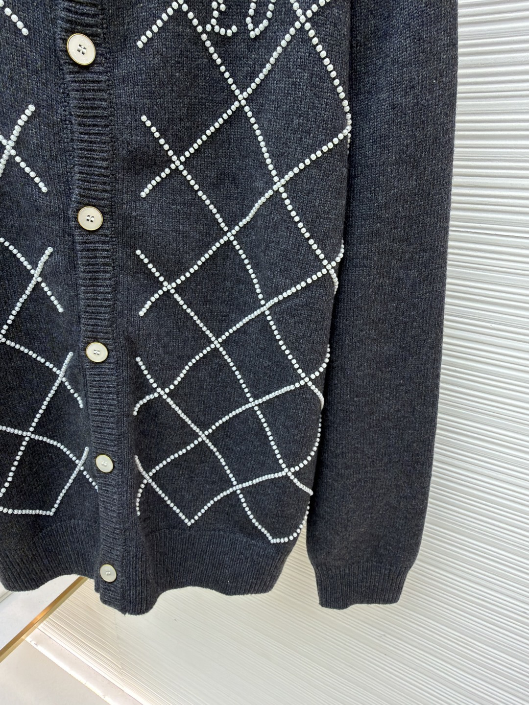 p610 LOUIS VUITTON 字母串珠格纹针织开衫毛衣
●原版：18049购入开发
●面料：羊毛面料
●工艺：针织制作
●颜色：灰色
●版型：合身版型
●克重：约790克
●尺码：S-M-L-XL
●描述：这款圆领开衫采用重磅羊毛混纺面料，深灰色基底质感软糯且保暖性优异，衣身通过手工钉珠工艺打造出立体菱格纹图案，每颗珍珠饰钉经精密定位固定，牢固不易脱落，兼具精致感与辨识度。门襟选用定制天然贝母纽扣，光泽细腻且开合顺滑，圆领及袖口、下摆均采用同色系高弹罗纹收边，经过预缩水处理，久穿不易变形松垮。衣身采用德国斯托尔针织机一体成型工艺，减少拼接缝线，穿着更贴合舒适，同时通过抗起球处理，日常穿着不易起毛起球，整体版型为微宽松剪裁，适配多种身形，是打造秋冬精致通勤造型的质感单品。整体走线平直细腻，面料舒适柔软，颜色一致无色差 能与同款搭配营造时尚造型，驾驭各种场合，定制辅料，三标齐全，男女同款！