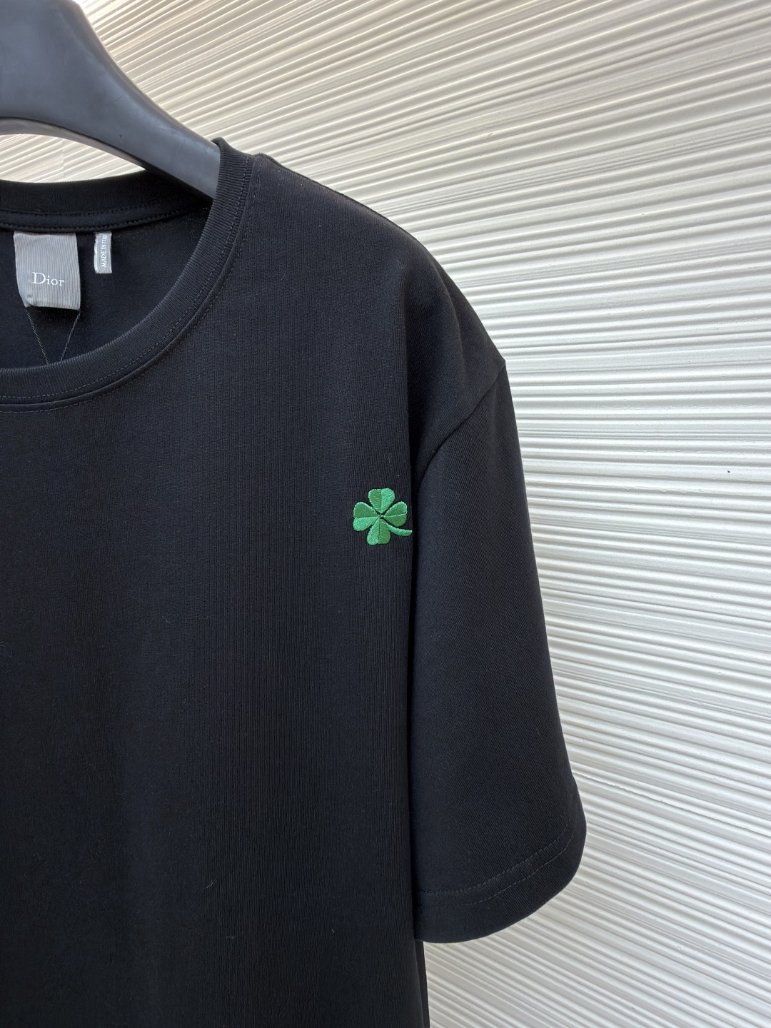 p225 Dior 棉质宽松圆领四叶草刺绣图案T恤
●原版：12000购入开发
●面料：精梳棉面料
●工艺：刺绣制作
●颜色：黑色
●版型：合身版型
●克重：约345克
●尺码：S-M-L-XL
●描述：这款黑色短袖T恤采用高支双股精梳棉混纺面料，经预缩与抗起球处理，触感柔软亲肤，透气吸汗且不易变形起球，色牢度达4级以上，久洗不易褪色发白。领口采用高弹力罗纹搭配三本针包边工艺，反复穿着不易松弛卷边；衣身侧缝采用双针埋夹工艺，走线平整牢固，减少皮肤摩擦感。衣身分布的绿色三叶草图案采用精密刺绣工艺，针脚细密均匀，图案立体饱满且不易脱线；右下角品牌标识采用精细胶印工艺，附着力强不易脱落。成衣经过验针、整烫、去污等多道质检工序，版型宽松有度，适配日常休闲、约会出游等多种场景，兼具精致细节与实穿性。整体走线平直细腻，面料舒适柔软，颜色一致无色差 能与同款搭配营造时尚造型，驾驭各种场合，定制辅料，三标齐全，男女同款！