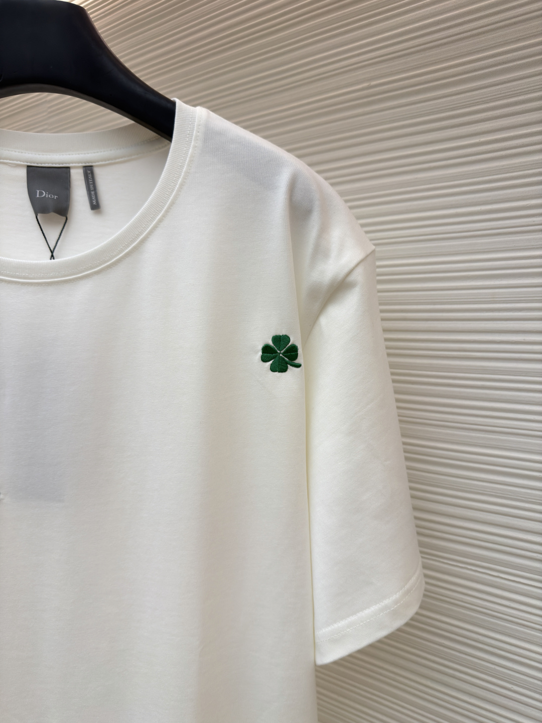 p225 Dior 棉质宽松圆领四叶草刺绣图案T恤
●原版：12000购入开发
●面料：精梳棉面料
●工艺：刺绣制作
●颜色：白色
●版型：合身版型
●克重：约335克
●尺码：S-M-L-XL
●描述：这款黑色短袖T恤采用高支双股精梳棉混纺面料，经预缩与抗起球处理，触感柔软亲肤，透气吸汗且不易变形起球，色牢度达4级以上，久洗不易褪色发白。领口采用高弹力罗纹搭配三本针包边工艺，反复穿着不易松弛卷边；衣身侧缝采用双针埋夹工艺，走线平整牢固，减少皮肤摩擦感。衣身分布的绿色三叶草图案采用精密刺绣工艺，针脚细密均匀，图案立体饱满且不易脱线；右下角品牌标识采用精细胶印工艺，附着力强不易脱落。成衣经过验针、整烫、去污等多道质检工序，版型宽松有度，适配日常休闲、约会出游等多种场景，兼具精致细节与实穿性。整体走线平直细腻，面料舒适柔软，颜色一致无色差 能与同款搭配营造时尚造型，驾驭各种场合，定制辅料，三标齐全，男女同款！