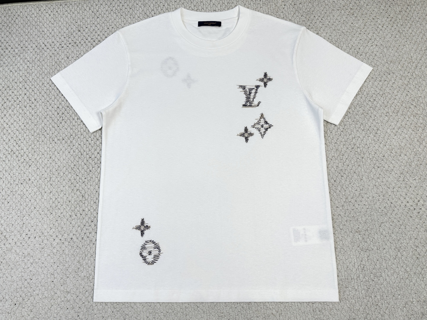 NO:843423,Lv, product introduction 1V / Sashiko embroidered logo T-shirt Fabric 15-count special woven compact cotton plain fabric / 230G Rib 32-count 1×1 rib / 340G This lightweight summer cotton T-shirt has a soft texture and is decorated with the series' iconic Sashiko embroidery. The design is inspired by traditional Japanese craftsmanship, with textured logos embroidered with contrasting yarns. The fine workmanship injects ingenious style into the classic wardrobe. The short sleeves are made of 15-count special-spun compact cotton plain fabric. The special-spun compact spinning process significantly reduces yarn hairiness and has a high pilling resistance level. The medium-high weight gives the fabric excellent bone texture and drape, which is crisp but not stiff. The neckline is made of 32-count spun yarn with ultra-high weight ribbing. It is extremely dense and thick, has high-strength binding force, and can firmly lock the neck arc. The embroidery logos embellished on the front and back adopt Sashiko style craftsmanship, with textured logos embroidered with contrasting yarns. Typical Sashiko embroidery uses thickly twisted cotton thread, and the stitches present a vague undulating texture on the surface of the fabric. Thickly twisted cotton embroidery thread is used in obvious contrast with the background color of the fabric, and the surface of the embroidery thread is slightly hairy. The computer embroidery machine smoothes the curves by shortening the length of the stitches and prevents jagged edges at the turning points. The stitches are arranged in parallel to outline the outline, and the small gaps between the stitches allow the background color of the fabric to faintly show through, forming a unique texture and handmade texture.,,louis vuitton,T-shirt,tees,t-shirt,19860909Lv,产品简介 1V / Sashiko刺绣标识T 恤 面料15支特纺紧密棉平纹面料 / 230G 罗纹32支1×1罗纹 / 340G 本款轻盈夏日棉质T恤质感柔和,饰有本系列标志性Sashiko刺绣.设计灵感源自日本传统工艺,以撞色纱线绣饰纹理感标识.精工之作为经典衣橱注入匠心格调. 短袖选用15支特纺紧密棉平纹面料,特纺紧密纺工艺显著减少了纱线毛羽,同时抗起毛球等级高.中高克重赋予面料极佳的骨感与垂坠性,挺括而不僵硬.领口采用32支细纱配合超高克重罗纹,极其致密厚重,具有高强度收束力,能牢牢锁定颈部弧线. 前后点缀的刺绣标识采用刺子绣风格工艺,以撞色纱线绣饰纹理感标识.典型刺子绣使用粗捻棉线,线迹在面料表面呈现隐约的起伏质感.使用与面料底色形成明显对比的粗捻棉绣线,绣线表面略带毛羽. 电脑绣花机通过缩短针步长度来平滑曲线,防止转折处出现锯齿状.针迹以平行排列的方式勾勒轮廓,针迹间的微小间隙让面料底色隐约透出,形成独特的纹理感与手工质感.,,louis vuitton,T-shirt,tees，t-shirt,,Men's clothing