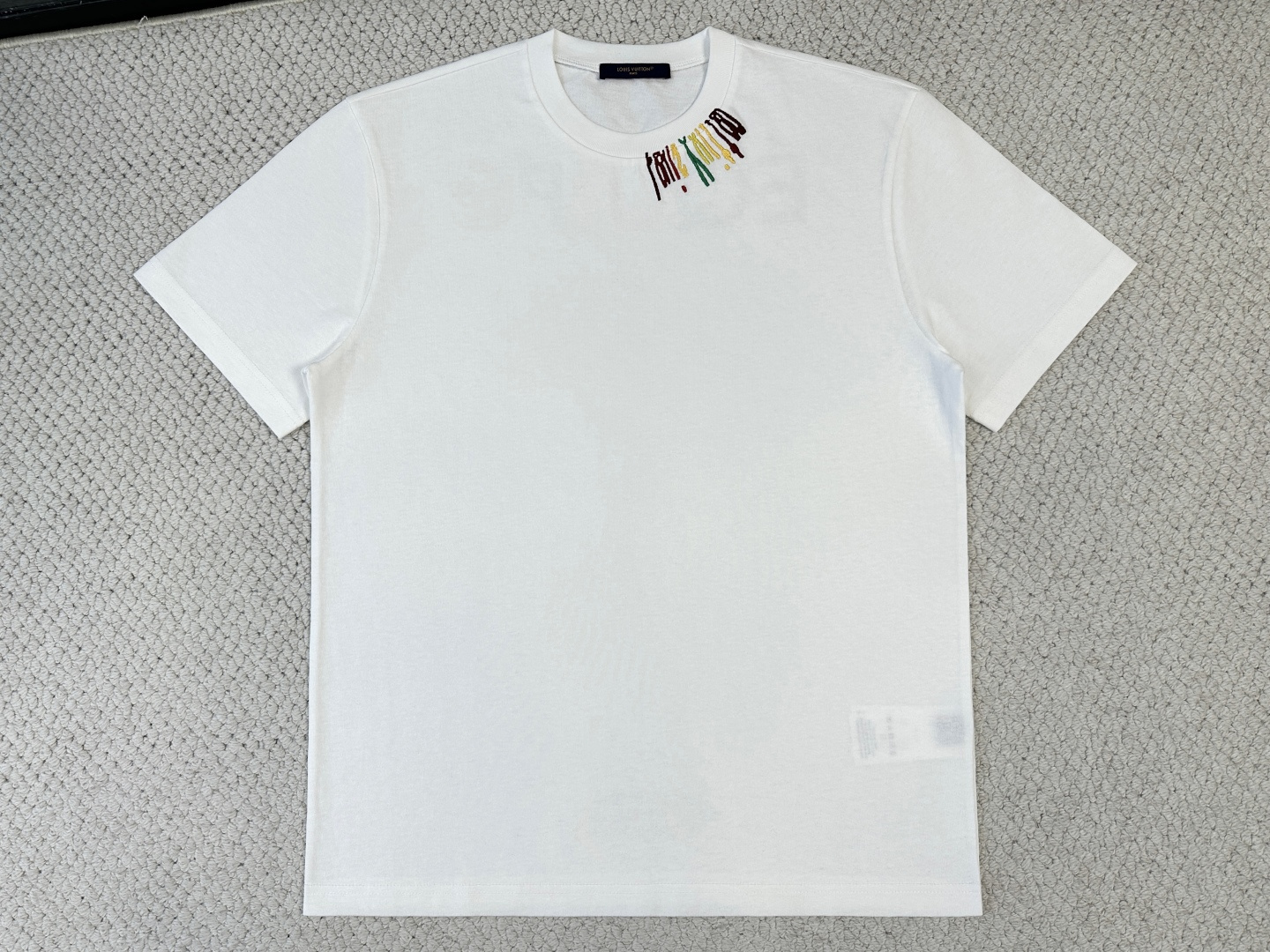 NO:956377,Ｌｖ Product Introduction 1V / Transportation team round neck T-shirt Fabric 15S special woven compact cotton / 230G Rib 32S 1×1 rib / 340G  Compact spinning technology effectively eliminates yarn hairiness, making the yarn body smooth and even, and the fabric presents a slightly matte high-end texture with excellent anti-pilling performance. The 15-count medium and low yarn count gives the fabric a solid fleshy feel and a flexible frame, with both a moderate drape and stiff support, and can naturally fit the body curve while maintaining a clear outline.  Four-color wool and cotton thread are used for needle embroidery. During the embroidery, the needle length is staggered and the needle direction is changed, so that the yarns of different colors form natural color gradients and texture transitions on the surface of the fabric; sharp edges are achieved through the precise narrowing of the cotton thread. The plush feeling of the wool gives the pattern a rich and full three-dimensional layer, and the smoothness of the cotton thread ensures clear details.  Special elastic glue is accurately transferred to the fabric through a high-mesh screen screen. The color logo is produced using a water-based polymer environmentally friendly elastic glue printing process. The printed area can expand and contract synchronously with the fabric without cracking or falling off, and is perfectly suitable for knitted fabrics. The smooth color blocks of the printing echo the three-dimensional texture of the embroidery, presenting a rich texture contrast.,,tees, t-shirt,19860909Ｌｖ 产品简介 1V / 运输团队圆领T恤 面料15S特纺紧密棉 / 230G 罗纹32S 1×1罗纹 / 340G 紧密纺技术有效消除纱线毛羽,使纱体光洁、条干均匀,面料呈现微雾面高级质感,抗起毛球性能优异.15支中低纱支赋予面料扎实肉感与柔韧骨架,兼具适度垂坠感与挺括支撑力,能自然贴合身体曲线同时保持清晰轮廓. 采用四色毛线加棉线插针绣,绣制时通过针脚长短交错、方向多变的插针手法,使不同颜色的纱线在面料表面形成自然的色彩渐变与肌理过渡；边缘处通过棉线的精密收针实现锐利边界.毛线自带的毛绒感赋予图案浑厚饱满的立体层次,棉线的光洁则确保细节清晰. 通过高目数丝网网版,将特制弹力胶浆精准转印至面料,彩色标识采用水性高分子环保弹力胶浆印花工艺制作.印花区域能随面料同步伸缩而不开裂、不脱落,完美适配针织面料.印花的平滑色块与刺绣的立体肌理相互呼应,呈现丰富的质感对比.,,tees，t-shirt,,Men's clothing