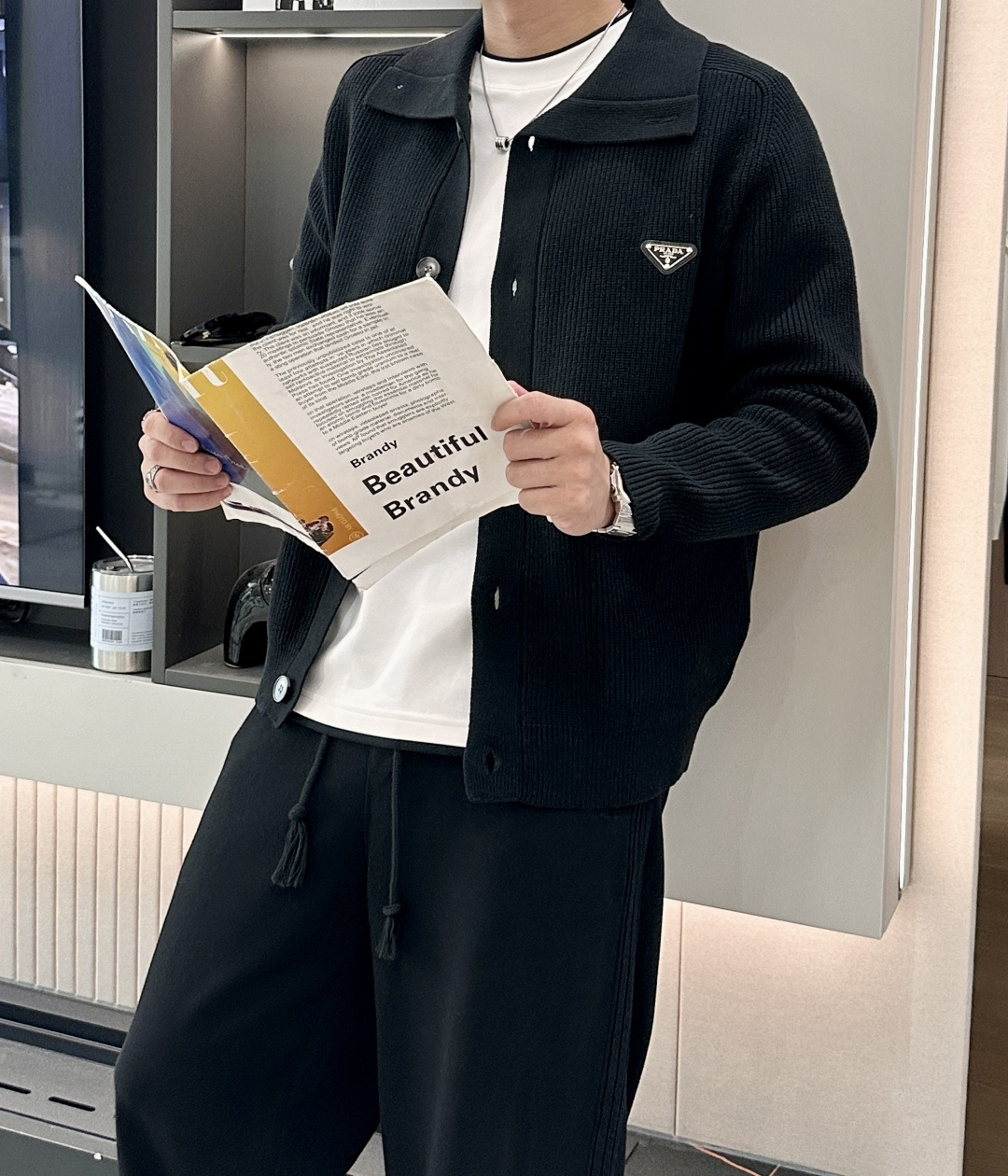 NO:540317,【PRADA Early Autumn Series】Minimalist declaration of triangle logo design narrative from nylon revolution to knitted poems This season's black knitted cardigan takes PRADA's iconic triangular metal logo as the visual core, reinterpreting the 'pragmatic aesthetic' since its founding in 1913. Designer Miuccia Prada extends the brand's classic Re-Nylon recycled nylon technology to the knitting field, creating a modern wardrobe item that combines environmentally friendly concepts and luxurious texture. Craft deconstruction uses 68 ultra-fine merino wool and recycled polyester fiber blending to achieve zero waste production through Swiss Santoni seamless knitting technology. The double-layer lapel design at the neckline is in line with the classic elements of PRADA's 1950s luggage. The front is customized matte black butterfly buttons, which form a material comparison with the metal triangular logo.  Contemporary interpretation of minimalism in styling grammar This cardigan redefines luxury and leisure with the design philosophy of 'less is more'. The straight silhouette and 62cm gold garment length shape a gender-free style that transcends gender. The double patch pocket design combines decorative and practicality. The oblique cutting process enhances the three-dimensional level. The black main tone and metal logo form a low-key luxury, adapted to multiple scenes. Size m-xxxl,,miumiu,prada,gold,alexander wang19860909【PRADA 早秋系列】三角徽标的极简主义宣言 设计叙事从尼龙革命到针织诗篇 本季黑色针织开衫以PRADA标志性的三角金属徽标为视觉核心,重新诠释品牌1913年创立以来的「实用主义美学」.设计师Miuccia Prada将品牌经典的Re-Nylon再生尼龙技术延伸至针织领域,打造兼具环保理念与奢华质感的现代衣橱单品. 工艺解构 采用68支超细美利奴羊毛与再生聚酯纤维混纺,通过瑞士Santoni无缝针织技术实现零浪费生产 领口处的双层翻领设计暗合PRADA 1950年代行李箱包的经典元素 前襟定制哑光黑蝶形纽扣,与金属三角徽标形成材质对比 造型语法极简主义的当代演绎 这款开衫以**「少即是多」**的设计哲学重新定义奢华休闲 直筒廓形与62cm黄金衣长塑造跨越性别的无性别风格 双贴袋设计兼具装饰性与实用性,袋口斜切工艺增强立体层次 黑色主调与金属徽标形成低调奢华感,适配多元场景 尺码m-xxxl,,miumiu,prada,gold,alexander wang,Men's clothing