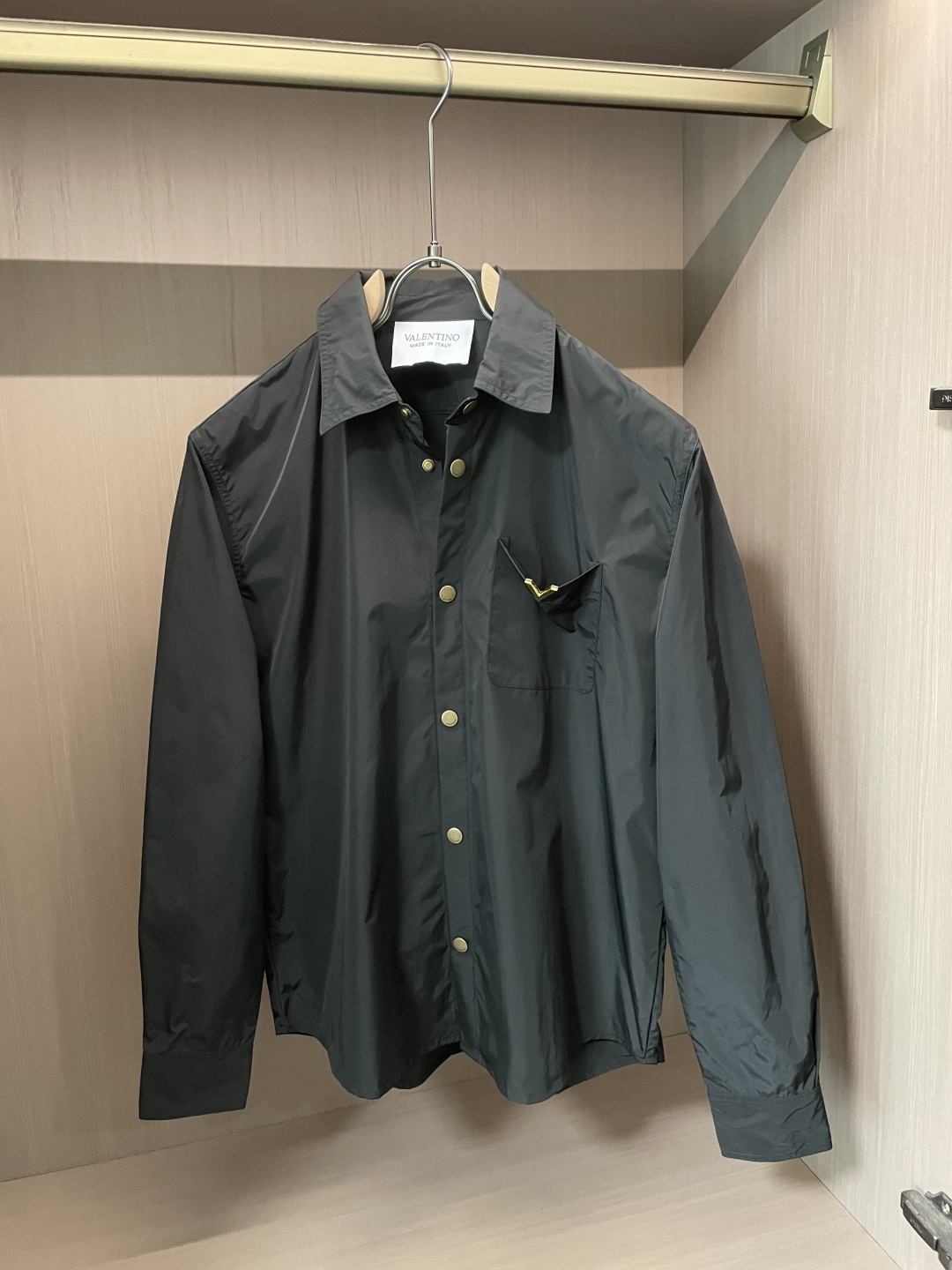 NO:838569,Valentino nylon shirt | low-key luxury brand language. The dark gray matte nylon fabric has a high-end matte texture. The neat tailoring weakens the rigidity of the shirt, but retains the neat aura of formal wear.  The metal V logo on the chest pocket is Valentino's signature ingenuity. The minimalist background hides the genes of the luxury brand that are immediately identifiable. The retro golden breast buttons echo the details, breaking the dark dullness and adding a sense of exquisite ritual to daily wear.  Made in Italy, the workmanship can stand up to fine details from routing to pattern. It can be worn alone to create a relaxed commuting style, or it can be layered with sweatshirts and sweaters, easily adapting to business and leisure scenes. It is a low-key yet high-quality item in the wardrobe. Sizes m-xxl,, valentino, valentino, hoodie, sweatshirts, sweaters, shirts,19860909Valentino 尼龙衬衫｜低调的奢牌语言 深灰调的哑光尼龙面料,自带高级雾面肌理感,利落剪裁弱化了衬衫的刻板,却保留了正装的利落气场. 胸前口袋的金属V标,是华伦天奴的标志性巧思,在极简的底色里藏着一眼可辨的奢牌基因.复古金色排扣呼应细节,打破深色沉闷,也让日常穿搭多了一份精致的仪式感. 意大利制造的做工,从走线到版型都经得起细品.可单穿打造松弛通勤风,也可叠搭卫衣、毛衣做层次,轻松适配商务与休闲场景,是衣柜里低调又能打得分的质感单品. 尺码m-xxl,,valentino,valentino,hoodie,sweatshirts,sweaters,shirts,,Men's clothing