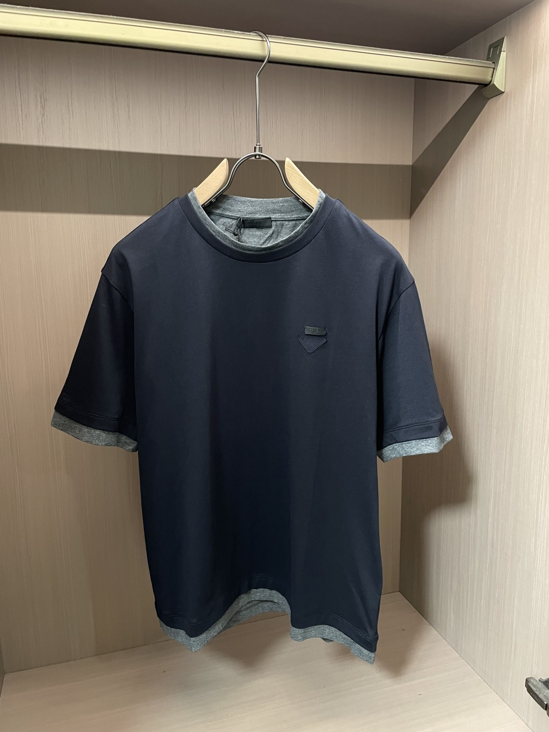 NO:912292,Prad's navy blue fake two-piece round neck short-sleeve, a low-key texture that men just need for commuting. It is made of high-hanging smooth icy fabric, which is smooth and not sweaty on the hand. It has a soft matte texture, which makes the upper body refreshing and breathable in summer, and will not wrinkle and deform easily after long-term wear. The fake two-piece is designed with contrasting gray edges, and the collar, cuffs, and hem have hidden gray layered details. No additional matching is needed, and it can be worn easily to create a sense of hierarchy, and say goodbye to monotonous basic styles.  The triangular logo on the left chest is low-key and has no exaggerated printing. The minimalist, light and luxurious tone is suitable for office commuting, daily leisure, and short-distance travel. The loose and slightly dropped shoulder cut is not tight or bulky, and can accommodate all body shapes. It is neat and stylish when worn alone. It looks calm and high-end when paired with casual trousers and linen trousers. It is a versatile item for mature boys' wardrobes. Sizes s-Xl, prada, T-shirt,19860909Prad 藏青假两件圆领短袖,低调质感男士通勤刚需 甄选高垂顺冰感面料,上手顺滑不闷汗,自带柔和哑光肌理,夏日上身清爽透气,久穿不易起皱变形. 假两件撞灰包边设计,领口、袖口、下摆暗藏灰色叠层细节,不用额外搭配,轻松穿出层次感,告别单调基础款. 左胸三角标低调标识,无浮夸印花,极简轻奢调性适配写字楼通勤、日常休闲、短途出行多种场景. 宽松微落肩剪裁,不紧绷不臃肿,包容各类身形,单穿利落有型,搭配休闲西裤、麻料长裤皆显沉稳高级,成熟男生衣橱百搭单品. 尺码s-Xl,,prada,T-shirt,,Men's clothing