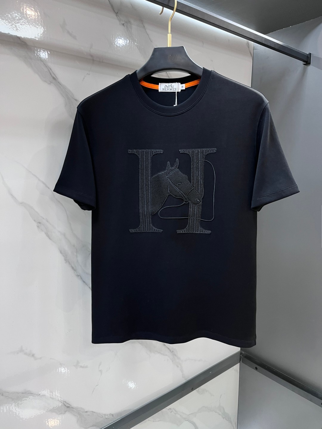 NO:835894,Hermès counter men's short-sleeved T-shirts belong to the brand's iconic equestrian theme series. - The front of the design uses eye-catching horse head embroidery/patches, with orange rein details, echoing the brand's profound equestrian tradition. The fabric is usually made of high-weight cotton, with a crisp texture, skin-friendly and breathable. - Positioned as a light luxury casual item, similar models on the official website are priced in the RMB range. Design highlights -  The equestrian element horse head pattern is the classic symbol of Hermès, originating from the history of harness manufacturing when the brand was founded in 1837. - The embroidery or leather patchwork details are exquisite, and the orange trim strip on the inside of the collar is also a highly recognizable detail of the brand. - The slightly wide tailoring combines comfort and fashion, and is suitable for daily leisure or light business occasions.……………………………………………………………… SizeM-XXXL, hermes, T-shirt, tees, t-shirt,19860909爱马仕 专柜男士短袖T恤,属于品牌标志性的马术主题系列. - 设计正面采用了醒目的马头刺绣/贴饰,搭配橙色缰绳细节,呼应品牌深厚的马术传统. 面料通常为高克重全棉材质,质感挺括,亲肤透气. - 定位轻奢休闲单品,官网类似款售价在人民币元区间.  设计亮点  - 马术元素马头图案是爱马仕的经典符号,源自品牌1837年创立之初的马具制造历史. - 工艺细节刺绣或拼皮工艺精致,领口内侧的橙色饰条也是品牌辨识度很高的细节. - 版型微阔剪裁,兼顾舒适与时尚感,适合日常休闲或轻商务场合.…………………………………………………… SizeM-XXXL,,hermes,T-shirt,tees，t-shirt,,Men's clothing