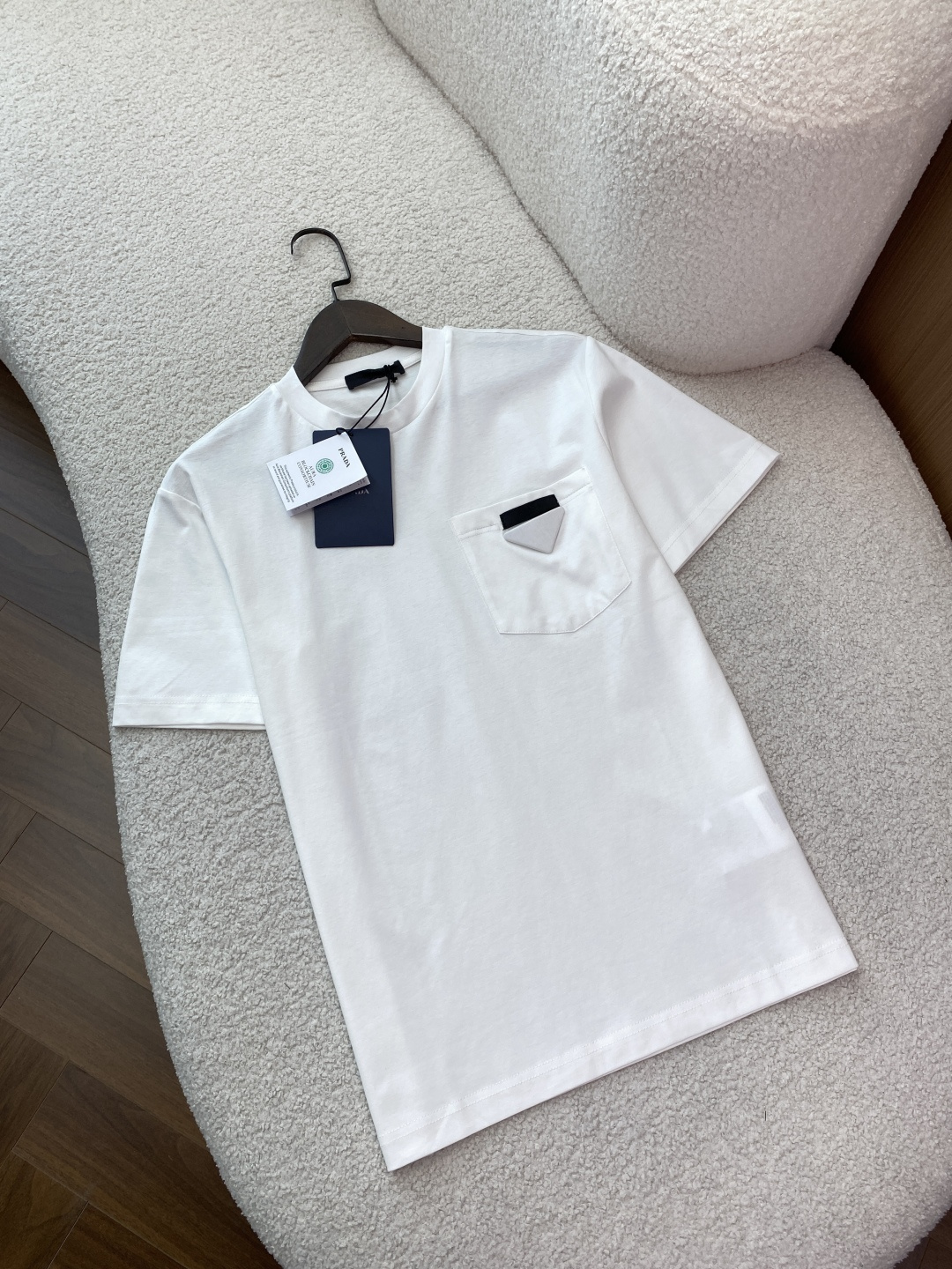 NO:884987,(Liquid ammonia mercerized fabric) Prada triangle pocket short-sleeved T-shirt. The brand logo is sewn with Prada's iconic triangle patch on the left breast pocket. This is a highly recognizable detail of the brand. The design is classic round neck short sleeves, slightly loose/square cut, and straight hem, taking into account both comfort and neatness. Fabric and ingredients Cotton, the fabric is high-count plain cotton, smooth and breathable, and good skin-friendly.  The silhouette has a slightly loose shoulder-drop effect at the back, which is not flattering and can modify the body shape. The pocket triangle mark becomes the visual focus, low-key and recognizable. Wearing scene: daily casual wear with jeans/casual pants + white shoes/sneakers to create a minimalist and high-end feel. Wear a light business suit jacket with this T-shirt inside to balance formality and relaxation. Black and white can be used as a couple's style, with unified style and different details.  Care instructions: Wash inside out with cold water, do not wring out, do not dry clean, cover the cloth surface when ironing to protect the triangle mark and fabric texture.,, prada, prada, jeans, jackets & coats, T-shirt, tees, t-shirt, business suit,19860909（液氨丝光面料） Prada（普拉达） 三角标口袋短袖T恤 品牌标识左胸口袋处缝制有Prada标志性三角标饰片.这是品牌辨识度极高的细节. 版型设计经典圆领短袖,版型偏微宽松/方正剪裁,直裁下摆,兼顾舒适感与利落感. 面料与成分棉,面料为高支平纹棉,触感顺滑透气,亲肤性佳. 版型呈现上身后为微宽松落肩效果,不挑身材,能修饰身形,口袋三角标成为视觉焦点,低调又有辨识度. 穿搭场景 日常休闲搭配牛仔裤/休闲裤+小白鞋/板鞋,打造极简高级感. 轻商务外搭西装外套,内搭这件T恤,平衡正式与松弛感. 情侣穿搭黑白两色可作为情侣款,风格统一又有细节差异. 护理说明需冷水反面清洗、不可拧干、不可干洗,熨烫时需覆盖布面,以保护三角标与面料质感.,,prada,prada,jeans,jackets & coats,T-shirt,tees，t-shirt,business suit,,Women's clothing
