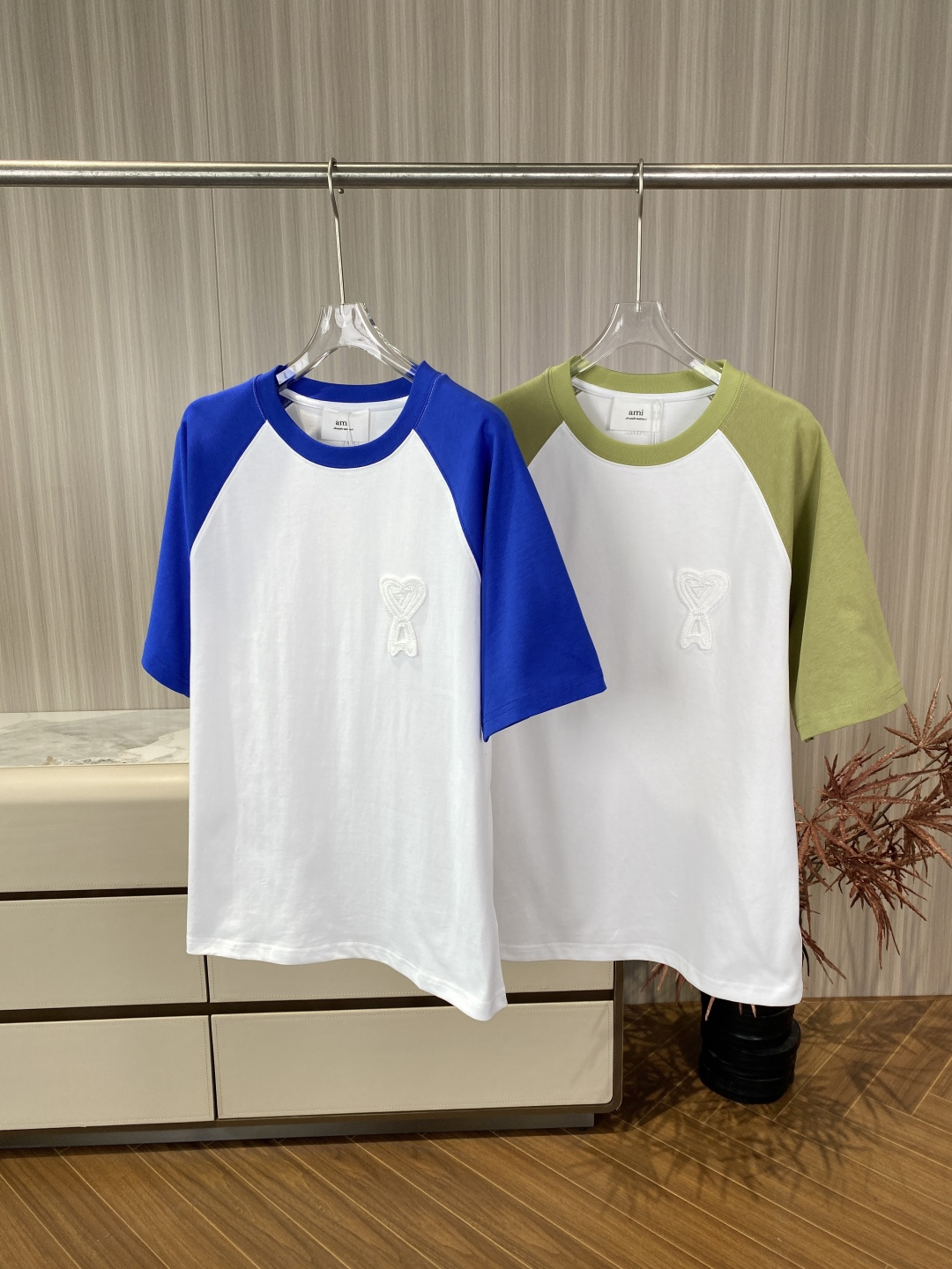 NO:835715,AMI Paris Raglan Sleeve Round Neck Short Sleeve T-shirt Design and Craftsmanship Details 1. The love A embroidery is located on the left chest, using the three-dimensional Terry Stitch process. The edge of the 'A' letter is clear and there is no white miscellaneous thread overflow; the love is full, and the embroidery is tight and flat, with no loose or rough feeling. The embroidered A bottom line is parallel and plump. 2. The raglan sleeve sleeve shape is classic Raglan  Sleeve, the arcs of the armholes are smooth, and the stitching at the connection with the body is neat and there are no excess threads. The blue and white/green and white colors are contrasting and there is no obvious color difference. 3. The ribbed round neckline is moderate in width and has good elasticity. The inside is edged with herringbone webbing, and the collar label is sewn on the webbing. It is fixed manually at only two points (one stitch at the top and bottom) for easy disassembly. 4.  The back collar has the same color 'AMI' letter embroidery on the inside of the neck, which is slightly raised to the touch and is clear and does not fall off. 5. Stitching and accessories Side seams, shoulder seams, cuffs, and hems are all double-lane stitching, with even and straight lines and no skipped stitches. The wash mark is made of satin material, with clear printing. The edges of the font and wash symbol are sharp and not blurred or smudged. The collar mark is black satin, with 'AMI ALEXANDRE' printed on it.  MATTIUSSI', the font is bold and clear, 'alexandre mattiussi' is in italics, and the letters are closely spaced. The version is the same for men and women, with a standard round neck, raglan sleeve design, and a slightly loose fit. Material: Organic Cotton, the fabric is thick and textured, feels stiff rather than soft, and has good breathability. Wear it casually for daily wear alone with jeans or sports shorts to create a casual French style.  Wear layered wear with a long-sleeved bottoming shirt inside and a denim jacket or suit jacket outside to increase the sense of style. As a popular CP style for couples, wearing the same color in different colors is tacit and eye-catching.,,shorts,jeans,jackets & coats,jackets & coats,T-shirt,tees,t-shirt,business suit,19860909AMI Paris 插肩袖圆领短袖T恤 设计与工艺细节 1. 爱心A刺绣位于左胸,采用立体毛巾绣（Terry Stitch）工艺.“A”字母边缘清晰,无白色杂线溢出；爱心饱满,刺绣绣得紧密、平整,无松散或毛糙感.刺绣的A字底边线条平行且丰满. 2. 插肩袖袖型为经典的Raglan Sleeve,袖窿弧线平滑,与衣身连接处缝线工整,无多余线头.蓝白/绿白配色对比鲜明,无明显色差. 3. 领口罗纹圆领,宽度适中,弹性好.内侧为鱼骨纹织带包边,领标缝于织带上,仅用两点手工固定（上下各一针）,方便拆卸. 4. 后领压印颈后内侧有同色“AMI”字样的字母刺绣,触感有轻微凸起,清晰不脱落. 5. 车线与辅料 侧缝、肩缝、袖口、下摆均为双道平车线,走线均匀、平直,无跳针. 洗水标为缎面材质,印刷清晰,字体和洗水符号边缘锐利,无模糊或晕染. 领标为黑色缎面,印有“AMI ALEXANDRE MATTIUSSI”,字体加粗、清晰,“alexandre mattiussi”为斜体,字母间距紧密. 版型男女同款,标准圆领,插肩袖设计,剪裁合身略宽松. 材质 有机棉（Organic Cotton）,面料厚实有质感,触感应是挺括而非软糯,透气性好. 日常休闲单穿搭配牛仔裤或运动短裤,打造随性法式风格. 层次穿搭内搭长袖打底衫,外穿牛仔夹克或西装外套,增加造型感. 情侣穿搭作为热门CP款,同穿不同配色,默契又吸睛.,,shorts,jeans,jackets & coats,jackets & coats,T-shirt,tees，t-shirt,business suit,,Women's clothing