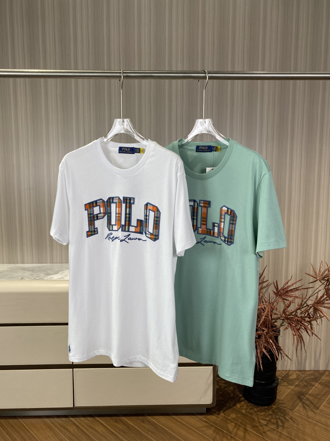 NO:873332,Polo Ralph Lauren plaid POLO letter short-sleeved T-shirt 1. The core vision of the chest logo is the large 'POLO' letter patch, which is made of classic orange and green plaid fabric (echoing the Scottish plaid element), and the edges are edged with thick navy blue lines. The stitching is dense and the three-dimensional effect is highlighted. The handwritten signature of Ralph Lauren is embroidered below the letters. The font is smooth and the stitching is delicate, which is a highly recognizable detail of the brand. The overall layout imitates the American college team jersey, full of retro sports atmosphere.  2. Hem and collar label: There is navy blue Pony embroidery on the left side of the hem, with a standard posture and fine stitching. The neckline is a ribbed round collar, which is highly elastic and not easily deformed. There is a main label with gold characters on a navy blue background sewn on the inside, with the words 'POLO RALPH LAUREN' printed on it. The font is clear and the gold stamping texture is uniform. Next to the main label is a size mark and place of origin, marked 'MADE IN CAMBODIA' (Made in Cambodia).  The hangtag has gold characters on a navy blue background, with 'POLO RALPH LAUREN' printed on the front, and the model number, size, material and other information on the back. The printing is clear and not blurry. The material is made of combed cotton, which is soft and skin-friendly, and has good breathability. It is suitable for spring and summer wear and is not prone to pilling and deformation after washing. The stitching is double-thread overlocked, and the collar, cuffs, and hem are all double-needle stitched, with even stitch spacing and solid workmanship.  The patch lettering adopts patch embroidery + overlocking technology, which has strong edges and is not easy to fall off or warp. Washing advice is to 'wash with clothes of similar colors'. It is recommended to machine wash in cold water, wash inside out, avoid exposure to the sun, and prevent the plaid patch from fading. Color matching: mint green, low saturation and fresh tone, white and soft style, suitable for matching with light-colored bottoms. Pure white classic versatile style, suitable for denim, khaki, black and other types of trousers, suitable for commuting and leisure. Version Regular  Fit (regular fit version), with moderate shoulder line and length that covers the waistline, it can be controlled regardless of body shape, even if you are slightly fat. Pair it with straight jeans and white shoes for daily casual wear, which gives you a full American retro feel. Wear a navy suit jacket outside for commuting, and wear this white T-shirt inside, which is simple and capable. Pair with sports pants and dad shoes to create a dynamic campus style. Couples wear mint green + white styles, the same version but different colors, full of tacit understanding.,, loro  piana,jeans,jackets & coats,T-shirt,tees,t-shirt,business suit,19860909Polo Ralph Lauren 格纹POLO字母短袖T恤 1. 胸前标识 核心视觉为大号“POLO”字母贴布,采用经典橙绿格纹面料（呼应苏格兰格纹元素）,边缘以藏青粗线滚边,针脚密实,立体感突出. 字母下方绣有Ralph Lauren手写体签名,字体流畅且针脚细腻,是品牌辨识度极高的细节. 整体排版模仿美式大学校队球衣,充满复古运动氛围. 2. 下摆与领标 下摆左侧绣有藏青色Pony小马刺绣,姿态标准,针脚细密. 领口为罗纹圆领,弹性好不易变形,内侧缝有藏青底金字主标,印有“POLO RALPH LAUREN”字样,字体清晰且烫金质感均匀. 主标旁附有尺码标与产地标,标注“MADE IN CAMBODIA”（柬埔寨制造）. 吊牌为藏青底金字,正面印有“POLO RALPH LAUREN”,背面标注款号、尺码、材质等信息,印刷清晰无模糊. 材质采用精梳棉,手感柔软亲肤,透气性佳,适合春夏季节穿着,洗后不易起球变形. 工艺 缝线采用双线包缝,领口、袖口、下摆均为双针车线,针距均匀,做工扎实. 贴布字母采用贴布绣+锁边工艺,边缘牢固,不易脱线或起翘. 洗涤建议“与颜色相似的衣物一起清洗”,建议冷水机洗、反面洗涤、避免暴晒,防止格纹贴布褪色. 配色 薄荷绿低饱和清新色调,显白且风格柔和,适合搭配浅色系下装. 纯白色经典百搭款,适配牛仔、卡其、黑色等各类裤装,通勤休闲皆可. 版型Regular Fit（常规合身版）,肩线适中,衣长盖过腰线,不挑身材,微胖体型也能驾驭. 日常休闲搭配直筒牛仔裤+小白鞋,美式复古感拉满. 通勤通勤外搭藏青西装外套,内搭此款白T,简约干练. 运动风搭配束脚运动裤+老爹鞋,打造活力校园风. 情侣穿搭薄荷绿+白色款搭配,同版型不同色,默契感十足.,,loro piana,jeans,jackets & coats,T-shirt,tees，t-shirt,business suit,,Women's clothing