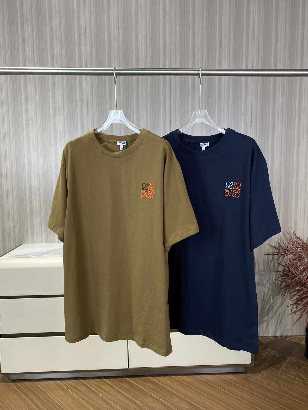 NO:824391,(Original customization) Loewe2026 Colorful Anagram Embroidered T-shirt This is Loewe's 2026 spring and summer core basic T-shirt, with the brand's iconic colorful Anagram (reflective pattern) embroidery as the visual core, focusing on minimalist light luxury and artistic sense. It is a popular must-have item in the light luxury fashion circle. 1. Core design Anagram embroidery technology visual details  The pattern design uses the brand's classic Anagram monogram embroidery on the chest, which is composed of 'L' and 'O'. The color matching (key point) uses contrasting double-thread embroidery technology - the main body is dark coffee/charcoal gray, embellished with bright orange lines. This red-brown color combination not only retains a sense of luxury, but also breaks the dull monochrome, and has a very artistic atmosphere. The embroidery density is ≥45 stitches per square centimeter, which is extremely high and completely opaque to the light.  There are no floating threads or skipped threads on the edges of the stitches, and there is a light interlining on the back of the embroidery, which feels uneven and feels like a full three-dimensional embroidery. Detailed craftsmanship The position is about 15cm from the left chest (standard position), and the visual center of gravity is stable. The textured embroidery thread is made of high-twisted polyester fiber, with soft gloss, no reflection, and no 'cheap shine', which is in line with Loewe's low-key and luxurious tone. Fabric details  The main component is Portuguese combed cotton (clearly marked on the washing label), which belongs to the category of heavyweight cotton. Fabric characteristics After pre-shrunk treatment and anti-pilling treatment, it will not shrink or pill after washing. It is made of double-ply worsted knitting, with a smooth and delicate surface, a matte texture visible to the naked eye, not soft, crisp and stylish. It has excellent breathability, does not stick to the body when sweating in summer, and has a good drape feeling. Loose cut, standard slightly (Relaxed)  Fit), not excessively oversized, with naturally dropped shoulder lines, which can modify slippery or wide shoulders. The neckline is 1x1 ribbed round neck, which is reinforced with three needles. The neckline has excellent elasticity (rebound rate ≥ 95) and will not become loose after long-term wear. The hem/cuffs are flat and hemmed, with no excess thread, and the hem length is just above the waistband and does not block the hips. Daily high-end casual (preferred) Off-white/light khaki straight casual pants (Brunello)  Cucinelli or Uniqlo U). Shoes: brown loafers (Church’s) or white retro running shoes (Asics). Jacket: light gray linen suit or khaki windbreaker. Effect navy top + light bottoms, clean color, red embroidery as the finishing detail, very suitable for dates and afternoon tea. Street fashion style: black ruined jeans (Levi’s 501 retro style). Shoes: black platform shoes (MM6).  Accessories include a silver Cuban necklace and a black baseball cap. The tough black bottoms balance the softness of the T-shirt and are full of street appeal. Minimalist commuting style. Dark gray draped trousers (Theory). Shoes: black minimalist sandals (The Row). The effect is simple and clean, without unnecessary color interference, suitable for work or formal light social occasions.,, brunello cucinelli, loewe, loewe, masion  margiela,versace,loafers,sandals,jeans,jackets & coats,tees,t-shirt,business suit,necklace,hats,19860909（原版定制） Loewe2026 彩色Anagram刺绣T恤 这是罗意威（Loewe）2026春夏核心基础款T恤,以品牌标志性的彩色Anagram（回纹）刺绣为视觉核心,主打极简轻奢与艺术感,是轻奢时尚圈的热门必入单品. 1. 核心设计Anagram刺绣工艺 视觉细节 图案设计胸前采用品牌经典的Anagram交织字母刺绣,由“L”与“O”组成. 色彩搭配（重点）采用撞色双线绣工艺——主体为深咖色/炭灰色,点缀亮橘红色线条.这种红棕配色既保留了高级感,又打破了单色的沉闷,非常有艺术氛围. 刺绣密度 每平方厘米针数≥45针,密度极高,对着光完全不透底布. 针脚边缘无浮线、无跳线,刺绣背面有轻薄衬布,触感凹凸有致,摸起来是饱满的立体绣感. 细节工艺 位置位于左胸15cm处左右（标准位置）,视觉重心平稳. 质感刺绣线采用高捻聚酯纤维,光泽度柔和,不反光、不“廉价发亮”,符合Loewe低调奢华的调性. 面料细节 主体成分葡萄牙精梳棉（洗标明确标注）,属于重磅重磅棉范畴. 面料特性 经过预缩水处理和抗起球处理,洗后不缩水、不起球. 采用双股精纺针织,表面光洁细腻,有肉眼可见的哑光质感,不软塌,挺括有型. 透气性优异,夏季出汗不粘身,具备良好的垂坠感. 版型剪裁 廓形标准微宽松（Relaxed Fit）,非过度Oversize,肩线自然下落,能修饰溜肩或宽肩. 领口1x1罗纹圆领,采用三本针加固工艺,领口弹力极佳（回弹率≥95）,久穿不松垮. 下摆/袖口平整包边,无多余线头,下摆长度刚好过裤腰,不卡胯. 日常高级休闲（首选） 下装米白色/浅卡其色直筒休闲裤（Brunello Cucinelli 或 Uniqlo U）. 鞋子棕色乐福鞋（Church’s）或 白色复古跑鞋（Asics）. 外套浅灰色亚麻西装 或 卡其色风衣. 效果藏青上衣+浅下装,色彩干净,红刺绣作为点睛细节,非常适合约会、下午茶. 街头潮流风 下装黑色破坏牛仔裤（Levi‘s 501 复古款）. 鞋子黑色厚底德训鞋（MM6）. 配饰银色古巴项链、黑色棒球帽. 效果硬朗的黑色下装平衡了T恤的柔美感,街头度拉满. 极简通勤风 下装深灰色垂坠西裤（Theory）. 鞋子黑色极简风凉鞋（The Row）. 效果简约干净,无多余色彩干扰,适合上班或正式轻社交场合.,,brunello cucinelli,loewe,loewe,masion margiela,versace,loafers,sandals,jeans,jackets & coats,tees，t-shirt,business suit,necklace,hats,,Women's clothing