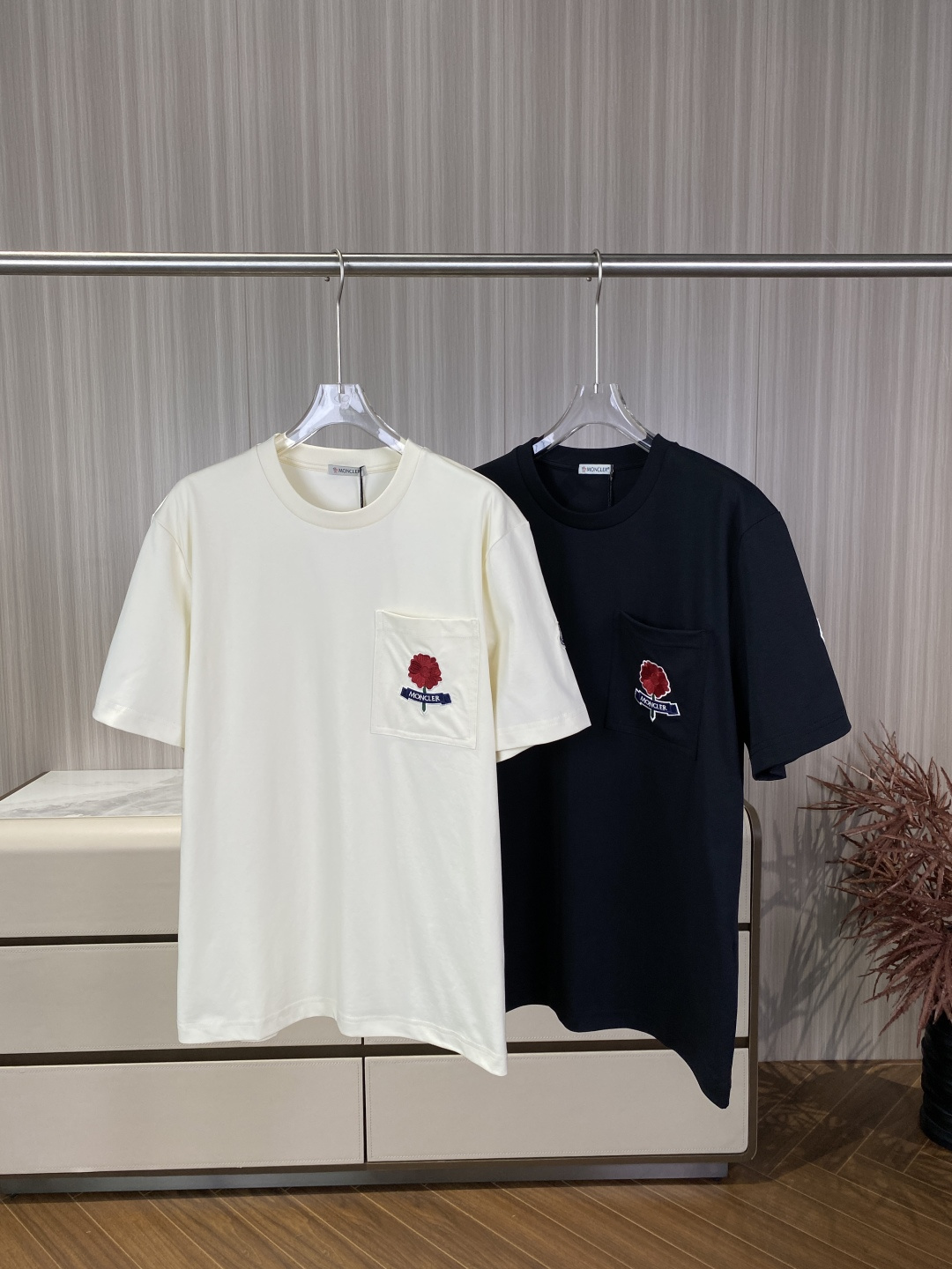 NO:837153,(Original customized model) Moncler Pocket Red Flower Embroidered T-shirt This T-shirt is a special item from Moncler's 2026 spring and summer 'Remembrance' series. It uses poppy flower embroidery as the core vision and combines the brand's outdoor genes and retro romanticism. It is a high-end casual item that is both recognizable and practical. Embroidery technology (soul details) The pattern implies that the red flowers in the chest pocket are poppies, symbolizing commemoration and hope, and is Moncler's design language to pay tribute to history.  Embroidery material: Petal polyester fiber high-twist thread, using layered embroidery technology, the outer layer is bright red, the inner layer is burgundy, forming a gradient three-dimensional effect. The flower stems/leaves are dark green threads, using satin embroidery, the lines are smooth, simulating the real plant shape. The ribbon is navy blue base fabric + white thread embroidery with the word 'MONCLER', and the edges are zigzag seams to prevent thread loss. The stitch standard is ≥40 stitches per square centimeter, the density is extremely high, and the base fabric cannot be seen through when facing the light.  There are no floating lines or skipped lines on the edges of the embroidery, and the petals have clear outlines and no blurring. Pocket structure: Patch pocket design: There is a square patch pocket on the left chest, measuring about 10cm × 10cm. It is sewn with double-needle topstitching. The bag mouth is straight and has no warped edges. The functional pocket can accommodate cards, headphones and other small items, which is both decorative and practical. The stitching process uses flat seams to stitch the pockets and the body, and the stitch spacing is strictly controlled at 2mm, with no exposed threads. Main fabric  Ingredients: Turkish combed cotton (Compact Cotton), a heavyweight plain knitted fabric. Features: Pre-shrunk + anti-pilling treatment, not easy to shrink or pill after washing. The surface is fine and smooth, with a slight matte luster, soft and sinewy to the touch, and has excellent drape. Excellent breathability, suitable for summer wear at 25-35°C, not sweaty. Rib part  The collar/cuff ribs are made of cotton, using a 2×2 rib weave, with an elastic rebound rate of ≥90, making it less likely to loosen and deform after long-term wear. The cut is loose and dropped shoulders (oversize), the shoulder line expands about 2cm, and the length is 3-4cm longer than the regular style, creating a lazy and casual street feel. Details: Double-layer ribbing on the neckline + two-pin seams, the height of the neckline is about 2.5cm, and it fits the neck without being tight.  The cuffs/hem are flat-stitched, with a cuff width of about 6cm, and a slit at the hem of about 3cm, improving freedom of movement. The side seams are overlocked, with no exposed raw edges, making it more comfortable to wear. Core matching principles 1. The color echoes the red color of the safflower embroidery and can echo accessories (such as red socks, red-framed sunglasses) to enhance the overall sense of coordination. 2. Material contrast Cotton T-shirts can be paired with different materials such as denim, linen, and leather to increase visual hierarchy. 3.  It is recommended to wear a loose T-shirt with balanced elasticity and slim fit bottoms (such as straight pants) to avoid being too bloated.,,versace,Moncler,tees,t-shirt,19860909（原版定制款） 蒙口 Moncler 口袋红花刺绣T恤 这款T恤是Moncler 2026春夏「Remembrance」特别系列单品,以罂粟花刺绣为核心视觉,融合了品牌户外基因与复古浪漫主义,是兼具辨识度与实用性的高端休闲单品. 刺绣工艺（灵魂细节） 图案寓意胸前口袋的红色花朵为罂粟花,象征纪念与希望,是Moncler致敬历史的设计语言. 刺绣材质 花瓣聚酯纤维高捻线,采用分层叠绣工艺,外层为亮红色,内层为酒红色,形成渐变立体感. 花茎/叶子深绿色线,采用缎面绣,线条流畅,模拟真实植物形态. 飘带藏蓝色底布+白色线绣「MONCLER」字样,边缘为锯齿形锁边,防止脱线. 针脚标准 每平方厘米针数≥40针,密度极高,对着光看不透底布. 刺绣边缘无浮线、跳线,花瓣轮廓清晰,无模糊晕染. 口袋结构 贴袋设计左胸为方形贴袋,尺寸约10cm×10cm,采用双针明线车缝,袋口平直,无翘边. 功能性口袋可容纳卡片、耳机等小物,兼具装饰与实用性. 拼接工艺口袋与衣身采用平缝拼接,车线间距严格控制在2mm,无外露线头. 主体面料 成分土耳其精梳棉（Compact Cotton）,属于重磅平纹针织. 特性 经过预缩+抗起球处理,洗后不易缩水、起球. 表面细腻光洁,有轻微哑光光泽,触感柔软且有筋骨,垂坠感极佳. 透气性优异,适合25-35℃夏季穿着,不闷汗. 罗纹部分 领口/袖口罗纹为棉,采用2×2罗纹组织,弹力回弹率≥90,长期穿着不易松垮变形. 版型剪裁 版型宽松落肩（Oversize）,肩线外扩约2cm,衣长比常规款长3-4cm,打造慵懒随性的街头感. 细节 领口双层罗纹+二本针锁边,领口高度约2.5cm,贴合颈部不紧绷. 袖口/下摆平车明线收边,袖口宽度约6cm,下摆开衩高度约3cm,提升活动自由度. 侧缝包缝工艺,无外露毛边,穿着更舒适. 搭配核心原则 1. 色彩呼应红花刺绣的红色可与配饰（如红袜、红框墨镜）呼应,提升整体协调感. 2. 材质对比棉质T恤可搭配牛仔、亚麻、皮革等不同材质,增加视觉层次. 3. 松紧平衡宽松T恤建议搭配修身下装（如直筒裤）,避免整体过于臃肿.,,versace,Moncler,tees，t-shirt,,Women's clothing