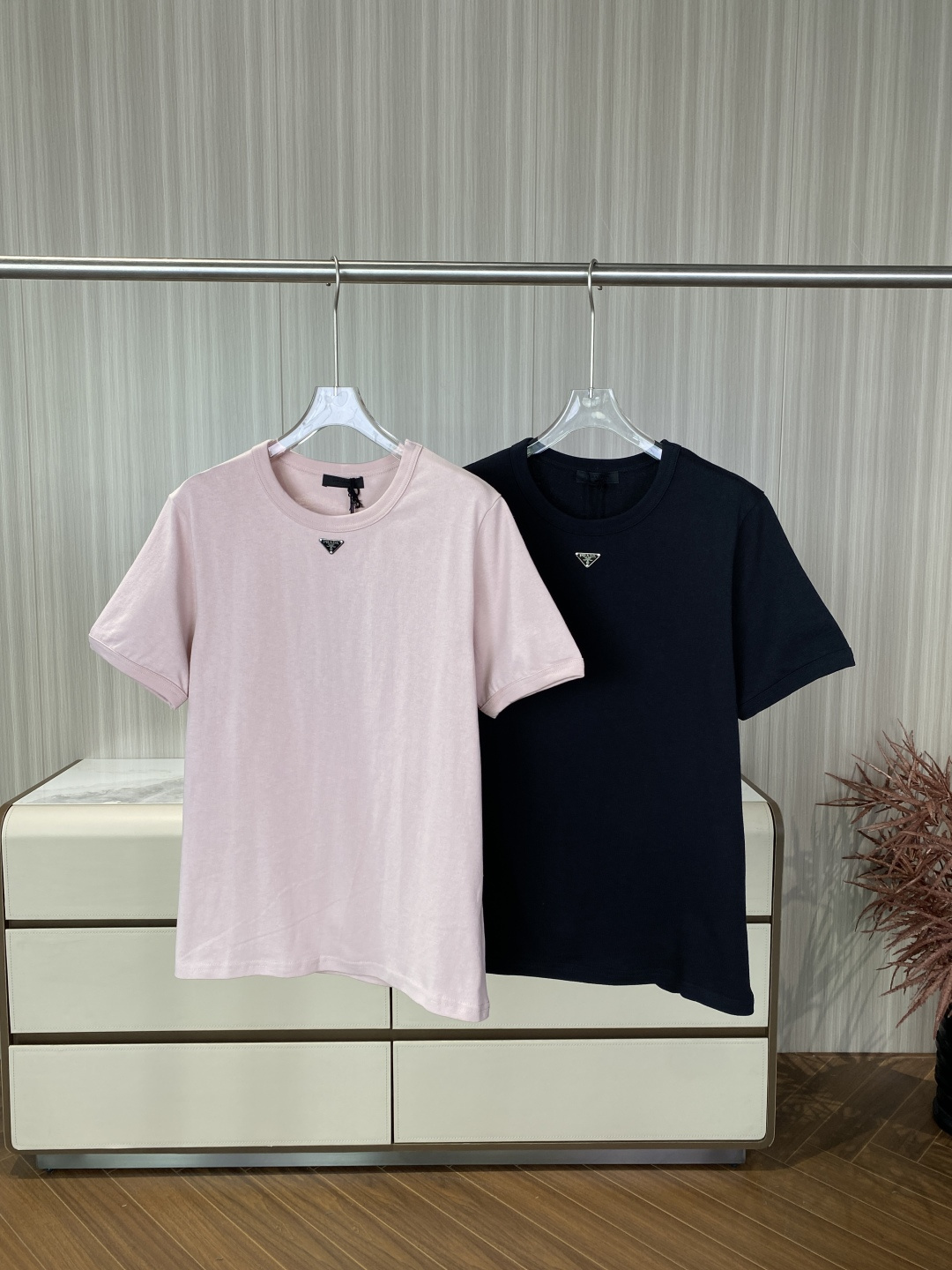 NO:873295,(Original customization) Prada classic metal triangle logo T-shirt. Iconic triangle logo. The metal enamel triangle logo is used on the chest, fixed with four rivets, and engraved with the words 'PRADA MILANO DAL 1913'. It is one of the most recognizable symbols of the brand. The tailoring is a classic fit. The ribbed round neck uses two-pin seaming technology. The cuffs and hem are flat stitched. The overall line is neat and not flattering. Color scheme  The two basic colors of nude pink and black are low-key and versatile, and can be easily integrated into various scenes such as commuting and leisure. The main fabric is made of high-quality combed cotton, which is soft and skin-friendly, has good breathability, and is not easy to deform or pill after washing. It is made of metal enamel with triangular logo technology, with smooth edges and firm rivets, which are not easy to fall off or oxidize, improving the overall texture.  Wearing suggestions: It is recommended to choose normal size, if you prefer an oversize effect, you can go up one size; you can wear it alone or layered with shirts and suit jackets to create a simple and light luxury style.,, prada, versace, jackets & coats, shirts, tees, t-shirt, business suit,19860909（原版定制） Prada 经典金属三角标T恤 标志性三角标 胸前采用金属珐琅三角徽标,以四颗铆钉固定,刻有「PRADA MILANO DAL 1913」字样,是品牌最具辨识度的符号之一. 版型剪裁 经典合身版型,罗纹圆领采用二本针锁边工艺,袖口与下摆为平车明线,整体线条利落,不挑身材. 配色方案 裸粉色与黑色两种基础色,低调百搭,可轻松融入通勤、休闲等多种场景. 主体面料优质精梳棉,触感柔软亲肤,透气性佳,洗后不易变形、起球. 三角标工艺金属珐琅材质,边缘打磨光滑,铆钉牢固,不易脱落或氧化,提升整体质感. 穿着建议建议选择正常尺码,若偏好oversize效果可大一码；可单穿或叠搭衬衫、西装外套,打造简约轻奢风格.,,prada,versace,jackets & coats,shirts,tees，t-shirt,business suit,,Women's clothing