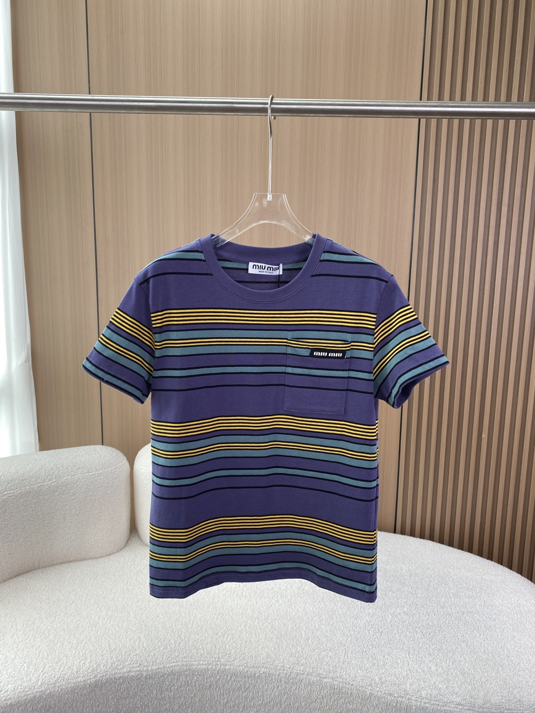 NO:835734,MIU MIU 2026 Early Spring Striped Pocket Short-Sleeved T-shirt This is the iconic item of the Miu Miu 2026 Early Spring series, with blue/bottle green/yellow stripes. Core design and features The style positioning is inspired by men's clothing, integrating retro college style and casual sense. The striped contrast design is full of vitality and is the representative of the brand's iconic 'miu girly feel'.  Fabric and fit: 100% cotton fabric, made of long-staple cotton jersey fabric, which is skin-friendly, breathable, has a muscular feel, and is not easy to collapse; the straight fit is not flattering on the figure, slim and versatile. Highlight details: chest patch pocket design, with 'miu miu' letter logo embroidered on the pocket, which is a highly recognizable brand logo. The combination of blue, yellow, and green stripes is rich in layers, visually more lively and youthful.  The basic style of round neck + short sleeves is suitable for wearing alone or layered with a white shirt and vest. Suggestions for matching: For casual style, pair with straight jeans, a baseball cap and canvas shoes to create an American retro feel. For college style, layer a white long-sleeved shirt with a pleated skirt and loafers to restore the classic miu style. For commuting style, wear a blazer and choose wide-leg trousers as bottoms to balance the sweet and cool look.  With its retro stripes and exquisite logo, this T-shirt has become a popular item in the early spring of 2026. It is suitable for daily outings and can also meet the needs of casual and mature style.,,miumiu,loafers,skirts,jeans,jackets & coats,shirts,T-shirt,tees,t-shirt,business suit,hats,19860909MIU MIU 2026早春条纹口袋短袖T恤 这是Miu Miu 2026早春系列的标志性单品,配色为蓝/瓶绿/黄条纹. 核心设计与特点 风格定位灵感源自男装,融合复古学院风与休闲感,条纹撞色设计充满活力,是品牌标志性的“miu系少女感”代表. 面料与版型100棉面料,采用长绒棉平纹针织面料,亲肤透气且有筋骨感,不易软塌；直筒版型,不挑身材,显瘦百搭. 细节亮点 胸前贴袋设计,袋口绣有“miu miu”字母徽标,是辨识度极高的品牌标识. 蓝、黄、绿三色条纹组合,层次丰富,视觉上更显活泼减龄. 圆领+短袖基础款型,适合单穿或叠穿白衬衫、背心. 搭配建议 休闲风搭配直筒牛仔裤、棒球帽与帆布鞋,打造美式复古感. 学院风叠穿白色长袖衬衫下摆,搭配百褶裙与乐福鞋,还原经典miu系穿搭. 通勤风外搭西装外套,下装选择阔腿西裤,平衡甜酷感. 这款T恤凭借复古条纹与精致徽标,成为2026早春热门单品,既适合日常出街,也能满足轻熟风穿搭需求.,,miumiu,loafers,skirts,jeans,jackets & coats,shirts,T-shirt,tees，t-shirt,business suit,hats,,Women's clothing