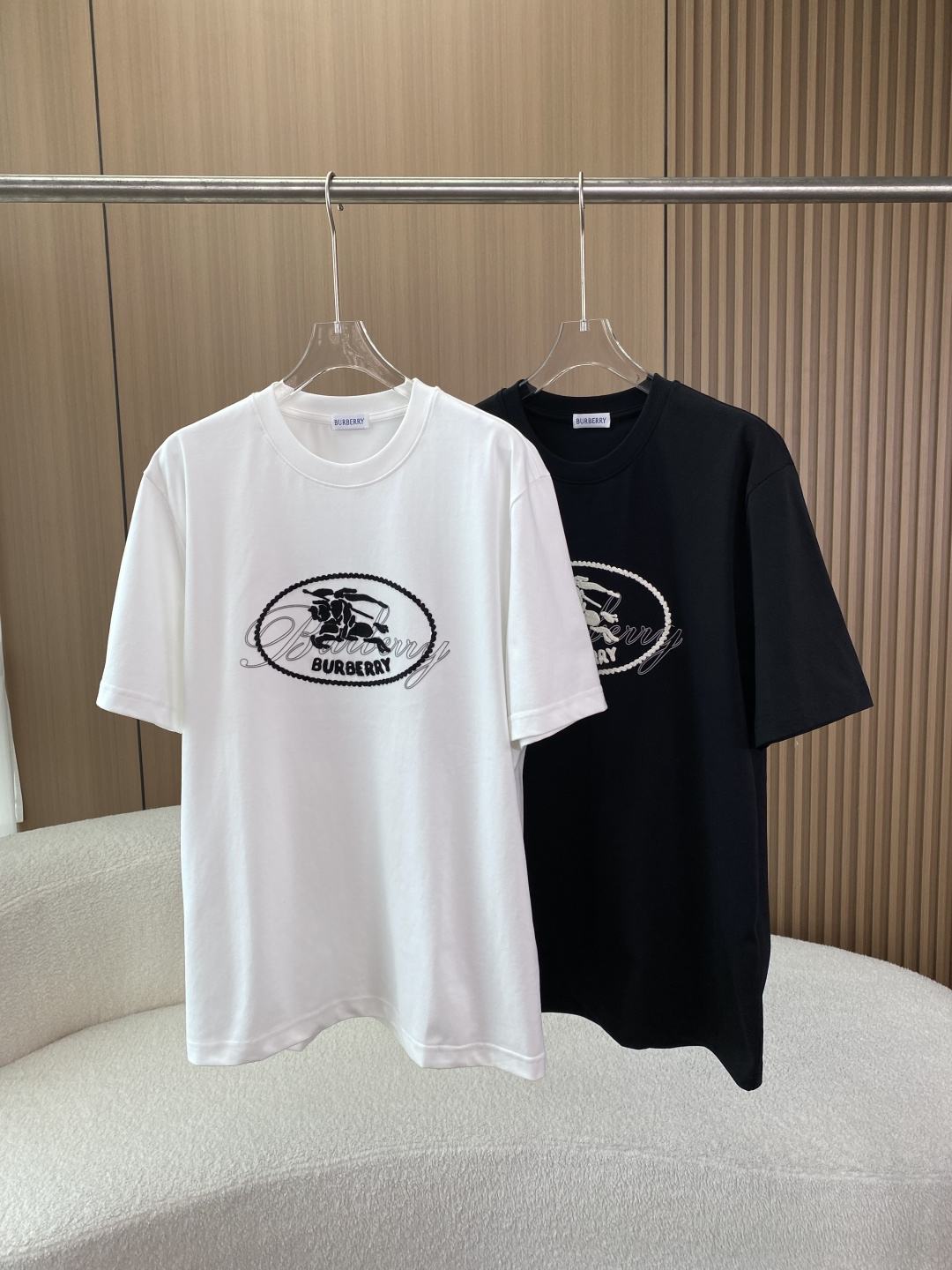 NO:841709,(Original customization) BURBERRY equestrian knight logo oval embroidery round neck short-sleeved T-shirt!  This is a round-neck short-sleeved T-shirt with oval embroidery of the equestrian knight logo launched by the British luxury brand BURBERRY (commonly known as Burberry). It is a special item of the brand that combines classic equestrian elements with modern casual style. 1. Brand background and design concept BURBERRY was founded by Thomas Burberry in Basingstoke, England in 1856. It is the benchmark for British luxury brands. The core logo includes the classic Vintage plaid and the equestrian knight logo (EKD). 1.  Core design elements: The main pattern is embroidered with an oval border on the chest, and the two classic symbols of the brand are integrated inside. The EKD logo, the brand’s iconic knight pattern with a shield and knight, is derived from the brand badge, symbolizing the spirit of chivalry and the British aristocratic bloodline; the cursive brand oval is surrounded by the handwritten letters 'BURBERRY', which is retro and elegant, and forms a layer with the knight logo; the bottom of the logo oval is printed with the capital 'BURBERRY' brand logo to enhance recognition.  Color matching logic: The white model uses black embroidery, with sharp black and white contrast, highlighting the exquisite pattern; the black model uses white/off-white embroidery, which is low-key yet high-end texture, in line with BURBERRY's 'low-key luxury' brand tone. 2. Design style The item combines retro British style and modern casual style. The embroidered pattern on the front avoids the monotony of solid-color T-shirts without being too ostentatious, making it suitable for daily wear and light social scenes; the same version for men and women adapts to the needs of all genders.  2. Style and tailoring This T-shirt adopts a conventional loose straight fit, which is an all-purpose tailoring that is not particular about your figure. The specific features are as follows: 1. The neckline is designed with a high weight ribbed round neck, the ribbing has excellent elasticity and resilience, and reinforced strips are added on the inside. It will not be easily deformed after repeated washing, and the collar will not collapse, and the neckline will not get stuck when wearing necklaces and other accessories; 2.  The body is straight cut and the length is moderate. It can cover the upper edge of the buttocks when worn normally. It can be worn alone or paired with a suit, knitted cardigan and other jackets; 3. The sleeves are of regular short sleeve length, and the cuffs are double-strand seamed. The threads are neatly routed and there are no problems with threading or curling. The sleeves are loose and not tight, and do not restrict arm movements; 3. Fabric and process details 1. Fabric composition: Main fabric cotton, customized high-count combed cotton from Portugal (washed label marked 'MADE IN'  PORTUGAL'), the weight is about 240-260g. The fabric is thick and crisp, not thin and soft, breathable and sweat-absorbent, not stuffy when worn in summer, and has been pre-shrunk, with low shrinkage after multiple washings; the neck fabric is 97 cotton + 3 spandex (ELASTHAN), adding a small amount of spandex to improve the elasticity of the neckline, taking into account the skin-friendliness of pure cotton and the resilience of the fabric, making it less likely to loosen after long-term wear. 2. Embroidery process  The chest logo is made of multi-thread high-density three-dimensional embroidery, which is the core quality of the genuine product. The stitching process is tight and full, and each stitch is evenly and neatly routed, with no skipping, missing stitches, burrs, or threading problems; the oval frame uses chain embroidery, with smooth lines and flat edges; the pattern of the equestrian knight logo has exquisite details, with clear character outlines and shield textures. The cursive letter font is the brand's exclusive handwriting, and the arc and spacing strictly follow the brand standards;  The texture shows that the embroidery fits the fabric well, without the risk of bulging or falling off. It has a three-dimensional concave and convex feeling when touched, and the texture is far superior to ordinary printing. 4. Wearing style and scene adaptation This T-shirt has strong compatibility and is suitable for a variety of styles and scenes 1. For daily casual wear, pair it with straight jeans, casual shorts, leggings, white shoes, and sneakers to create a British relaxed feeling, suitable for shopping, commuting, and daily travel; 2.  For light business/commuting, wear a suit jacket, a knitted cardigan, cigarette pants, or straight trousers to create a simple and advanced workplace look that balances formality and comfort; 3. Choose one size larger for the trendy street style to create an oversize style, pair it with overalls, wide-leg pants, dad shoes, baseball caps, and necklaces, which is suitable for fashionable people going out and at music festivals; 4.  Retro British style with plaid skirts, loafers, or with windbreakers and Chelsea boots to restore BURBERRY's classic British retro outfits, suitable for traveling and taking photos.,,burberry,burberry,versace,loafers,boots,skirts,shorts,jeans,jackets & coats,T-shirt,tees,t-shirt,business suit,necklace,hats,19860909（原版定制） 巴宝莉BURBERRY 马术骑士徽标椭圆刺绣圆领短袖T恤！ 这款是英国奢侈品牌BURBERRY（博柏利,俗称巴宝莉）推出的马术骑士徽标椭圆刺绣款圆领短袖T恤,属于品牌融合经典马术元素与现代休闲风格的特色单品. 一、品牌背景与设计理念 BURBERRY由Thomas Burberry于1856年在英国贝辛斯托克创立,是英伦奢侈品牌的标杆,核心标识包含经典Vintage格纹、马术骑士徽标（EKD）. 1. 核心设计元素 主体图案胸前采用椭圆边框刺绣,内部融合品牌两大经典符号 马术骑士徽标（EKD）品牌标志性的骑手持盾骑士图案,源自品牌徽章,象征骑士精神与英伦贵族血统； 草书品牌字样椭圆内环绕手写体“BURBERRY”字母,复古优雅,与骑士徽标形成层次； 下方标识椭圆底部印有大写“BURBERRY”品牌标识,强化辨识度. 配色逻辑白色款采用黑色刺绣,黑白对比鲜明,凸显图案精致；黑色款采用白色/米白色刺绣,低调中不失高级质感,符合BURBERRY“低调奢华”的品牌调性. 2. 设计风格 单品兼顾复古英伦风与现代休闲风,正面刺绣图案既避免了纯色T恤的单调,又不会过于张扬,适合日常穿搭与轻社交场景；男女同款版型,适配全性别穿搭需求. 二、版型与剪裁 这款T恤采用常规宽松直筒版型,属于不挑身材的万能剪裁,具体特征如下 1. 领口高克重罗纹圆领设计,罗纹弹性与回弹性优异,内侧加加固包条,多次洗涤后不易变形、不塌领,佩戴项链等配饰也不会卡领口； 2. 衣身直筒剪裁,衣长适中,正常穿着可覆盖臀部上缘,可单穿也可搭配西装、针织开衫等外套； 3. 袖型常规短袖长度,袖口采用双股线锁边工艺,走线工整,无脱线、卷边问题,袖身宽松不紧绷,不限制手臂活动； 三、面料与工艺细节 1. 面料成分 主体面料棉,为葡萄牙定制高支精梳棉（水洗标标注“MADE IN PORTUGAL”）,克重约240-260g.面料厚实挺括,无单薄软塌感,透气吸汗,夏季穿着不闷热,且经过预缩水处理,多次洗涤后缩水率低； 领口面料97棉 + 3氨纶（ELASTHAN）,添加少量氨纶提升领口弹性,兼顾纯棉的亲肤性与面料的回弹性,久穿不易松垮. 2. 刺绣工艺 胸前徽标采用多线高密度立体刺绣,是正品的核心品质体现 针脚工艺针脚紧密饱满,每一针走线均匀工整,无跳线、漏针、毛边、脱线问题；椭圆边框采用锁链式刺绣,线条流畅,边缘平整； 图案马术骑士徽标细节细腻,人物轮廓、盾牌纹理清晰,草书字母字体为品牌专属手写体,弧度、间距严格遵循品牌标准； 质感表现刺绣与面料贴合度高,无凸起、脱落风险,触摸时有立体凹凸感,质感远超普通印花. 四、穿搭风格与场景适配 这款T恤穿搭兼容性极强,适配多种风格与场景 1. 日常休闲单穿搭配直筒牛仔裤、休闲短裤、束脚卫裤,脚踩小白鞋、板鞋,打造英伦松弛感,适合逛街、通勤、日常出行； 2. 轻商务/通勤内搭西装外套、针织开衫,下搭烟管裤、直筒西裤,打造简约高级的职场造型,兼顾正式感与舒适度； 3. 潮流街头选大一码打造Oversize风格,搭配工装裤、阔腿裤,脚踩老爹鞋,搭配棒球帽、项链,适合潮人出街、音乐节； 4. 复古英伦风搭配格纹半身裙、乐福鞋,或搭配风衣、切尔西靴,还原BURBERRY经典英伦复古穿搭,适合出游、拍照.,,burberry,burberry,versace,loafers,boots,skirts,shorts,jeans,jackets & coats,T-shirt,tees，t-shirt,business suit,necklace,hats,,Women's clothing