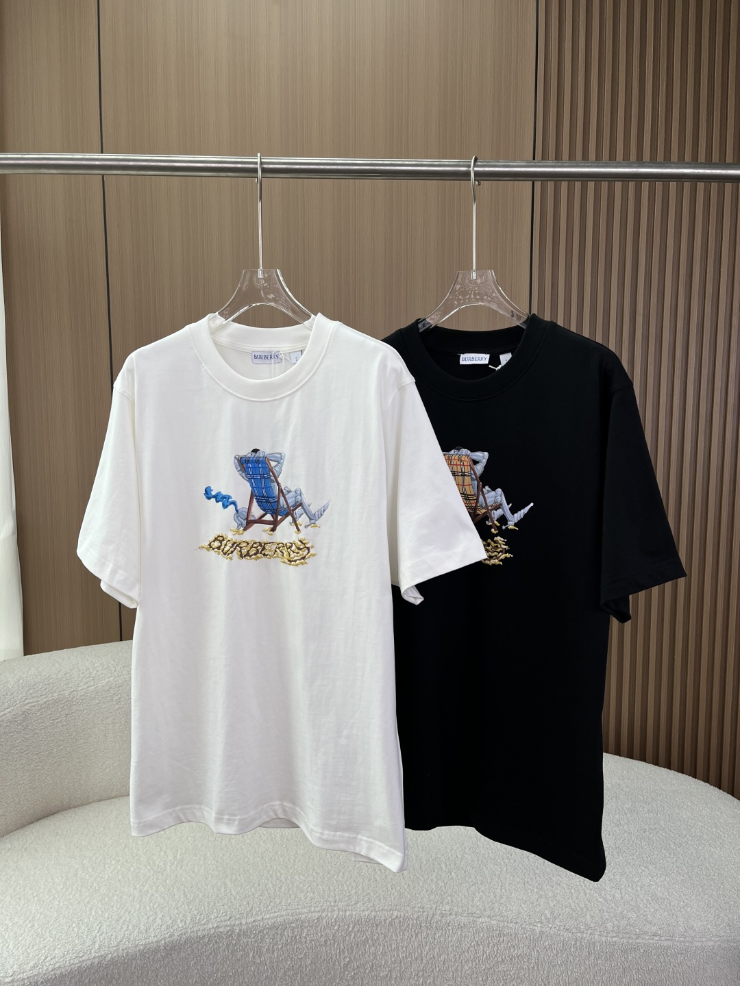 NO:832049,(Awesome in kind, original and customized) Burberry Lounge Chair Knight printed T-shirt!  The core pattern on the chest is a creative print of an equestrian knight (EKD) on a leisure lounge chair, which is a second creation of the brand's classic knight logo in a 'vacation style'. The lounge chair adopts the brand's iconic plaid (blue plaid for the white model, classic yellow-brown plaid for the black model), and the old-style Burberry letter logo below, which has both recognition and design. The color scheme is off-white and black, two basic versatile colors, suitable for different wear styles.  The style is casual and loose, regardless of figure, suitable for both men and women, and friendly to Asian figures. 2. Fabric and technology The main fabric is pure cotton plain weave, high weight material, thick and crisp to the touch, skin-friendly and breathable, and not easy to deform. The collar fabric is 97 cotton + 3 spandex, which increases the elasticity of the collar and prevents the collar from collapsing after long-term wear. The process uses screen printing technology, the pattern is clear and full, the color reproduction is high, and it is not easy to crack and fall off. 3. Details  The collar label is a white cloth label with the word BURBERRY hot-stamped. The font is clear and evenly spaced without blur or misalignment. The hang tag is light green and printed with the blue EKD logo and the word PRORSUM. The hot stamping process is exquisite. Design background and style 1. Design inspiration  This model belongs to Burberry's knight-themed creative series, which continues the brand's iconic equestrian knight logo (EKD, a classic brand symbol registered in 1901), while incorporating a modern casual and vacation design language, rejuvenating the classic elements of the traditional British luxury brand and adapting to daily wear scenarios. 2. Wearing Adaptation The style is suitable for casual, street, and light luxury commuting, and can be worn alone or layered with sweatshirts/denim jackets.  Can be paired with jeans, casual pants, or shorts to easily create a relaxed look. Suitable for both men and women.,,burberry,burberry,hoodie,sweatshirts,shorts,jeans,jackets & coats,tees,t-shirt,19860909（实物超赞、原版定制） Burberry 巴宝莉躺椅骑士印花T恤 ！ 核心图案胸前为休闲躺椅上的马术骑士（EKD） 创意印花,将品牌经典骑士徽标做了“度假风”二次创作,躺椅采用品牌标志性格纹（白色款为蓝格、黑色款为经典黄棕格）,下方搭配做旧风格的Burberry字母标识,兼具辨识度与设计感. 配色米白、黑色两款基础百搭色,适配不同穿搭风格. 版型休闲宽松版型,不挑身材,男女同款,对亚洲身材友好. 2. 面料与工艺 主体面料纯棉平织棉,高克重材质,手感厚实挺括,亲肤透气,不易变形. 衣领面料97棉+3氨纶,增加领口弹性,久穿不易塌领. 工艺采用丝网印花工艺,图案清晰饱满,色彩还原度高,不易开裂脱落. 3. 细节 领标白色布标,烫印BURBERRY字样,字体清晰、间距均匀,无模糊或错位. 吊牌淡绿色吊牌,印有蓝色马术骑士徽标（EKD）与PRORSUM字样,烫金工艺精致. 设计背景与风格 1. 设计灵感 该款属于Burberry骑士主题创意系列,延续了品牌标志性的马术骑士徽标（EKD,1901年注册的品牌经典符号）,同时融入了现代休闲、度假的设计语言,将传统英伦奢侈品牌的经典元素年轻化,适配日常穿搭场景. 2. 穿搭适配 风格休闲、街头、轻奢通勤多场景适配,可单穿、叠穿卫衣/牛仔外套. 搭配搭配牛仔裤、休闲裤、短裤均可,轻松打造松弛感穿搭. 人群男女同款.,,burberry,burberry,hoodie,sweatshirts,shorts,jeans,jackets & coats,tees，t-shirt,,Women's clothing