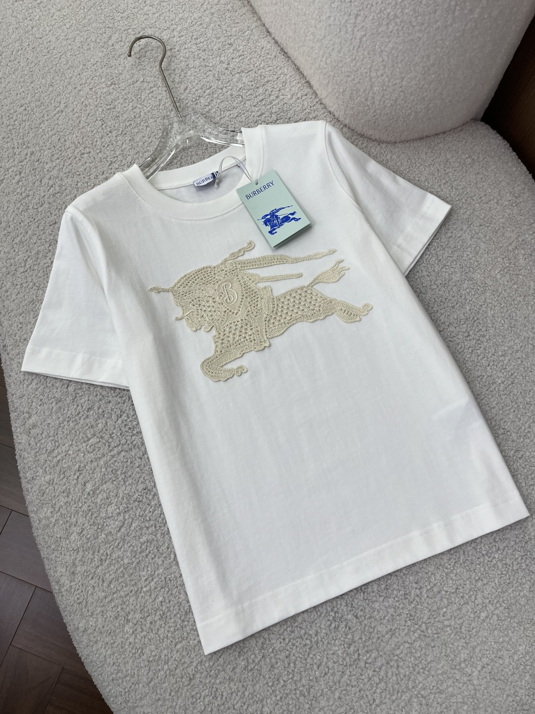 NO:884997,(Original customization) Burberry Women's Crochet Knight Logo T-shirt!  The core craftsmanship uses hand-made crochet/hollow embroidery technology on the chest to present the brand's iconic Equestrian Knight logo (EKD). The off-white crochet pattern and off-white background form a high-end texture of the same color. The letter 'B' on the knight's shield has clear details and exquisite three-dimensional craftsmanship. The version fits the right shoulder, is not picky, and is suitable for daily leisure, light business and other scenarios. The color is off-white, clean and versatile, weakening the publicity of the logo, and making it more low-key, light and luxurious. 2.  Fabrics and Ingredients The main fabric is pure cotton, which is skin-friendly and breathable. The high-gram weight material ensures a crisp feel and is not easy to deform. The collar fabric is 97 cotton + 3 spandex, which improves the elasticity of the collar and prevents the collar from collapsing after long-term wear. The decorative polyester fiber ensures the stiffness and shape of the crochet and is not easy to deform. Washing instructions: Gentle machine wash at 30°C. Bleaching, tumble drying, and high-temperature ironing are prohibited. It is recommended to wash the reverse side to avoid damage to the crochet. Design background and process 1.  Traceability of brand elements The Equestrian Knight logo (EKD) is the core symbol of the brand used by Burberry since 1901, representing the brand's British equestrian culture and craftsmanship. This model reinterprets the traditional logo with hand-crocheted technology, blending retro craftsmanship and modern casual style, and is a representative design of the brand's classic elements that are younger. 2. Craftsmanship highlights The crochet pattern adopts a hollow weaving structure, which has both three-dimensionality and breathability. It is visually more layered and textured, different from ordinary printed models.  The same color design weakens the presence of the logo and is suitable for consumers who pursue low-key luxury and do not like exaggerated logos. Outfit and care suggestions 1. Suitable outfits The style is suitable for casual, commuting, and light business. It can be worn alone or layered with denim jackets, suits, and windbreakers. It can be paired with jeans, casual trousers, and shorts to easily create a relaxed and high-end look.,,burberry,burberry,shorts,jeans,jackets &  coats,tees,t-shirt,business suit,19860909（原版定制） Burberry 巴宝莉女款钩花骑士徽标T恤 ！ 核心工艺胸前采用手工钩编/镂空刺绣工艺,呈现品牌标志性马术骑士徽标（EKD）,米白色钩花与米白底色形成同色系高级质感,骑士盾牌处的字母'B'细节清晰,工艺精致立体. 版型合身正肩版型,不挑身材,适配日常休闲、轻商务等多场景. 配色米白色,干净百搭,弱化logo的张扬感,更显低调轻奢. 2. 面料与成分 主体面料纯棉,亲肤透气,高克重材质保证挺括感,不易变形. 衣领面料97棉+3氨纶,提升领口弹性,久穿不易塌领. 装饰部分聚酯纤维,保证钩花的挺括度与造型感,不易变形. 洗涤说明30℃水温轻柔机洗,禁止漂白、滚筒烘干、高温熨烫,建议反面洗涤,避免钩花勾丝损坏. 设计背景与工艺 1. 品牌元素溯源 马术骑士徽标（EKD）是Burberry自1901年起使用的品牌核心符号,代表品牌的英伦马术文化与匠心工艺.该款将传统徽标以手工钩编工艺重新演绎,融合了复古手工艺与现代休闲风格,是品牌经典元素年轻化的代表设计. 2. 工艺亮点 钩花采用镂空编织结构,兼具立体感与透气性,视觉上更具层次与质感,区别于普通印花款. 同色系设计弱化了logo的存在感,适合追求低调轻奢、不喜欢夸张大标的消费者. 穿搭与护理建议 1. 穿搭适配 风格休闲、通勤、轻商务多场景适配,可单穿、叠穿牛仔外套、西装、风衣. 搭配搭配牛仔裤、休闲西裤、短裤均可,轻松打造松弛感、高级感穿搭.,,burberry,burberry,shorts,jeans,jackets & coats,tees，t-shirt,business suit,,Women's clothing