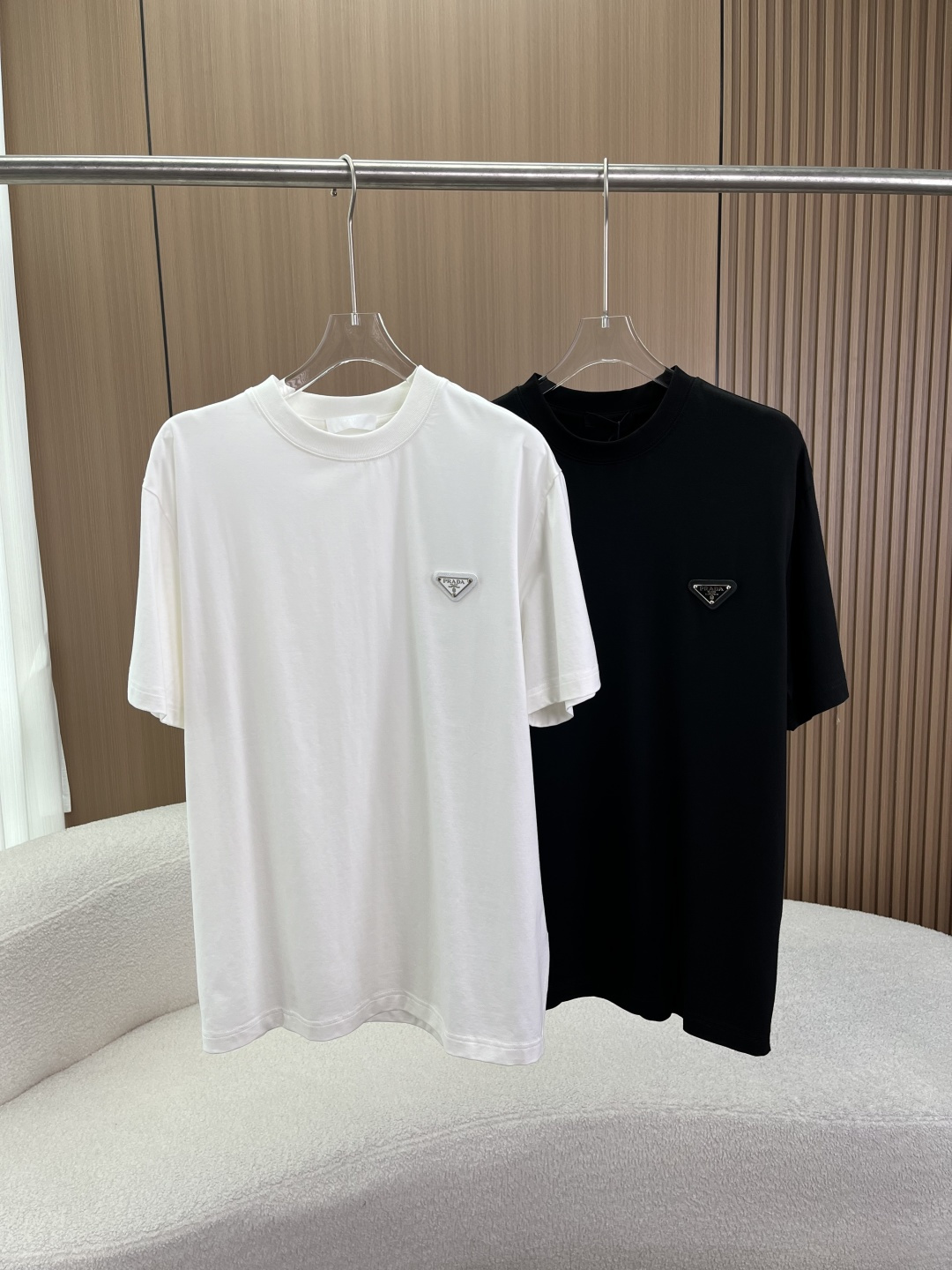 NO:808358,Prada classic metal triangle logo cotton T-shirt!  1. Fabric and material Core ingredient Cotton (BOMULL/cotton) The fabric features are made of high-count combed cotton, which has undergone special pre-shrunk treatment and high-density weaving process. The wearing experience is delicate and skin-friendly, has excellent breathability and strong sweat absorption ability; it also has excellent drape and stiffness, and is not easy to collapse or deform when worn. Say goodbye to the cheap and loose feeling of ordinary pure cotton. 2. Iconic design details  This T-shirt maximizes brand recognition through a minimalist design, and every detail highlights Italian sophistication. The metal triangle logo is located on the left chest of Prada's soul logo - the metallic triangle logo. The logo is made of zinc alloy die-casting technology, and the surface has been polished and oxidized. It has a thick texture, high gloss, and a strong three-dimensional effect. The metal logo forms a strong texture contrast with the body of the shirt, which is both low-key and luxurious, and highly brand-recognizable.  The minimalist round neck design adopts a highly elastic and tightly ribbed round neck, and the inner side of the collar is hemmed in the same color without unnecessary decoration. The neckline is extremely finely made and has been reinforced to prevent it from deforming or loosening after long-term wear and washing, and maintains neat lines. The simple cut adopts a slightly loose/dropped shoulder version, and is a unisex design for men and women. This cut is not body-selective, and can not only create a relaxed feeling for daily leisure, but also can be paired with suits and jackets to create a light and luxurious layering look, suitable for many scenes.  The hem and cuff hem adopt double-needle hemming technology, with neat routing and no excess thread; the cuffs are also flat hemmed, and the details reflect the brand's high-end quality control. The overall appearance is clean and neat, without redundant decoration. 3. Applicable scenarios: Daily casual strolls, outings, and family gatherings, creating a relaxed, comfortable and stylish daily look. For business and light socializing, paired with casual trousers and loafers, it is suitable for informal business meetings and afternoon tea, showing an elegant old-money style.  Lightly luxurious, layer it with a suit jacket, windbreaker or knitted cardigan to enhance the layering of the outfit. It is a classic combination of high-end 'old money style'.,, prada, prada, loafers, jackets & coats, jackets & coats, tees, t-shirt, business suit,19860909普拉达Prada 经典金属三角标纯棉T恤 ！ 1. 面料与材质 核心成分 棉（BOMULL/棉） 面料特性采用高支数精梳棉,经过特殊的预缩水处理与高密度织造工艺. 穿着体验触感细腻亲肤,透气性极佳,吸汗能力强；同时具备极佳的垂坠感与挺括度,穿着不易软塌、变形,告别普通纯棉的廉价松垮感. 2. 标志性设计细节 这件T恤通过极简的设计,将品牌辨识度拉满,每一处细节都彰显意式精致 金属三角徽标左胸位置是Prada的灵魂标识——金属质感三角徽标.徽标采用锌合金压铸工艺,表面经过抛光氧化处理,质感厚重、光泽度高,立体感极强.金属标与衣身形成强烈的质感对比,既低调奢华,又极具品牌辨识度. 极简圆领设计采用高弹紧密罗纹圆领,领口内侧为同色系包边,无多余装饰.领口做工极其精细,经过加固处理,长期穿着洗涤后不易变形、不松垮,保持利落的线条感. 简约版型剪裁采用微宽松/落肩版型,男女同款的中性设计.这种剪裁不挑身材,既能打造日常休闲的松弛感,也能搭配西装、夹克打造轻奢叠穿造型,适配多场景穿搭. 下摆与袖口下摆采用双针锁边工艺,走线工整,无多余线头；袖口同样为平整包边,细节处体现品牌的高端品控,整体干净利落,无冗余装饰. 3. 适用场景 日常休闲逛街、出游、家庭聚会,打造轻松舒适且不失格调的日常造型. 商务轻社交搭配休闲西裤、乐福鞋,适用于非正式商务会面、下午茶,展现儒雅的老钱风. 轻奢叠穿内搭西装外套、风衣或针织开衫,提升穿搭层次感,是高端「老钱风」的经典搭配.,,prada,prada,loafers,jackets & coats,jackets & coats,tees，t-shirt,business suit,,Women's clothing
