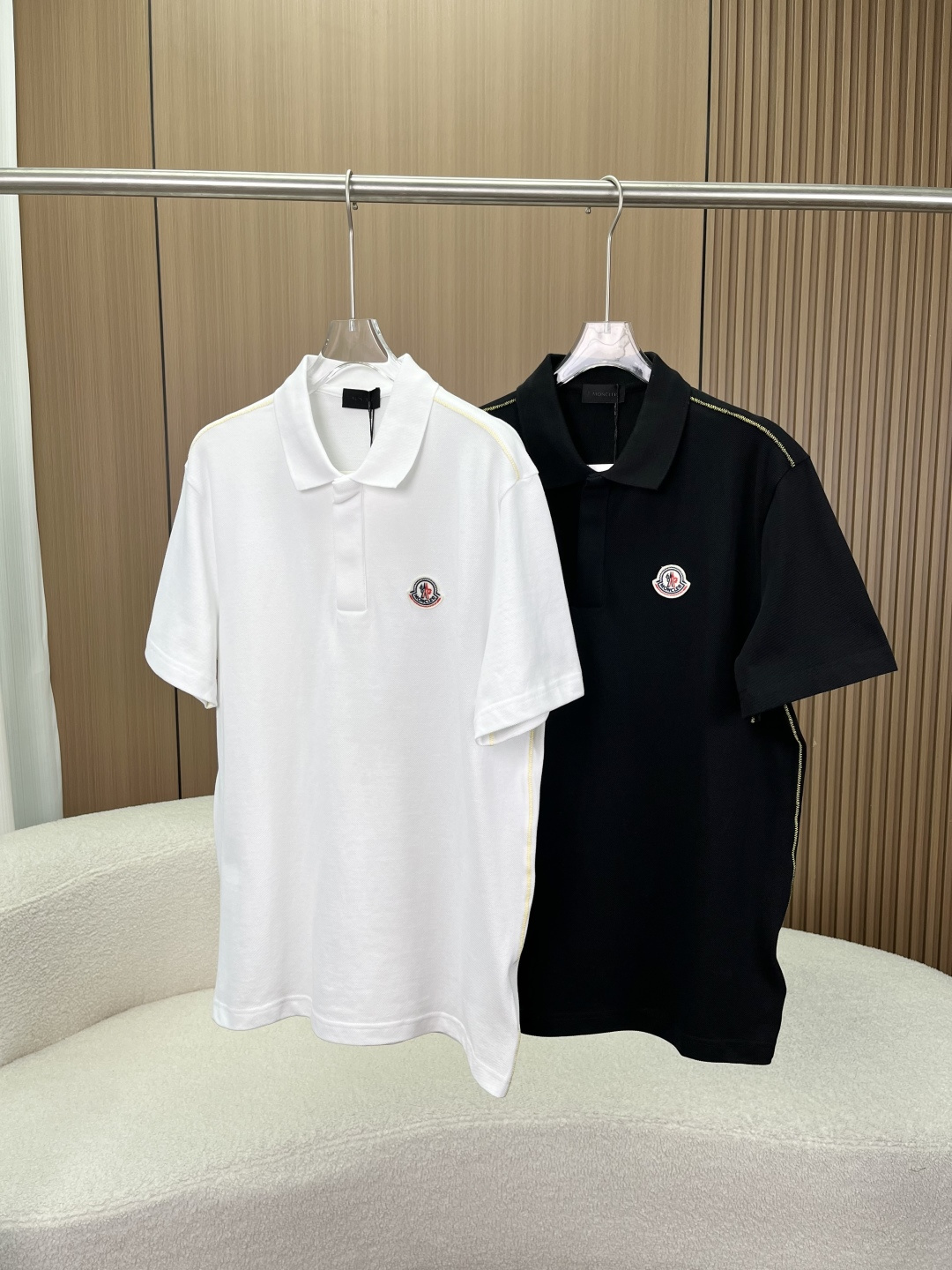 NO:824293,Moncler men's classic lapel Polo shirt. The main fabric is pique mesh cotton. It is made of high-count double-strand pique cotton fabric, which is a classic high-end fabric for Polo shirts. In terms of structure, the surface of the fabric is honeycomb mesh, and its breathability is much better than ordinary plain cotton. It will not make you sweaty when worn in summer. In terms of texture, the fabric is stiff and not easy to collapse, and it is not easy to deform after long-term wear. It also takes into account the skin-friendly softness to avoid the rough feeling of cheap pique cotton;  It has excellent anti-wrinkle performance and is not prone to wrinkles when worn for daily commuting and travel, and does not require frequent ironing. 2. Seams and craftsmanship details. The yellow topstitching on the side seams/shoulders is used as a design highlight, decorated with contrasting yellow stitches. The stitches are even and fine, with a stable number of stitches per inch, and no skipping or leaking stitches. This not only strengthens the body structure, but also adds a level of detail to the basic model;  The neckline is made of double-layer rib knitting. The neckline is stiff and not easy to collapse. It can maintain its straight shape even after multiple machine washes, avoiding the problem of loose and deformed necklines of ordinary Polo shirts. The hem and cuffs are made of double-needle lockstitch technology, with flat edges and no excess threads. The wiring is symmetrical and neat, reflecting the quality control standards of luxury goods. 3. Button details: Moncler brand letters are clearly printed on the surface of the buttons, with a warm texture and no cheap plastic feel;  The placket adopts a hidden half placket design, with evenly spaced buttons and smooth opening and closing, which not only retains the formal feel of the Polo shirt, but also avoids the tediousness of a full placket. 4. Brand emblem embroidery The Moncler badge on the left chest is the brand's iconic identification element. The bottom of the badge is a thick wool felt base, with a wavy edge at the edge, tight and full stitches, and no floating threads;  The embroidery colors are standard red, white and blue, with uniform colors and no color bleed or color difference; the brand letters 'MONCLER' are clearly embroidered, with natural stroke connections and no deformation or missed stitches; the overlock stitching on the edge of the badge is neat and fits closely with the body of the garment, without warping or falling off.,,Moncler,19860909Moncler（蒙口）男士经典翻领Polo衫 主体面料珠地网眼棉 采用高支双股珠地棉面料,这是Polo衫的经典高端面料 结构上,面料表面呈蜂窝状网眼,透气性远优于普通平纹棉,夏季穿着不闷汗； 质感上,面料挺括不易软塌,久穿不易变形,同时兼顾亲肤柔软度,避免廉价珠地棉的粗糙感； 抗皱性表现优异,日常通勤、旅行穿着不易起皱,无需频繁熨烫. 2. 缝线与工艺细节 侧缝/肩部黄色明线作为设计亮点,采用撞色黄色线迹装饰,针脚均匀细密,每英寸针数稳定,无跳线、漏线,既加固了衣身结构,也让基础款多了细节层次； 领口工艺采用双层罗纹针织包边,领口挺括不易塌,多次机洗后也能保持立挺形态,避免普通Polo衫领口松垮变形的问题； 下摆与袖口采用双针平缝工艺,边缘平整,无多余线头,走线对称工整,体现奢侈品的品控标准. 3. 纽扣细节 纽扣表面清晰印有Moncler品牌字母,质感温润,无廉价塑料感； 门襟采用隐藏式半开襟设计,纽扣间距均匀,开合顺滑,既保留了Polo衫的正式感,又避免了全开门襟的繁琐. 4. 品牌徽章刺绣 左胸的Moncler徽章是品牌标志性识别元素 徽章底部为厚实的羊毛毡底座,边缘呈波浪形锁边,针脚紧密饱满,无虚浮线头； 刺绣配色为标准的红白蓝三色,颜色均匀,无串色、色差；品牌字母“MONCLER”刺绣清晰,笔画衔接自然,无变形、漏针； 徽章边缘的锁边线迹工整,与衣身贴合紧密,不会出现起翘、脱落的情况.,,Moncler,,Women's clothing