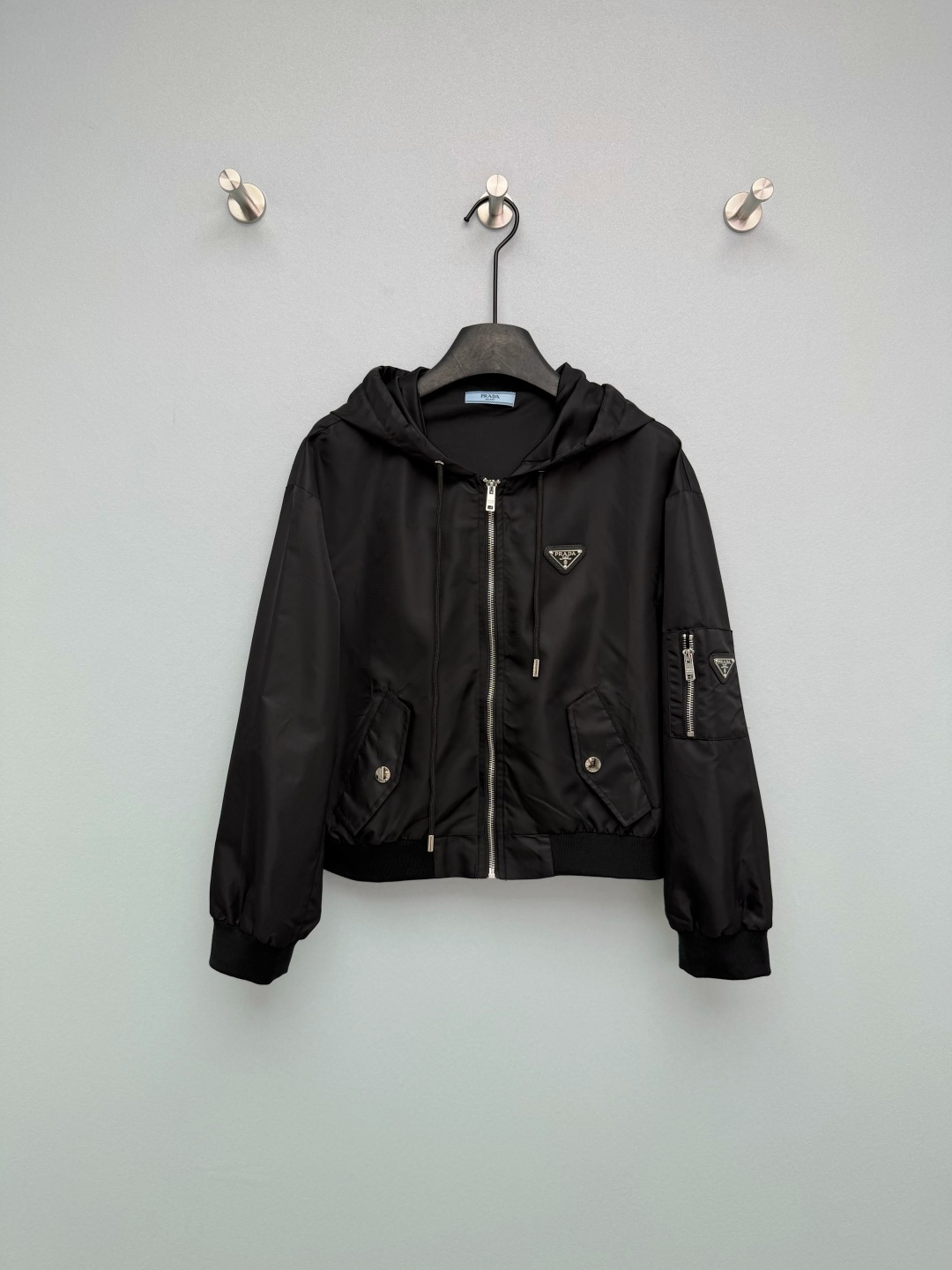 NO:776528,PRAD*26 new triangle logo hooded nylon flight jacket  It is made of high-density waterproof nylon fabric, which is smooth to the touch and has good windproof and anti-wrinkle properties. The upper body is light and has no weight-bearing feeling. The chest, arm pockets and zipper pullers are all equipped with the same color triangular metal LOGO, which has a full texture and instantly enhances the luxury of the item. It is P  The core identification point of home style. The black model is a timeless classic, cool and slim, suitable for all ages; the ice blue model is very 'golden', fresh and age-reducing, the fabric is crisp and not easy to wrinkle, easy to take care of, and has a good drape, which can well support the pattern!  The flight jacket is my destiny!  2 colors and 3 codes SML,Prada-clothing,prada,prada,jackets & coats,jackets & coats,hats,19860909PRAD*26新款三角标连帽尼龙飞行夹克外套 采用高密防水尼龙面料,触感顺滑且具备良好的防风抗皱性能,上身轻盈无负重感.胸前、臂袋及拉链头均配备同色系三角金属LOGO,质感饱满,瞬间提升单品奢华感,是P家风格的核心识别点.黑色款是永不过时的经典,酷飒显瘦,适配全年龄段；冰蓝款则极具“千金感”,清新减龄,面料挺括不易皱,方便打理,且垂坠感好,能很好地支撑版型！本命飞行夹克了！2色3码SML,普拉达-服装,prada,prada,jackets & coats,jackets & coats,hats,,Women's clothing