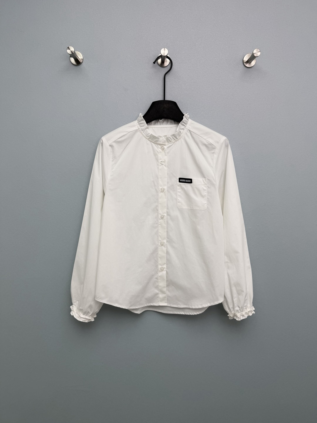 NO:777968,Miu Mi*26 new fungus stand-collar long-sleeved shirt. The collar and cuffs are double-layered with fungus stitching. The lines are neat, smart and sweet, which is the soul element of the sweet style. The left chest pocket is inlaid with the brand's classic black background and white text woven label, which is highly recognizable and full of light luxury. The details are exquisite. The slightly loose version is not flattering, and the flesh is directly hidden. The white is clean and refreshing, and the light blue is gentle and white, welding the girly feeling on the body!  2 colors and 3 codes SML, Miumiu-clothing, miumiu, shirts,19860909Miu Mi*26新款木耳边立领长袖衬衫 领口、袖口双层木耳边拼接,走线工整,灵动甜美,是甜系风格的灵魂元素.左胸口袋处镶嵌品牌经典黑底白字织唛,辨识度拉满,轻奢感十足,细节精致.微宽松版型不挑身材,拜拜肉直接藏住 白色干净清爽,浅蓝温柔显白,把少女感焊在身上！2色3码SML,缪缪-服装,miumiu,shirts,,Women's clothing